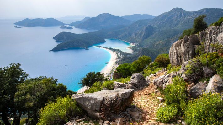 Bir tarafta yol boyunca görünüp kaybolan Akdeniz'in sonsuz maviliği, diğer tarafta ise yemyeşil çam ormanları, görkemli dağ manzaraları ve tarihe tanıklık eden antik şehirle...