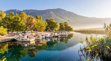 Bazen sadece doğanın sesini dinleyebileceğin, huzurlu bir an istediğini biliyoruz. G&ouml;kova tam da bu isteğini karşılamak i&ccedil;in seni bekliyor. Doğanın t&uuml;m c&ouml;mertliğini sergilediği bir yery&uuml;z&uuml; cenneti G&ouml;kova. Sakar Ge&ccedil;idi&rsquo;nde karşına &ccedil;ıkacak u&ccedil;suz bucaksız ova ve mavi k&ouml;rfez, ilk andan itibaren seni modern d&uuml;nyanın karmaşasından uzaklaştırıp huzurlu bir atmosfere davet edecek. G&ouml;kova&rsquo;da asırlık okalipt&uuml;s ağa&ccedil;larının g&ouml;lgesinde derin bir nefes alabilir ve kartpostal g&uuml;zelliğinde fotoğraflar &ccedil;ekebilirsin. Buz gibi Azmak Nehri ve karakteristik ahşap mimarisi ile &uuml;nl&uuml; Akyaka da G&ouml;kova&rsquo;nın incileri arasında yer alıyor. Ege&rsquo;nin en &ouml;zel k&ouml;şelerinden biri olan G&ouml;kova, deniz ve doğa tutkunlarının yanı sıra tarih meraklıları i&ccedil;in de her k&ouml;şesinde başka bir hazine gizliyor. G&ouml;kova nasıl bir yer? G&ouml;kova, Ege&rsquo;nin turkuaz suları ile &ccedil;am ormanlarını kusursuz bir uyum ile birleştiren masalsı bir yer. Akyaka&rsquo;nın el iş&ccedil;iliği ahşap evleri, buz gibi suyuyla &uuml;nl&uuml; Azmak Nehri ve tertemiz plajlar, G&ouml;kova atmosferini tamamlıyor. Sakar Ge&ccedil;idi&rsquo;nin b&uuml;y&uuml;leyici manzarası, bakir koylar, efsanevi Sedir Adası ve her zaman esen serin r&uuml;zg&acirc;rı ile G&ouml;kova, Ege&rsquo;nin en samimi sığınaklarından biri. G&ouml;kova ile Muğla arası ne kadar s&uuml;r&uuml;yor? Muğla merkezi ile G&ouml;kova arasındaki mesafe yaklaşık 28 kilometre. &Ouml;zel ara&ccedil;la yapacağın bu yolculuk, trafik durumuna bağlı olarak ortalama 25-30 dakika s&uuml;r&uuml;yor. Bu keyifli rota, b&ouml;lgenin en ikonik noktalarından Sakar Ge&ccedil;idi&rsquo;ni de kapsıyor. Buradan t&uuml;m G&ouml;kova K&ouml;rfezi&rsquo;ni kuş bakışı g&ouml;rmen m&uuml;mk&uuml;n. Eğer ulaşım i&ccedil;in Muğla merkezden kalkan toplu taşıma ara&ccedil;larını veya dolmuşları tercih edersen, yol &uuml;st&uuml;ndeki duraklamalarla birlikte yolculuk s&uuml;resi yaklaşık 45-50 dakikaya &ccedil;ıkabiliyor. G&ouml;kova&rsquo;da hangi b&ouml;lgede kalmak daha mantıklı? G&ouml;kova&rsquo;da konaklama tercihi, bir tatilden ne beklediğine g&ouml;re değişiyor. Eğer her şey elimin altında olsun, gece dışarı &ccedil;ıkayım, sabah nehre y&uuml;r&uuml;yeyim diyorsan, ahşap mimarili butik otellerin bulunduğu Akyaka merkezi en mantıklı se&ccedil;im. Doğayla baş başa kalmak, sabahları kuş sesleri ve nehrin serinliği ile uyanmak istiyorsan Azmak Nehri kıyısındaki huzurlu tesisleri tercih edebilirsin. &Ouml;nceliğin d&uuml;nya standartlarında bir u&ccedil;urtma s&ouml;rf&uuml; (kiteboard) deneyimi yaşamak ise bu sporun kalbinin attığı Ak&ccedil;apınar b&ouml;lgesindeki k&ouml;y evlerini veya kamp alanlarını se&ccedil;ebilirsin. Kalabalıktan uzak, izole bir tatil arıyorsan Akb&uuml;k Koyu, G&ouml;kova'nın o huzurlu ruhunu en saf haliyle hissetmeni sağlayabilir. {calismasaatleri}G&ouml;kova&rsquo;ya gitmeden &ouml;nce bilmen gerekenler En iyi ay: G&ouml;kova&rsquo;yı ziyaret etmek i&ccedil;in en ideal zamanlar mayıs, haziran, eyl&uuml;l ve ekim ayları. Temmuz ve ağustos ayları, hem sıcak hem de &ccedil;ok kalabalık. &Ouml;zellikle denizin sıcaklığının ideal olduğu, kalabalığın azaldığı ve doğanın yenilendiği eyl&uuml;l ayı, sakinlik arayanlar i&ccedil;in G&ouml;kova&rsquo;nın en g&uuml;zel zamanı. &Ouml;deme se&ccedil;enekleri: G&ouml;kova&rsquo;da restoranların, otellerin ve mağazaların &ccedil;oğunda kredi kartı ge&ccedil;erli. Ancak Azmak Nehri &uuml;zerindeki k&uuml;&ccedil;&uuml;k tekneler, k&ouml;y pazarları veya Akb&uuml;k gibi daha izole koylardaki işletmeler i&ccedil;in yanında mutlaka bir miktar nakit bulundurmanı &ouml;neririz. Ulaşım: G&ouml;kova&rsquo;ya en yakın havalimanı yaklaşık 1 saat uzaklıktaki Dalaman Havalimanı. G&ouml;kova&rsquo;ya Muğla merkezinden veya Marmaris'ten d&uuml;zenli dolmuş seferleri bulabilirsin. B&ouml;lgeyi keşfetmenin en konforlu yolu ise ara&ccedil; kiralamak. Akyaka merkezi, Ak&ccedil;apınar ve Aşıklar Yolu gibi d&uuml;z rotaları keşfetmek i&ccedil;in bisiklet de kiralayabilirsin. İnternet: G&ouml;kova&rsquo;da otellerin, kafelerin ve restoranın &ccedil;oğunda &uuml;cretsiz Wi-Fi hizmeti bulabilirsin. Şehir merkezinde ve ana yollarda mobil veri &ccedil;ekim g&uuml;c&uuml; olduk&ccedil;a y&uuml;ksek. Ancak k&ouml;rfezin i&ccedil; kısımlarında, denizin ortasındaki teknelerde veya Akb&uuml;k Koyu'na giden virajlı yollarda internet sinyalinde zaman zaman kısa s&uuml;reli kesintiler yaşanabiliyor.{/calismasaatleri} {insightBoxStart}G&ouml;kov​a seyahatin i&ccedil;in ipu&ccedil;ları En iyi fotoğraf noktası: G&ouml;kova&rsquo;nın g&ouml;rkemli manzarasını tek bir kareye sığdırmak i&ccedil;in ilk uğraman gereken yer Sakartepe Seyir Terası. Buradan k&ouml;rfezin turkuaz denizi ile ovaların yeşilini bir arada g&ouml;rebilirsin. G&uuml;n&uuml;n ilk ışıklarında veya g&uuml;n batımı &ouml;ncesinde Aşıklar Yolu'nun dev okalipt&uuml;sleri de masalsı bir atmosfer yaratıyor. Azmak Nehri&rsquo;nin su altındaki rengarenk bitki &ouml;rt&uuml;s&uuml; ve kristal berraklığı ise su altı fotoğraf&ccedil;ılığı i&ccedil;in Ege&rsquo;nin en canlı doğal setini sunuyor. Yeme-i&ccedil;me: G&ouml;kova&rsquo;nın ruhunu tam anlamıyla hissetmek i&ccedil;in sabah saatlerinde Azmak Nehri kıyısındaki restoranlarda, uzun ve sakin bir Ege kahvaltısı yapabilirsin. &Ouml;ğle molasında Ak&ccedil;apınar&rsquo;ın meşhur tost&ccedil;ularında yerel malzemelerle hazırlanan &uuml;nl&uuml; tostun ve yanında buz gibi ev yapımı ayranın tadına bakabilirsin. Akşam yemeğinde ise Akyaka&rsquo;nın butik restoranlarında Ege otlarıyla hazırlanan mezeleri ve g&uuml;nl&uuml;k taze deniz &uuml;r&uuml;nlerini tadarak g&uuml;n&uuml; lezzetli bir şekilde sonlandırabilirsin.{insightBoxEnd} {insightBoxStart}İpucu: En iyi otel fiyatlarını tek bir yerde g&ouml;rmek, se&ccedil;eceğin otel hakkında bilgi almak ve saniyeler i&ccedil;inde rezervasyon yapmak i&ccedil;in ENUYGUN'da otel araştırmasına başlayabilirsin.{insightBoxEnd} {hotel_search_form_banner} 1. G&ouml;kova K&ouml;rfezi Muğla&rsquo;nın en b&uuml;y&uuml;leyici manzaralarını sunan G&ouml;kova K&ouml;rfezi, kuzeyde Bodrum g&uuml;neyde ise Dat&ccedil;a Yarımadası arasında uzanıyor. K&ouml;rfez, mavinin her tonunu barındıran bir doğa harikası. K&ouml;rfezin kalbi sayılan Akyaka, geleneksel Nail &Ccedil;akırhan mimarisi ile inşa edilmiş ahşap evleri ve "Cittaslow" (Sakin Şehir) olarak seni huzur dolu bir atmosfere davet ediyor. B&ouml;lgenin simgesi haline gelen Azmak Nehri ise buz gibi suyu ve berraklığı ile &uuml;nl&uuml;. Azmak Nehri, sazlıklar arasında s&uuml;z&uuml;len tekneleri ve lezzet durakları ile ferahlatıcı bir mola noktası. G&ouml;kova K&ouml;rfezi&rsquo;nin asıl b&uuml;y&uuml;s&uuml; ise kıyı boyunca sıralanan ve her biri ayrı bir hik&acirc;ye saklayan bakir koylar. D&uuml;nyaca &uuml;nl&uuml; altın sarısı kumlarıyla Sedir Adası (Kleopatra Plajı), antik &ccedil;ağlardan g&uuml;n&uuml;m&uuml;ze ulaşan kalıntıları ve berrak suları ile masalsı g&ouml;r&uuml;n&uuml;yor. K&ouml;rfezin r&uuml;zg&acirc;rlı yapısı da burayı d&uuml;nya &ccedil;apında bir kiteboard (u&ccedil;urtma s&ouml;rf&uuml;) merkezi haline getirmiş durumda. G&ouml;kova K&ouml;rfezi, Akb&uuml;k&rsquo;&uuml;n dinginliğinden Sakartepe Seyir Terası&rsquo;nın nefes kesen manzarasına kadar her k&ouml;şesi ayrı bir g&uuml;zellik sunuyor. Konum Linki 2. G&ouml;kova Ovası Sakar Ge&ccedil;idi&rsquo;nin virajlı yollarından aşağıya doğru inerken, bir anda karşına G&ouml;kova Ovası&rsquo;nın u&ccedil;suz bucaksız yeşil manzarası &ccedil;ıkacak. Dağların bittiği yerde başlayan bereketli ova, Ege&rsquo;nin maviliğine kavuşmadan &ouml;nce doğanın sergilediği en huzurlu manzara. Yılın her d&ouml;nemi farklı bir renk ile s&uuml;slenen ovanın her yanı mısır tarlaları, narenciye bah&ccedil;eleri ve b&ouml;lgeye &ouml;zg&uuml; susam tarlaları ile kaplı. Burası sadece tarımsal bir merkez değil, aynı zamanda Sakar&rsquo;ın zirvesinden k&ouml;rfezin turkuaz sularına uzanan o meşhur manzaranın en canlı &ouml;rneği. Bisiklet s&uuml;rebileceğin veya doğa y&uuml;r&uuml;y&uuml;şlerine &ccedil;ıkabileceğin G&ouml;kova Ovası, ağa&ccedil;ların arasından s&uuml;z&uuml;len g&uuml;neş ışıklarını fotoğraflamak i&ccedil;in de eşsiz bir ortam sunuyor. Ova, aynı zamanda pek &ccedil;ok g&ouml;&ccedil;men kuşun da dinlenme noktası. Azmak Nehri&rsquo;nin tatlı sularıyla beslenen bu d&uuml;zl&uuml;k, Akyaka&rsquo;nın hareketli plajlarına ge&ccedil;meden &ouml;nce Ege&rsquo;nin o saf ve huzurlu ruhunu hissedebileceğin sakin bir ka&ccedil;ış rotası. Konum Linki 3. Sakartepe Seyir Terası G&ouml;kova&rsquo;nın Muğla&rsquo;dan Marmaris&rsquo;e doğru uzanan panoramik manzaralarını en g&uuml;zel Sakartepe Seyir Terası&rsquo;ndan izleyebilirsin. Deniz seviyesinden 900 metre y&uuml;kseklikteki teras, G&ouml;kova K&ouml;rfezi&rsquo;nin turkuaz sularını, Azmak Nehri&rsquo;ni ve Akyaka&rsquo;nın karakteristik mimarisini dev bir tablo gibi &ouml;n&uuml;ne serecek. Sakar Ge&ccedil;idi&rsquo;nin keskin virajlarından aşağıya inmeden &ouml;nce seyir terasında keyifli bir mola verebilirsin. Ege&rsquo;nin bu g&uuml;zel manzaralarını izlerken gezinin en &ouml;zel fotoğraflarını &ccedil;ekebilirsin.&nbsp; Sakartepe&rsquo;yi asıl b&uuml;y&uuml;leyici kılan şey ise &ouml;zellikle g&uuml;n batımında g&ouml;ky&uuml;z&uuml;n&uuml;n b&uuml;r&uuml;nd&uuml;ğ&uuml; kızıl manzara. G&ouml;kova Ovası&rsquo;nın yemyeşil tarlaları ile denizin maviliği arasındaki o keskin ge&ccedil;iş, fotoğraf tutkunları i&ccedil;in harika kompozisyonlar sunuyor. Havanın a&ccedil;ık olduğu bir g&uuml;nde ufukta Dat&ccedil;a Yarımadası&rsquo;nın sil&uuml;etini bile g&ouml;rebilirsin. Sakartepe&rsquo;de aşağıda s&uuml;z&uuml;len rengarenk u&ccedil;urtma s&ouml;rflerini de birer k&uuml;&ccedil;&uuml;k nokta gibi izleyerek ruhunu dinlendirebilirsin. Konum Linki 4. Sedir Adası Sedir Adası, G&ouml;kova K&ouml;rfezi&rsquo;nin ortasında masalsı bir durak. D&uuml;nyaca &uuml;nl&uuml; Kleopatra Plajı ile tanınan ada, doğa ve efsanenin i&ccedil; i&ccedil;e ge&ccedil;tiği eşsiz bir yer. Sedir Adası&rsquo;nın en b&uuml;y&uuml;k &ouml;zelliği ise sadece bu b&ouml;lgeye &ouml;zg&uuml; altın sarısı, k&uuml;&ccedil;&uuml;k ve yuvarlak yapılı &ouml;zel kumları. Efsaneye g&ouml;re bu kumlar, Romalı komutan Marcus Antonius tarafından sevgilisi Kleopatra i&ccedil;in Mısır&rsquo;dan gemilerle adaya getirilmiş. Kumlar koruma altında ve adadan &ccedil;ıkarılması yasak. Bu kumların d&uuml;nyada &ccedil;ok nadir olduğu, hatta sadece Sedir ve Girit&rsquo;te bulunduğu s&ouml;yleniyor. G&uuml;neş altında dahi asla ısınmayan bu kumlar, doğaya yeniden hayran kalmanı sağlayacak. Adada nadide kumların uzandığı cam berraklığındaki turkuaz sulara kendini bırakarak Maldivler benzeri adanın tadını &ccedil;ıkarabilirsin. Sedir Adası&rsquo;nın g&uuml;zelliği sadece plajı ile sınırlı değil. Ada, Kedrai Antik Kenti'nin etkileyici kalıntılarıyla tarih meraklılarını da kendine &ccedil;ekiyor. &Ouml;zellikle denize bakan konumuyla b&ouml;lgedeki en estetik yapılardan biri olan antik tiyatro, Karya d&ouml;neminin g&ouml;rkemini g&uuml;n&uuml;m&uuml;ze taşıyor. Şehir surları, tapınak kalıntıları ve asırlık zeytin ağa&ccedil;ları arasında yapacağın bir y&uuml;r&uuml;y&uuml;ş, seni binlerce yıllık mistik bir yolculuğa &ccedil;ıkaracak. Konum Linki {insightBoxStart}Yazar Notu: Sedir Adası&rsquo;na gitmek i&ccedil;in &Ccedil;amlı K&ouml;y&uuml; iskelesinden kalkan dolmuş teknelere binebilirsin. Bu yolculuk yaklaşık 15-20 dakika s&uuml;r&uuml;yor ve tekneler sezona g&ouml;re değişmekle birlikte genellikle sabah saatlerinden itibaren d&uuml;zenli aralıklarla hareket ediyor. Daha geniş bir rota sunan ve Akyaka limanından kalkan g&uuml;nl&uuml;k G&ouml;kova tekne turlarına da katılabilirsiniz. Adadaki Kedrai Antik Kenti&rsquo;ne M&uuml;zeKart ile &uuml;cretsiz girebilirsin.{insightBoxEnd} 5. Kleopatra Plajı G&ouml;kova K&ouml;rfezi&rsquo;nin en &ouml;zel noktalarından Kleopatra Plajı, sadece turkuaz deniziyle değil, &uuml;nl&uuml; altın sarısı kumlarıyla da bir efsaneye ev sahipliği yapıyor. Rivayete g&ouml;re Roma komutanı Marcus Antonius, sevgilisi Mısır Krali&ccedil;esi Kleopatra&rsquo;nın Sedir Adası&rsquo;nın adayı &ccedil;ok sevmesi ancak kumsalını yetersiz bulması &uuml;zerine, Mısır&rsquo;dan 60 b&uuml;y&uuml;k gemiyle bu &ouml;zel kumları buraya getirmiş. &ldquo;Oolitik" adı verilen her biri aynı boyutta, yuvarlak ve parlak bu kum taneleri, g&uuml;neş altında aşırı ısınmama gibi farklı &ouml;zelliklere sahip. Sedir Adası&rsquo;nın kalbindeki Kleopatra Plajı, Kedrai Antik Kenti&rsquo;nin kalıntıları ile i&ccedil; i&ccedil;e olmasıyla da etkileyici bir tarihsel dokuya sahip. Zeytin ağa&ccedil;larının arasından ge&ccedil;erek plaja ulaştığında, suyun altına uzanan antik duvarlar ve plajın arkasındaki 2.500 kişilik g&ouml;rkemli antik tiyatroyu g&ouml;rebilirsin. Kleopatra Plaj, sığ denizi ve beyaz kumları ile aileler i&ccedil;in de Ege&rsquo;nin en g&uuml;zel y&uuml;zme alanlarından biri olma &ouml;zelliği taşıyor. Konum Linki {insightBoxStart}Yazar Notu: Bu &ouml;zel kumları korumak amacıyla Kleopatra Plajı&rsquo;nda koruma altındaki kum alanına havlu veya terlikle girmek kesinlikle yasak.{insightBoxEnd} 6. Apollon Tapınağı G&ouml;kova K&ouml;rfezi&rsquo;nin kalbi Sedir Adası, sadece&nbsp; Kleopatra Plajı ile değil, antik &ccedil;ağın izlerini taşıyan Apollon Tapınağı ile de insanları kendine &ccedil;ekiyor. Kedrai Antik Kenti&rsquo;nin en kutsal alanı olan tapınak, g&uuml;neşin ve sanatın tanrısı Apollon&rsquo;a adanmış. Tapınak, adanın en y&uuml;ksek noktalarından birinde &ccedil;arpıcı manzaralar eşliğinde y&uuml;kseliyor. G&uuml;n&uuml;m&uuml;ze ulaşan karakteristik Dor d&uuml;zenindeki s&uuml;tun kalıntılar ve taşlar, binlerce yıl &ouml;ncesinin estetik anlayışını yansıtıyor. &Ccedil;evredeki asırlık zeytin ağa&ccedil;ları ise tapınağa b&uuml;y&uuml;leyici bir a&ccedil;ık hava m&uuml;zesi atmosferi veriyor. Apollon Tapınağı&rsquo;na yapacağın kısa y&uuml;r&uuml;y&uuml;şte masmavi G&ouml;kova K&ouml;rfezi&rsquo;nin antik taşlarla birleştiği &ccedil;arpıcı manzaralara şahit olacaksın. G&ouml;rkemli antik tiyatro ve surlarla birleşen bu kutsal alan, Sedir Adası&rsquo;nın sadece bir plajdan ibaret olmadığını, Karya d&ouml;neminin &ouml;nemli bir din&icirc; ve k&uuml;lt&uuml;rel merkezi olduğunu kanıtlıyor. &Ouml;zellikle &ouml;ğleden sonra g&uuml;neşinin antik mermerler &uuml;zerine d&uuml;şen altın sarısı ışıkları altında, Apollon Tapınağı&rsquo;nın en g&uuml;zel fotoğraflarını &ccedil;ekebilirsin. Konum Linki 7. Akyaka G&ouml;kova&rsquo;nın en pop&uuml;ler tatil cennetlerinden Akyaka, "Sakin Şehir" (Cittaslow) &uuml;nvanını sonuna kadar hak ediyor. Akyaka, tek tip mimarisiyle oluşan estetik ruhu ile seni ilk bakışta b&uuml;y&uuml;leyecek. Gazeteci ve şair Nail &Ccedil;akırhan&rsquo;ın başlattığı, beyaz duvarlar ve el iş&ccedil;iliği ahşap tavanlarla s&uuml;sl&uuml; bu evler, Akyaka&rsquo;nın sokaklarında karşına &ccedil;ıkacak. Akyaka&rsquo;nın yanındaki soğuk suları ile &uuml;nl&uuml; Azmak Nehri ise sazlıkları ve su altındaki rengarenk bitki &ouml;rt&uuml;s&uuml; ile doğal bir akvaryumu andırıyor. Nehir kıyısındaki restoranlarda kahvaltı yapmak ise burada en sevilen etkinliklerden. Akyaka, sadece huzur arayanların değil, adrenalin tutkunlarının da Ege&rsquo;deki en g&uuml;zel duraklarından biri. D&uuml;nyanın en iyi kiteboard (u&ccedil;urtma s&ouml;rf&uuml;) parkurlarından birine ev sahipliği yapan Akyaka&rsquo;nın geniş sahili, rengarenk bir manzara sunuyor. Sığ ve kumluk denizi ile &ccedil;ocuklu aileler i&ccedil;in de g&uuml;venli olan Akyaka Plajı ise doyasıya y&uuml;zmek i&ccedil;in ideal. İster nehrin buz gibi sularında serinleyin, ister r&uuml;zg&acirc;rın g&uuml;c&uuml;yle denizin &uuml;zerinde s&uuml;z&uuml;len Akyaka, modern hayatın karmaşasından uzaklaşıp nefes almak i&ccedil;in ger&ccedil;ek bir sığınak. Konum Linki 8. Nail &Ccedil;akırhan Akyaka evleri Akyaka&rsquo;nın &uuml;nl&uuml; manzarasını oluşturan ahşap evler, modern mimar&icirc; ile geleneksel T&uuml;rk evi estetiğinin en zarif buluşmasını sunuyor. Bu &ouml;zg&uuml;n akım, gazeteci ve şair olan Nail &Ccedil;akırhan&rsquo;ın 1970&rsquo;lerde geleneksel Ula evlerinden ilham alarak kendine inşa ettiği ev ile başlamış. &Ccedil;akırhan&rsquo;ın herhangi bir mimarlık eğitimi almadan ortaya koyduğu bu mimar&icirc; eser, doğayla kurduğu &ouml;zel bağ ile 1983 yılında prestijli Ağa Han Mimarlık &Ouml;d&uuml;l&uuml;&rsquo;ne layık g&ouml;r&uuml;ld&uuml;. Bug&uuml;n Akyaka&rsquo;nın tamamına yayılan bu evler, betonlaşmaya karşı doğayı koruyan bir kalkan g&ouml;revi g&ouml;r&uuml;yor. G&ouml;kova evlerinin en ayırt edici &ouml;zellikleri ise beyaz badanalı taş duvarları, yerel malzemeleri ve titizlikle işlenmiş devasa ahşap balkonları. Evlerin tavanlarından pencere pervazlarına kadar her k&ouml;şede g&ouml;rebileceğin el iş&ccedil;iliği ahşap oymalar ise evlere sıcak ve samimi bir ruh katıyor. Muğla mimarisinin simgesi olan ve r&uuml;zg&acirc;rı en iyi şekilde sirk&uuml;le edecek şekilde tasarlanan Muğla bacaları da bu evlerin &ccedil;atılarında estetik bir şekilde y&uuml;kseliyor.&nbsp; Konum Linki 9. Azmak Nehri Doğanın c&ouml;mert davrandığı yerlerden olan Azmak Nehri, suyunun berraklığı nedeniyle "doğal akvaryum" olarak biliniyor. Azmak Nehri&rsquo;nin kristal berraklığındaki sularında rengarenk su bitkileri, r&uuml;zg&acirc;rda dans eden sazlıklar ve canlı su altı yaşamını g&ouml;rebilirsin. Nehrin su sıcaklığı yıl boyu yaklaşık 8-10 derece civarında. Buz gibi sulara girmek b&uuml;y&uuml;k bir cesaret istese de Ege&rsquo;nin kavurucu sıcağında bu mikroklima etkisi seni anında serinletecek. O berrak ve buz gibi suya elini daldırdığında serinliğin parmak u&ccedil;larından v&uuml;cuduna yayıldığını hissedeceksin. Azmak Nehri&rsquo;ni keşfetmenin en klasik ve keyifli yolu ise sazlıkların arasından s&uuml;z&uuml;len geleneksel tekneler ile yapılan kısa turlar. Tekne ile nehrin denize kavuştuğu noktaya kadar ilerlerken &ouml;rdeklerin, kazların ve şanslıysan nadir g&ouml;r&uuml;len su samurlarının bu yolculuğa eşlik ettiğini g&ouml;rebilirsin. Nehir kıyısındaki asırlık ağa&ccedil;ların g&ouml;lgesindeki restoranlarda da sağlıklı bir Ege kahvaltısı yaparak g&uuml;ne başlayabilir veya akşam taze deniz &uuml;r&uuml;nlerinin tadını &ccedil;ıkarabilirsin.&nbsp; Konum Linki 10. &Ccedil;ınar Plajı &Ccedil;ınar Plajı, farklı bir G&ouml;kova K&ouml;rfezi manzarası g&ouml;rebileceğin keyifli sahil yolu ve el değmemiş g&uuml;zellikleri ile &uuml;nl&uuml;. &Ccedil;ınar Plajı&rsquo;nı b&ouml;lgedeki diğer kumsallardan ayıran en belirgin &ouml;zellik, kıyısını s&uuml;sleyen rengarenk p&uuml;r&uuml;zs&uuml;z &ccedil;akıl taşları ve arkasında y&uuml;kselen sarp kayalıkların yarattığı vahşi g&uuml;zellik. Plajın denizi ise Azmak Nehri&rsquo;nden gelen soğuk su akıntılarının etkisiyle olduk&ccedil;a serin. Ege&rsquo;nin en kavurucu yaz g&uuml;nlerinde bile soğuk kalan bu sularda anında ferahlayabilir, keyifli bir deniz g&uuml;n&uuml; yaşayabilirsin. Suyu kristal berraklığında olan &Ccedil;ınar Plajı, sığ olmaması ve y&uuml;ksek su altı g&ouml;r&uuml;ş mesafesiyle de şnorkelli dalış tutkunları i&ccedil;in g&uuml;zel bir keşif alanı. Kayalıkların diplerinde s&uuml;z&uuml;len balık s&uuml;r&uuml;lerini izleyerek, deniz keyfini bambaşka bir boyuta taşıyabilirsin. Plaj &ccedil;evresinde asırlık &ccedil;ınar ağa&ccedil;larının g&ouml;lgesinde dinlenebileceğin butik tesisler de hizmet veriyor.&nbsp; Konum Linki {{campaignsSlider}} 11. Ak&ccedil;apınar G&ouml;kova Ovası&rsquo;nın kalbinde yer alan Ak&ccedil;apınar, daha ilk andan seni b&uuml;y&uuml;leyecek, doğallığını g&uuml;n&uuml;m&uuml;ze kadar korumuş bir Ege k&ouml;y&uuml;. 1930&rsquo;lu yıllarda bataklığı kurutmak amacıyla dikilen devasa okalipt&uuml;s ağa&ccedil;ları ile &uuml;nl&uuml; Ak&ccedil;apınar, dinlendirici bir y&uuml;r&uuml;y&uuml;ş yapmak isteyenler i&ccedil;in eşsiz bir atmosfer sağlıyor. Ağa&ccedil;ların arasından s&uuml;z&uuml;len g&uuml;neş ışıkları altında bu yolda y&uuml;r&uuml;mek, G&ouml;kova seyahatinin en nostaljik ve g&uuml;zel anlarından biri olabilir. Ak&ccedil;apınar&rsquo;ı sadece bir ge&ccedil;iş noktası olmaktan &ccedil;ıkaran &ouml;zelliklerden biri de b&ouml;lgenin gastronomik simgesi haline gelen meşhur Ak&ccedil;apınar tostu. K&ouml;ydeki k&uuml;&ccedil;&uuml;k işletmelerde yerel malzemelerle hazırlanan bu &uuml;nl&uuml; lezzet, yanında buz gibi ev yapımı ayranla birleşince tam bir Ege klasiğine d&ouml;n&uuml;ş&uuml;yor. K&ouml;y&uuml;n hemen yanından başlayan Ak&ccedil;apınar Azmağı (Amazon Azmağı) ise kano tutkunları i&ccedil;in sazlıklar arasında gizemli bir keşif rotası sunuyor. Nehrin denize d&ouml;k&uuml;ld&uuml;ğ&uuml; noktadaki geniş kumsal da pop&uuml;ler kiteboard (u&ccedil;urtma s&ouml;rf&uuml;) merkezlerinden biri. Konum Linki {insightBoxStart}Yazar Notu: Amazon Azmağı&rsquo;nda ilk kez kano yapacaksan, tekne trafiğine (Amazon tur tekneleri) dikkat etmelisin. B&uuml;y&uuml;k tekneler ge&ccedil;erken oluşan dalgalardan etkilenmemek i&ccedil;in kano burnunu dalgaya dik tutmaya &ccedil;alışmalısın.{insightBoxEnd} 12. Aşıklar Yolu (Okalipt&uuml;s Yolu) G&ouml;kova Ovası&rsquo;nın ortasında y&uuml;kselen asırlık okalipt&uuml;slerin oluşturduğu bu &uuml;nl&uuml; yeşil t&uuml;nel, romantik manzarasıyla Aşıklar Yolu olarak biliniyor. Yol, sadece g&ouml;rsel bir ş&ouml;len sunmuyor, aynı zamanda b&uuml;y&uuml;k bir azmin hik&acirc;yesini de anlatıyor. Okalipt&uuml;s ağa&ccedil;ları, 1930&rsquo;lu yıllarda b&ouml;lgedeki bataklığı kurutmak ve sıtma hastalığıyla m&uuml;cadele etmek amacıyla d&ouml;nemin valisi ve "Halikarnas Balık&ccedil;ısı" Cevat Şakir Kabaağa&ccedil;lı&rsquo;nın &ouml;nc&uuml;l&uuml;ğ&uuml;nde dikilmiş. Bug&uuml;n ağa&ccedil;lar, g&ouml;ky&uuml;z&uuml;n&uuml; kapatan devasa bir doğal kemere d&ouml;n&uuml;şm&uuml;ş durumda. Aşıklar Yolu boyunca ilerlerken ağa&ccedil;ların arasından s&uuml;z&uuml;len ışık oyunlarını izleyebilir ve okalipt&uuml;slerin o kendine has taze kokusunu i&ccedil;ine &ccedil;ekebilirsin.&nbsp; Aşıklar Yolu, fotoğraf tutkunlarının ve romantik bir y&uuml;r&uuml;y&uuml;ş yapmak isteyenlerin vazge&ccedil;ilmez durağı. Yaklaşık 3 kilometrelik bu rotada y&uuml;r&uuml;yerek veya bisiklet s&uuml;rerek, zamanın yavaşladığını hissedebilirsin. Eğer fotoğraf &ccedil;ekeceksen, ağa&ccedil;ların yola d&uuml;şen karakteristik g&ouml;lgelerini yakalamak i&ccedil;in sabahın erken saatlerini veya g&uuml;n batımı &ouml;ncesini tercih edebilirsin. Konum Linki 13. Akb&uuml;k Koyu G&ouml;kova&rsquo;nın gizli akvaryumu olarak bilinen Akb&uuml;k Koyu, b&ouml;lgenin en sakin ve berrak denizine sahip. Akb&uuml;k&rsquo;&uuml;n denizi &ccedil;ok durgun ve şeffaf olduğu i&ccedil;in balık s&uuml;r&uuml;lerini bile kolaylıkla g&ouml;rebilirsin. Dağların g&ouml;lgesinde, r&uuml;zg&acirc;ra kapalı olan Akb&uuml;k Koyu, cam gibi suyu ile sana bir denizde değil de doğal ve devasa bir akvaryumda y&uuml;z&uuml;yormuş gibi hissettirecek. &Ccedil;evresindeki sınırlı yapılaşma ile doğallığını koruyan koy, modern hayatın g&uuml;r&uuml;lt&uuml;s&uuml;nden uzaklaşıp doğanın i&ccedil;inde dinlenmek isteyenler i&ccedil;in ideal.&nbsp; Akb&uuml;k Koyu&rsquo;nun asıl &ouml;zel kılan şey ise suyunun berraklığı sayesinde sunduğu y&uuml;ksek su altı g&ouml;r&uuml;ş mesafesi. Şnorkelli dalışlar yaparak kıyıdan sadece birka&ccedil; metre uzakta, kaya diplerinde gezinen balık s&uuml;r&uuml;lerini ve deniz altındaki zengin yaşamı en ince detayına kadar izleyebilirsin. B&ouml;lgenin sit alanı olarak korunması da bu bakir g&uuml;zelliğin bozulmadan kalmasını sağlıyor. Akb&uuml;k Koyu&rsquo;na ulaşım biraz virajlı ve zor olsa da yol boyunca sana eşlik eden k&ouml;rfez manzarası buna değecek. Konum Linki G&ouml;kova'nın huzurlu atmosferi sana iyi geldiyse rotanı Muğla'nın hen&uuml;z keşfedilmemiş koylarına &ccedil;evirmeye ne dersin? O halde Muğla&rsquo;nın en g&uuml;zel koyları yazımız tam sana g&ouml;re.