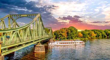 Prusya&rsquo;nın mirasını g&uuml;n&uuml;m&uuml;ze taşıyan Potsdam, Berlin&rsquo;in yanı başında masalsı bir d&uuml;nya sunuyor. Potsdam, Havel Nehri&rsquo;nin &ccedil;evresindeki parkları ve birbirine bağlanan g&uuml;zel g&ouml;lleri ile &uuml;nl&uuml;. UNESCO D&uuml;nya Mirası Listesi&rsquo;ndeki onlarca sarayla Potsdam, Avrupa&rsquo;nın en zarif k&uuml;lt&uuml;r başkentlerinden de biri. Brandenburg&rsquo;un bu b&uuml;y&uuml;leyici şehri, sadece tarih değil, doğası ve aristokratik ruhuyla da sana estetik bir g&ouml;rsel ş&ouml;len sunacak. Potsdam&rsquo;ın Rokoko tarzı saray bah&ccedil;elerinde kaybolabilir, casusluk filmlerine konu olmuş tarih&icirc; k&ouml;pr&uuml;lerinde y&uuml;r&uuml;yerek ge&ccedil;mişe bir yolculuğa &ccedil;ıkabilirsin. Hollanda Mahallesi&rsquo;nin karakteristik kırmızı tuğlalı evlerinden, Rus mimarisinin nadide &ouml;rneği Alexandrowka&rsquo;ya kadar her k&ouml;şede farklı bir k&uuml;lt&uuml;rel esinti bulabilirsin. Potsdam, "Almanya&rsquo;nın Versay&rsquo;ı" unvanını sonuna kadar hak ediyor. Potsdam nasıl bir şehir? Potsdam, g&ouml;rkemli Prusya krallığının tarih&icirc; mirası ile modern Alman yaşam tarzını kusursuz bir şekilde harmanlayan, saraylar ve bah&ccedil;eler şehri. Şehir, UNESCO D&uuml;nya Mirası Listesi'nde yer alan u&ccedil;suz bucaksız parklar, Sanssouci gibi masalsı saraylar ve Havel Nehri&rsquo;nin &ccedil;arpıcı manzaralar ile s&uuml;sl&uuml;. Potsdam, Avrupa'nın en estetik şehirlerinden biri. Potsdam ile Berlin arası ne kadar s&uuml;r&uuml;yor? Potsdam ile Berlin birbirine olduk&ccedil;a yakın ve entegre şehirler. Bu iki merkez arasındaki yolculuk, tercih ettiğin ulaşım aracına bağlı olarak 25 ila 45 dakika arasında s&uuml;r&uuml;yor. S-Bahn (S7 hattı), b&ouml;lgesel trenler (RE1, RE7, RB21) ile Potsdam Ana İstasyonu'na (Potsdam Hauptbahnhof) ulaşmak son derece kolay. Potsdam&rsquo;da hangi b&ouml;lgede kalmak daha mantıklı? Potsdam&rsquo;da tarih&icirc; merkezi Innenstadt ve Hollanda Mahallesi&rsquo;nin &ccedil;evresi, konaklamak i&ccedil;in en keyifli yerler. Bu b&ouml;lgelerden Brandenburg Kapısı ve Sanssouci Parkı gibi ikonik yapılara y&uuml;r&uuml;yerek kolayca ulaşabilirsin. Akşamları ise şık restoran, kafe ve butik mağazaların canlı atmosferinin tadını &ccedil;ıkarabilirsin. Daha sakin bir konaklama ve g&ouml;l manzarası arıyorsan, Heiliger See kıyısındaki villalar veya Berliner Vorstadt b&ouml;lgesi de g&uuml;zel se&ccedil;enekler sunuyor. {calismasaatleri}Potsdam&rsquo;a gitmeden &ouml;nce bilmen gerekenler Vize:&nbsp;Almanya, Schengen b&ouml;lgesinde yer aldığı i&ccedil;in T&uuml;rkiye Cumhuriyeti vatandaşlarının (bordo pasaport) ge&ccedil;erli bir Schengen vizesine sahip olması gerekiyor. Yeşil (hususi) pasaport sahipleri ise vizesiz giriş yapabilirler. En iyi ay:&nbsp;Potsdam&rsquo;ı ziyaret etmek i&ccedil;in en ideal zamanlar, mayıs-eyl&uuml;l ayları arası. Saray bah&ccedil;elerinin tam anlamıyla &ccedil;i&ccedil;ek a&ccedil;tığı ve a&ccedil;ık hava etkinliklerinin yapıldığı haziran ile temmuz ayları da şehrin en g&uuml;zel zamanları arasında. Para birimi:&nbsp;Almanya&rsquo;nın resm&icirc; para birimi Euro (&euro;). Şehirdeki d&uuml;kkan ve restoranların &ccedil;oğunda kredi kartı ge&ccedil;erli. K&uuml;&ccedil;&uuml;k kafeler veya hediyelik eşya tezg&acirc;hları i&ccedil;in ise yanında bir miktar nakit bulundurmanı &ouml;neririz. Dil:&nbsp;Potsdam&rsquo;da resm&icirc; dil Almanca. Ancak şehir bir turizm ve &uuml;niversite merkezi olduğu i&ccedil;in hemen her yerde &ccedil;ok iyi derecede İngilizce konuşuluyor. Ulaşım:&nbsp;Potsdam, Berlin&rsquo;e trenle sadece 25-45 dakika uzaklıkta. Şehir i&ccedil;inde ulaşım ise gelişmiş bir tramvay ve otob&uuml;s ağıyla sağlanıyor. D&uuml;z yollar sayesinde şehri keşfetmenin en keyifli yolu bisiklet kiralamak. Elektrik:&nbsp;Almanya&rsquo;da T&uuml;rkiye ile aynı olan standart Avrupa tipi (C ve F tipi) ikili priz sistemi kullanılıyor. T&uuml;rkiye'den g&ouml;t&uuml;receğin elektronik cihazlar, Almanya&rsquo;daki prizlere herhangi bir d&ouml;n&uuml;şt&uuml;r&uuml;c&uuml; (adapt&ouml;r) kullanmadan uyabilir. İnternet:&nbsp;Potsdam&rsquo;da otellerin, restoranların ve kamu binalarının &ccedil;oğunda &uuml;cretsiz Wi-Fi mevcut. T&uuml;rkiye&rsquo;deki operat&ouml;rlerin yurt dışı paketlerini kullanarak veya yerel bir SIM kart edinerek internetten faydalanabilirsin. Berlin-Potsdam hattı boyunca mobil veri &ccedil;ekim g&uuml;c&uuml; olduk&ccedil;a y&uuml;ksek.{/calismasaatleri} {insightBoxStart}Potsdam seyahatin i&ccedil;in ipu&ccedil;ları En iyi fotoğraf noktası:&nbsp;Potsdam&rsquo;da en ikonik kareleri yakalamak i&ccedil;in Sanssouci Sarayı&rsquo;nın teraslı bah&ccedil;eleri, ilk durağın olmalı. Buradaki etkileyici &uuml;z&uuml;m bağları, manzaraya harika bir derinlik katıyor. G&uuml;n batımında ise Heiliger See kıyısından Marmorpalais'i (Mermer Saray) ve sarayın suya yansıyan sil&uuml;eti, masalsı fotoğraflar &ccedil;ekme şansı veriyor. Glienicke K&ouml;pr&uuml;s&uuml; de &ccedil;evresindeki saraylar ile Potsdam&rsquo;ın en pop&uuml;ler fotoğraf noktalarından biri. Yeme-i&ccedil;me:&nbsp;Potsdam&rsquo;ın ruhunu hissetmek i&ccedil;in Hollanda Mahallesi&rsquo;ndeki butik kafelerde mola verebilirsin. Burada meşhur Alman usul&uuml; peynirli kekini (Kasekuchen) mutlaka denemelisin. Akşam yemeği i&ccedil;in ise Alexandrowka b&ouml;lgesindeki tarih&icirc; ahşap evlerde sunulan geleneksel Rus mutfağını veya Havel Nehri kıyısındaki restoranlarda taze balık &ccedil;eşitlerini tadarak Potsdam gezine yerel lezzetler katabilirsin.{insightBoxEnd} 1. Nauen Kapısı (Nauener Tor) Potsdam&rsquo;ın en hareketli noktalarından olan Nauen Kapısı, şehrin ayakta kalan &uuml;&ccedil; tarih&icirc; kapısından biri. Nauen, Avrupa&rsquo;nın İngiliz Neogotik mimarisinin ilk &ouml;rneklerinden biri. 1755 yılında yapılan kapı, Orta &Ccedil;ağ kale mimarisini anımsatan sivri kuleleri ve kemerli ge&ccedil;işleriyle hemen dikkat &ccedil;ekiyor. Hollanda Mahallesi&rsquo;nin sonunda g&ouml;rebileceğin Nauen Kapısı, bir zamanlar şehri &ccedil;evreleyen surların bir par&ccedil;asıymış. Bug&uuml;n ise kapı, Potsdam&rsquo;ın tarih&icirc; merkezi ile modern dokusunu birbirine bağlayan estetik bir ge&ccedil;it. Nauen Kapısı ve &ccedil;evresi, şehrin en pop&uuml;ler buluşma noktaları arasında. Kapının &ouml;n&uuml;ndeki meydan ve sokaklar da şık kafeler, restoranlar ve barlarla dolu. &Ouml;zellikle akşam saatlerinde ışıklandırılan kulelerin yarattığı masalsı atmosfer, halkı ve turistleri burada &ccedil;ekiyor. Haftalık kurulan semt pazarları ve canlı sosyal hayatı ile Nauen Kapısı, Potsdam&rsquo;ın aristokratik ge&ccedil;mişini modern ve enerjik şehir k&uuml;lt&uuml;r&uuml;yle birleştiriyor. Konum Linki 2. Hollanda Mahallesi (Dutch Quarter) Potsdam&rsquo;ın en karakteristik ve b&uuml;y&uuml;leyici b&ouml;lgelerinden biri Dutch Quarter (Hollanda Mahallesi). Burası seni Almanya&rsquo;nın kalbinden alıp Amsterdam&rsquo;ın dar ve şirin sokaklarına taşıyacak. 1733-1742 yılları arasında inşa edilen mahalle, Avrupa'nın Hollanda dışındaki en b&uuml;y&uuml;k Hollanda tarzı mimar&icirc; topluluğuna sahip. Kırmızı tuğlalı cepheleri, karakteristik &uuml;&ccedil;gen &ccedil;atıları ve titizlikle korunmuş Barok dokusuyla mahalle, adeta bir film setini andırıyor. Toplam 134 evden oluşan mahalle, Potsdam&rsquo;ın en somut estetik yerlerinden. Hollanda Mahallesi, şehrin en pop&uuml;ler yaşam ve alışveriş merkezlerinden biri. Mahallenin dar sokaklarında y&uuml;r&uuml;rken antika d&uuml;kkanları, butik sanat galerileri, şık kafeler ve yerel tasarım mağazaları arasında kaybolabilirsin. &Ouml;zellikle hafta sonları &ccedil;ok hareketlenen mahallede Hollanda usul&uuml; taze krep kokuları eşliğinde a&ccedil;ık havada keyifli molalar verebilirsin. Her yıl d&uuml;zenlenen Lale Festivali (Tulpenfest) ve kışın kurulan Sinterklaas Noel Pazarı gibi etkinlikler ise Hollanda ruhunu en canlı haliyle deneyimlemek i&ccedil;in harika fırsatlar sunuyor. Konum Linki 3. Brandenburg Kapısı Potsdam&rsquo;ın Brandenburg Kapısı, &ccedil;oğu zaman Berlin&rsquo;deki adaşıyla karıştırılsa da aslında ondan yaklaşık 20 yıl daha eski. Kendine has bir ihtişama sahip tarih&icirc; kapı, 1770-1771 yıllarında Yedi Yıl Savaşları'ndaki zaferin anısına inşa edilmiş. Roma'daki Konstantin Takı'ndan ilham alınarak tasarlanan Brandenburg Kapısı, Potsdam&rsquo;ın &uuml;&ccedil; tarih&icirc; şehir kapısından en g&ouml;rkemli olanı. İlgin&ccedil; mimar&icirc; detaylara sahip kapının iki y&uuml;z&uuml;, iki farklı mimar tarafından tasarlanmış. Bu y&uuml;zden şehre bakan taraf ile dışarıya bakan taraf, birbirinden farklı dekoratif unsurlarla dolu. Anıtsal Brandenburg Kapısı, g&uuml;n&uuml;m&uuml;zde Potsdam&rsquo;ın en canlı noktalarından biri. Kapının &ccedil;evresinde şık d&uuml;kkanlar ve kafelerin sıralandığı Brandenburger Caddesi uzanıyor. Kapının &ouml;n&uuml;ndeki geniş Luisenplatz Meydanı ise fıskiyeleri ve dinlenme alanlarıyla turistlerin mola verdiği bir yer. Sanssouci Parkı'na olduk&ccedil;a yakın olan Brandenburg Kapısı, akşam saatlerindeki ışıklandırmasıyla fotoğraf&ccedil;ılara da eşsiz kareler yakalama fırsatı sunuyor.&nbsp; Konum Linki 4. Barberini M&uuml;zesi (Museum Barberini) Potsdam&rsquo;ın Eski Pazar Meydanı'nda (Alter Markt) bulunan Barberini M&uuml;zesi, şehrin k&uuml;lt&uuml;rel r&ouml;nesansının en g&ouml;rkemli sembollerinden. 2. D&uuml;nya Savaşı'nda yıkılan Barberini Sarayı'nın modern teknolojiyle yeniden inşa edilmesiyle a&ccedil;ılan m&uuml;ze, 2017 yılından beri Avrupa&rsquo;nın en &ouml;nemli sanat duraklarından. M&uuml;zenin en &ouml;nemli noktası ise Paris dışında Avrupa&rsquo;da en fazla Monet eserinin g&ouml;r&uuml;lebildiği, Empresyonist resim koleksiyonu. Claude Monet, Pierre-Auguste Renoir ve Berthe Morisot gibi ustaların eserlerini g&ouml;rebileceğin bu galeri, g&uuml;n ışığıyla aydınlanan geniş salonlarıyla adeta b&uuml;y&uuml;leyici bir g&ouml;rsel ş&ouml;len sunuyor. Barberini M&uuml;zesi, kalıcı koleksiyonunun yanı sıra ge&ccedil;ici sergileriyle de sanat d&uuml;nyasında ses getiriyor. Klasik modernizmden &ccedil;ağdaş sanata kadar uzanan geniş yelpazede k&uuml;rat&ouml;rl&uuml;k &ccedil;alışmalarını koleksiyonlarda inceleyebilirsin. Barberini M&uuml;zesi, sadece tablolarıyla değil, dijital rehberler ve interaktif &ouml;ğrenme alanlarıyla da modern bir m&uuml;ze deneyimi yaşatıyor.&nbsp; Konum Linki 5. Alexandrowka M&uuml;zesi UNESCO D&uuml;nya Mirası Listesi&rsquo;nde yer alan Alexandrowka, seni 19. y&uuml;zyılın geleneksel bir Rus k&ouml;y&uuml;ne davet ediyor. 1826-1827 yılları arasında inşa edilen meyve ağa&ccedil;ları arasındaki iki katlı evler, ince oyma iş&ccedil;ilikleri ile Rus mimarisinin en zarif &ouml;rneklerini Almanya&rsquo;nın kalbine taşıyor. Bu otantik evler arasında dolaşırken, Rus k&uuml;lt&uuml;r&uuml;n&uuml;n mistik dokusunu her k&ouml;şede hissedebilirsin.&nbsp; Altın kubbeleriyle parıldayan Alexander Newski Anıt Kilisesi de Potsdam&rsquo;ın en egzotik yapılarından biri. B&ouml;lgedeki evlerde hizmet veren m&uuml;ze-restoranlar, geleneksel Rus lezzetlerini denemek ve b&ouml;lgenin k&ouml;kl&uuml; tarihini &ouml;ğrenmek isteyenler i&ccedil;in ideal duraklar. Alexandrowka, iki b&uuml;y&uuml;k imparatorluk arasındaki derin dostluğun hik&acirc;yesini anlatan masalsı havasıyla Potsdam gezilerinin en &ouml;zel rotalarından biri. Konum Linki 6. Potsdam M&uuml;zesi (Sanat ve Tarih Forumu) Potsdam&rsquo;ın k&ouml;kl&uuml; ge&ccedil;mişine ışık tutan Potsdam M&uuml;zesi, Alter Markt&rsquo;taki g&ouml;rkemli Eski Belediye Binası (Altes Rathaus) i&ccedil;inde yer alıyor. M&uuml;ze, 18. y&uuml;zyıldan kalma Barok mimarisi ve tepesindeki d&uuml;nyayı sırtında taşıyan altın kaplama Atlas heykeliyle dikkat &ccedil;ekiyor. M&uuml;zenin koleksiyonları ise yaklaşık 1.000 yıllık yerel tarihi, Orta &Ccedil;ağ'dan g&uuml;n&uuml;m&uuml;ze uzanan geniş bir yelpazede sunuyor. Prusya kralları d&ouml;neminden 2. D&uuml;nya Savaşı sonrası yaşanan değişimlere ve Doğu Almanya yıllarına kadar uzanan bu yolculuk, interaktif sergiler ve zengin bir koleksiyonla anlatılıyor. M&uuml;zenin en dikkat &ccedil;ekici b&ouml;l&uuml;m&uuml; olan "Potsdam: Bir Şehir Tarih Yazıyor" sergisi, yaklaşık 1.300 metrekarelik bir alanda 1.000&rsquo;den fazla değerli par&ccedil;ayı bir araya getiriyor. Mobilyalardan kost&uuml;mlere ve end&uuml;striyel tasarımlara kadar her detay, Potsdam&rsquo;ın yaşayan bir k&uuml;lt&uuml;r merkezi olduğunu g&ouml;steriyor. Sanat meraklıları, yıl boyunca d&uuml;zenlenen &ouml;zel sergilerde yerel sanat&ccedil;ıların eserleri ve b&ouml;lgeye ait sanatsal akımlarını da m&uuml;zede g&ouml;rebilirler.&nbsp; Konum Linki 7. Aziz Nikolaos Kilisesi (St. Nicholas&rsquo; Church) Alter Markt&rsquo;ta ihtişamla y&uuml;kselen Aziz Nikolaos Kilisesi, Potsdam siluetini oluşturan en ikonik yapılardan. Kilise, &uuml;nl&uuml; Prusyalı mimarlar tarafından Neoklasik tarzda tasarlanmış. Kilisenin 77 metre y&uuml;ksekliğindeki turkuaz renkli g&ouml;rkemli kubbeleri, ilk dikkat &ccedil;eken &ouml;zellik. Roma'daki Aziz Petrus Bazilikası ve Londra'daki Aziz Paul Katedrali&rsquo;nden izler taşıyan kilise, Prusya&rsquo;nın mimar&icirc; dehasını yansıtan bir başyapıt kabul ediliyor. 2. D&uuml;nya Savaşı&rsquo;nda ağır hasar alan ve yenilenen kilise, g&uuml;n&uuml;m&uuml;zde hem bir ibadethane hem de şehrin direncinin sembol&uuml;. Aziz Nikolaos Kilisesi&rsquo;nin i&ccedil; b&ouml;l&uuml;m&uuml; ise Korint s&uuml;tunları ve pastel tonlardaki zarif s&uuml;slemeleriyle masalsı bir atmosfere sahip. Turistlerin en &ccedil;ok ilgisini &ccedil;eken şeylerden biri ise 42 metre y&uuml;kseklikteki seyir terası. Yaklaşık 200 basamakla ulaşılan bu terastan Potsdam&rsquo;ın tarih&icirc; merkezi, Barberini M&uuml;zesi, Havel Nehri ve Sanssouci Parkı&rsquo;nı kapsayan 360 derecelik panoramik manzarayı seyredebilirsin. Konum Linki 8. Potsdam Şehir Sarayı (Stadtschloss) Eski Kent (Altstadt) merkezinde gezebileceğin Potsdam Şehir Sarayı, şehrin kraliyet ge&ccedil;mişinin ve modern mimar&icirc; restorasyonun en etkileyici sembollerinden biri. Saray, ilk olarak 1600&rsquo;l&uuml; yıllarda inşa edildi ve zamanla muhteşem devasa bir Barok saraya d&ouml;n&uuml;şt&uuml;r&uuml;ld&uuml;. 2. D&uuml;nya Savaşı'nda ağır hasar g&ouml;ren saray, 2013 yılında yenilenerek adeta k&uuml;llerinden doğdu. Bug&uuml;n sarı tonlarındaki dış cephe ve g&ouml;rkemli heykellerle s&uuml;sl&uuml; &ccedil;atısıyla meydanı aydınlatan saray, Brandenburg Eyalet Parlamentosu'na ev sahipliği yapıyor. Potsdam Şehir Sarayı&rsquo;nın en b&uuml;y&uuml;leyici yanlarından biri de tarihin estetiği ile modern olanakları birleştirmesi. Sarayın avlusunda, d&ouml;nemin kraliyet ihtişamını hissedebilir ve mimar&icirc; detayları inceleyebilirsin. Sarayın yanındaki "Kader Kapısı" olarak bilinen Fortunaportal ise altın yaldızlı s&uuml;slemeleriyle b&ouml;lgenin en sevilen fotoğraf noktalarından. Potsdam Şehir Sarayı, Nikolaikirche ve Barberini M&uuml;zesi ile bir b&uuml;t&uuml;nl&uuml;k oluşturarak manzarayı tamamlıyor. Konum Linki 9. Filmmuseum Potsdam Potsdam&rsquo;ın tarih&icirc; merkezinde gezebileceğin Filmmuseum Potsdam, Almanya&rsquo;nın en eski film m&uuml;zesi olma unvanına sahip. Almanya&rsquo;nın sinematografik ruhunu keşfetmek isteyenler i&ccedil;in burası &ouml;nemli bir durak. 1685 yılından kalan m&uuml;ze binası da şehrin ayakta kalan en eski yapılarından biri olmasıyla dikkat &ccedil;ekiyor. Barok mimarisiyle dikkat &ccedil;eken yapı, Avrupa&rsquo;nın en b&uuml;y&uuml;k film platosu olan Babelsberg St&uuml;dyoları&rsquo;nın 100 yılı aşkın mirasına ev sahipliği yapıyor. M&uuml;zenin kalıcı sergisi olan "R&uuml;ya Fabrikası" ise bir filmin ilk fikirden galaya uzanan yolculuğunu interaktif bir şekilde ziyaret&ccedil;ilerine sunuyor. Filmmuseum&rsquo;da eski kameraları veya otantik kost&uuml;mlerin yanında ses montajı yapmak, oyunculuk yeteneklerini denemek veya film m&uuml;zikleri kurgulamak gibi etkileşimli deneyimler de yaşayabilirsin. M&uuml;zenin sinema salonu ise nadir bulunan sessiz filmlerin tarih&icirc; bir org eşliğinde canlı m&uuml;zikle g&ouml;sterildiği &ouml;zel seanslarıyla &uuml;nl&uuml;. Sergileri gezdikten sonra m&uuml;ze mağazasından sinema tarihine dair &ouml;zg&uuml;n hediyelikler alabilirsin.&nbsp; Konum Linki 10. Freundschaftsinsel (Dostluk Adası) Potsdam&rsquo;ın kalbinde akan Havel Nehri&rsquo;nin kollarının birleştiği noktada bulunan Freundschaftsinsel, şehrin en sevilen ka&ccedil;ış noktalarından biri. Turistik ada, tarih&icirc; şehir merkezine ve ana istasyona sadece birka&ccedil; dakikalık y&uuml;r&uuml;me mesafesinde. Freundschaftsinsel, &ouml;zellikle etkileyici bir botanik mirasa ev sahipliği yapmasıyla &uuml;nl&uuml;. İlkbahar ve yaz aylarında binlerce egzotik bitki ve rengarenk &ccedil;i&ccedil;eklerle s&uuml;slenen bah&ccedil;eler, adeta bir a&ccedil;ık hava sergisini andırıyor. Adanın &ccedil;evresini saran y&uuml;r&uuml;y&uuml;ş yollarında nehir manzarasının ve doğal atmosferin tadını &ccedil;ıkarabilirsin. Freundschaftsinsel, aileler ve sanat tutkunları i&ccedil;in de pek &ccedil;ok &ouml;zellik sunuyor. &Ccedil;ocuklar i&ccedil;in tasarlanmış geniş ve modern oyun parkı, ailelerin favorisi. Adanın d&ouml;rt bir yanını s&uuml;sleyen heykeller ve k&uuml;&ccedil;&uuml;k sanat galerisi ise doğal g&uuml;zelliklere k&uuml;lt&uuml;rel bir derinlik katıyor. Nehirde su sporları olanakları da sunuluyor. Dilersen mevsimine g&ouml;re sandal veya kano kiralayarak Potsdam&rsquo;ın g&uuml;zelliklerini su &uuml;zerinden farklı a&ccedil;ılardan g&ouml;rebilirsin. Konum Linki {{campaignsSlider}} 11. Sanssouci Parkı Potsdam denince akla gelen ilk yerlerden biri UNESCO D&uuml;nya Mirası Listesi'nde de yer alan ve Prusya'nın Versay'ı olarak bilinen Sanssouci Parkı. Yaklaşık 300 hektarlık devasa bir alana yayılan park, B&uuml;y&uuml;k Friedrich&rsquo;in "kaygısız" bir yaşam s&uuml;rme hayalinin ger&ccedil;eğe d&ouml;n&uuml;şm&uuml;ş hali. Parkta yapacağın y&uuml;r&uuml;y&uuml;şte Prusya krallığının g&uuml;c&uuml;n&uuml; simgeleyen g&ouml;rkemli fıskiyeleri, mitolojik heykelleri ve rengarenk &ccedil;i&ccedil;ek bah&ccedil;elerini keşfedebilirsin. Sanssouci Parkı&rsquo;nın i&ccedil;ine doğru ilerledik&ccedil;e, her biri farklı bir hikaye anlatan birbirinden eşsiz yapılarla karşılaşacaksın. Sembolik Sanssouci Sarayı, altın s&uuml;slemeleri ile &uuml;nl&uuml; &Ccedil;in &Ccedil;ay Evi, devasa boyutlarıyla &uuml;nl&uuml; Yeni Saray (Neues Palais), masalsı Oranjeri Sarayı ve antik esintiler taşıyan Roma hamamları, parkın k&uuml;lt&uuml;rel zenginliğinin par&ccedil;aları. Her mevsim b&uuml;y&uuml;leyici bir atmosfer g&ouml;rebileceğin Sanssouci Parkı, hem tarih meraklıları hem de doğa aşıkları i&ccedil;in adeta bir a&ccedil;ık hava m&uuml;zesi.&nbsp; Konum Linki {insightBoxStart}Yazar Notu: Sanssouci Parkı&rsquo;nın bir ucundan (Sanssouci Sarayı) diğer ucuna (Yeni Saray) y&uuml;r&uuml;mek yaklaşık 30-40 dakika s&uuml;r&uuml;yor. Parktaki t&uuml;m yapıları gezmek istersen tam bir g&uuml;n&uuml;n&uuml; ayırmalısın. Park i&ccedil;indeki &uuml;cretsiz ulaşım ara&ccedil;larını veya bisiklet kiralama se&ccedil;eneğini değerlendirebilirsin.{insightBoxEnd} 12. Sanssouci Sarayı&nbsp; Potsdam&rsquo;ın m&uuml;cevheri Sanssouci Sarayı, Prusya Kralı B&uuml;y&uuml;k Friedrich&rsquo;in kişisel sığınağı ve yaşam alanı. 1745-1747 yılları arasında inşa edilen g&ouml;rkemli saray, adını Fransızca "sans souci" (kaygısız) ifadesinden alıyor. Bu tek katlı Rokoko şaheseri, kralın sanat, felsefe ve doğa ile baş başa kalabileceği samimi bir yer olarak tasarlanmış. Sarayın en ikonik manzarası ise altı katlı teraslar halinde y&uuml;kselen &uuml;z&uuml;m bağlarının tepesindeki zarif konumu. Sanssouci Sarayı&rsquo;nın dış cephesi, heykelleri ve yeşil kubbesi ise insanın doğa &uuml;zerindeki estetik hakimiyetinin bir sembol&uuml;. UNESCO D&uuml;nya Mirası Listesi&rsquo;nde yer alan Sanssouci Sarayı&rsquo;nın i&ccedil;ine adım attığında, Kral Friedrich&rsquo;in zevkini yansıtan "Friedrich d&ouml;nemi Rokokosu" tarzı zengin salonlar seni karşılayacak. &Ouml;zellikle dairesel formdaki &ldquo;Mermer Salon&rdquo; ve duvarları &ccedil;i&ccedil;ek motifli altın s&uuml;slemeli &ldquo;M&uuml;zik Odası&rdquo;, d&ouml;nemin sanat anlayışını yansıtıyor. Sanssouci Sarayı, b&uuml;y&uuml;leyici bah&ccedil;eleri ve odalarıyla Avrupa&rsquo;nın en masalsı yapılarından biri olarak kabul ediliyor. Konum Linki 13. Yeni Saray (Neues Palais) Sanssouci Parkı&rsquo;nın batı ucundaki Yeni Saray, Prusya&rsquo;nın asker&icirc; ve siyas&icirc; g&uuml;c&uuml;n&uuml;n mimar&icirc; bir g&ouml;vde g&ouml;sterisi. Yedi Yıl Savaşları'ndaki zaferi kutlamak i&ccedil;in inşa edilen devasa yapı, m&uuml;tevazı Sanssouci Sarayı&rsquo;nın aksine misafirleri etkilemek ve krallığın zenginliğini sergilemek amacıyla tasarlanmış. Yeni Saray&rsquo;ın 200 metreden uzun cephesi, 400&rsquo;den fazla heykeli ve devasa bakır kubbesi, Ge&ccedil; Barok ile Rokoko tarzının en g&ouml;rkemli &ouml;rneklerinden. Yeni Saray, Prusya&rsquo;nın "son b&uuml;y&uuml;k sarayı" olmasıyla da &uuml;nl&uuml;. Yeni Saray&rsquo;ın i&ccedil; mek&acirc;nları ise dış cephesinden bile daha şaşırtıcı detaylara sahip. &Ouml;zellikle duvarları binlerce deniz kabuğu, kuvars ve değerli taşlarla s&uuml;sl&uuml; &ldquo;Mağara Salonu&rdquo;, su altında hissi veren benzersiz bir tasarıma sahip. Devasa &ldquo;Mermer Salon&rdquo; ise değerli mermer zeminleri ve tavan resimleriyle sarayın resm&icirc; t&ouml;renlerdeki g&ouml;rkemini yansıtıyor. Kraliyet dairesinden tiyatro salonuna kadar 200'den fazla odaya sahip olan Yeni Saray, Prusya tarihinin en ihtişamlı d&ouml;nemine a&ccedil;ılan altın yaldızlı bir kapı. Konum Linki 14. Friedenskirche (Barış Kilisesi) Sanssouci Parkı&rsquo;nın i&ccedil;indeki Marly Bah&ccedil;esi&rsquo;ndeki Friedenskirche, sana Almanya&rsquo;da İtalya&rsquo;nın huzurlu atmosferini yaşatacak &ouml;zel bir yapı. Kilise, 19. y&uuml;zyılın ortalarında kralın sanat tutkusunu yansıtmak amacıyla Orta &Ccedil;ağ İtalyan manastır mimarisinden esinlenerek tasarlanmış. Kilisenin en b&uuml;y&uuml;leyici &ouml;zelliği ise apsis kısmında bulunan ve Venedik&rsquo;teki bir kiliseden getirilen 13. y&uuml;zyıla ait orijinal altın mozaik. G&ouml;ky&uuml;z&uuml; mavisi ve altın sarısı tonlarıyla parlayan bu tarih&icirc; mozaik, kiliseye mistik bir derinlik katıyor. Friedenskirche kompleksinin revaklı avluları ve narin &ccedil;an kulesi, g&ouml;l kenarındaki romantik konumla birleşince adeta birer sanat eserini andırıyor. Kilisenin yanındaki kraliyet mozolesi ise kiliseye tarih&icirc; bir ağırlık kazandırıyor. Kilisenin &ouml;n&uuml;ndeki g&ouml;letin sularına yansıyan sil&uuml;eti, &ouml;zellikle g&uuml;n batımında fotoğraf tutkunları i&ccedil;in eşsiz kareler sunuyor. Sanssouci Parkı&rsquo;nın kalabalığından uzaklaşıp sessiz bir zaman yolculuğuna &ccedil;ıkmak i&ccedil;in Friedenskirche, harika bir se&ccedil;im. Konum Linki 15. Oranjeri Sarayı (Orangerieschloss) Sanssouci Parkı&rsquo;nda &ccedil;arpıcı bir İtalyan mimarisi olarak y&uuml;kselen Oranjeri Sarayı, Kral IV. Friedrich Wilhelm&rsquo;in İtalya&rsquo;ya olan derin hayranlığının en somut kanıtı. 1851-1864 yılları arasında inşa edilen devasa saray, Roma&rsquo;daki Villa Medici ve Floransa&rsquo;daki Uffizi Galerisi'nden ilham alınarak tasarlanmış. Oranjeri, Almanya topraklarında ger&ccedil;ek bir R&ouml;nesans esintisi yaratıyor. Saray, narin kuleleri ve s&uuml;tunlu revaklarıyla da &uuml;nl&uuml;. Burası sadece bir konut değil, soğuğa dayanıklı olmayan egzotik bitkilerin kış aylarında korunduğu devasa bitki salonu. G&uuml;n&uuml;m&uuml;zde bu devasa salonları, palmiyeler ve portakal ağa&ccedil;ları s&uuml;sl&uuml;yor. Oranjeri Sarayı&rsquo;nın i&ccedil; mek&acirc;nlarındaki en b&uuml;y&uuml;leyici nokta ise İtalyan usta Raphael&rsquo;in eserlerinin birebir kopyalarıyla donatılmış olan Raffaelsaal (Raphael Salonu). Kırmızı ipek duvar d&ouml;şemeleri ve 50&rsquo;den fazla tablo ile s&uuml;sl&uuml; salon, seni 19. y&uuml;zyılın aristokratik sanat d&uuml;nyasına g&ouml;t&uuml;recek. Oranjeri Sarayı&rsquo;nın heykellerle s&uuml;sl&uuml; nişleri, fıskiyeli havuzları ve Akdeniz tarzı teras bah&ccedil;eleri, Potsdam&rsquo;ın kuzeyindeki en romantik ve fotojenik duraklar. Konum Linki 16. Klausberg Belvedere Sanssouci Parkı&rsquo;na hakim bir tepede y&uuml;kselen Klausberg Belvedere, Prusya mimarisinin doğayla buluştuğu en zarif noktalardan. 1770-1772 yılları arasında inşa edilen yapı, Potsdam&rsquo;ın savaş sonrası yıkımından kurtulan ilk b&uuml;y&uuml;k seyir kulesi. Roma'daki İmparator Nero'nun sarayından esinlenilerek tasarlanan Belvedere, iki katlı dairesel yapısı ve &ccedil;evresini saran korint s&uuml;tunlu galerileriyle klasik antik &ccedil;ağ atmosferi sunuyor.&nbsp; Belvedere, 2. D&uuml;nya Savaşı sırasında ağır hasar g&ouml;rm&uuml;ş ve 1990'lı yıllarda restorasyon &ccedil;alışmalarıyla eski ihtişamına kavuşmuş. Yapının teraslarından Sanssouci Parkı&rsquo;nın u&ccedil;suz bucaksız yeşil dokusu, Yeni Saray&rsquo;ın devasa kubbesi ve Havel Nehri&rsquo;nin mavi suları, ayaklarının altına serilecek. &Ouml;zellikle g&uuml;n batımında, altın sarısı g&uuml;neş ışıklarının s&uuml;tunlar arasından s&uuml;z&uuml;l&uuml;ş&uuml;n&uuml; izlemek, Potsdam seyahatinin en unutulmaz anlarından biri olabilir.&nbsp; Konum Linki 17. Winzerberg (&Uuml;z&uuml;m Dağı) Potsdam&rsquo;ın şarap k&uuml;lt&uuml;r&uuml;n&uuml; yansıtan Winzerberg (&Uuml;z&uuml;m Dağı), şehrin merkezinde bir Akdeniz r&uuml;zg&acirc;rı estiriyor. Sanssouci Parkı'nın hemen kuzeydoğusundaki bu teraslı tepe, Prusya kraliyet ailesi i&ccedil;in meyve ve &uuml;z&uuml;m yetiştirilmesi amacıyla 18. y&uuml;zyılda tasarlanmış. Yıllar sonra g&ouml;n&uuml;ll&uuml;lerin &ccedil;abalarıyla yeniden hayata d&ouml;nd&uuml;r&uuml;len alan, Almanya&rsquo;nın en kuzeyindeki &uuml;z&uuml;m bağlarından biri. İtalyan tarzı mimarisi, g&uuml;neşin sıcaklığını emen tarih&icirc; tuğla duvarları ve titizlikle d&uuml;zenlenen terasları ile Winzerberg, b&uuml;y&uuml;leyici bir peyzaj sanatı sunuyor. Winzerberg, &ouml;zellikle yaz aylarında yerel halkın ve turistlerin g&uuml;n batımını izlemek i&ccedil;in buluştuğu sosyal bir merkez. Teraslardan izleyeceğin panoramik manzara, Potsdam&rsquo;ın &ccedil;atılarından ve kulelerinden başlayarak uzaklardaki ormanlık alanlara kadar uzanıyor. Burada d&uuml;zenlenen şarap tadım etkinliklerine katılarak &ouml;zel şarapları yudumlayabilirsin. Şehrin hareketli caddelerinden sadece birka&ccedil; adım &ouml;tedeki Winzerberg, Potsdam&rsquo;ın sunduğu en otantik ve romantik ka&ccedil;ış noktalarından biri. Konum Linki {insightBoxStart}Yazar Notu: Winzerberg bir kamu parkı değil, g&ouml;n&uuml;ll&uuml;ler tarafından korunan tarih&icirc; bir miras. Bu nedenle genellikle sadece hafta sonları ve belirli etkinlik g&uuml;nlerinde ziyarete a&ccedil;ık.{insightBoxEnd} 18. Glienicke K&ouml;pr&uuml;s&uuml; (Casuslar K&ouml;pr&uuml;s&uuml;) Havel Nehri &uuml;zerinden Potsdam ile Berlin&rsquo;i birbirine bağlayan Glienicke K&ouml;pr&uuml;s&uuml;, d&uuml;nyada "Casuslar K&ouml;pr&uuml;s&uuml;" adıyla biliniyor. Tarih&icirc; k&ouml;pr&uuml;, Soğuk Savaş d&ouml;neminin en gerilimli ve gizemli noktalarından biri. İlk bakışta yeşil boyalı, zarif bir &ccedil;elik yapı gibi g&ouml;r&uuml;nse de bu k&ouml;pr&uuml;, on yıllar boyunca Batı ve Doğu blokları arasındaki sınırın tam merkezi oldu. Berlin Duvarı'nın bir par&ccedil;ası olarak sivillere kapatılan k&ouml;pr&uuml;, 1962 yılında Sovyet casusu Rudolf Abel ile Amerikalı pilot Francis Gary Powers'ın takas edilmesiyle tarihe ge&ccedil;ti. K&ouml;pr&uuml;, o d&ouml;nemde bir&ccedil;ok &uuml;nl&uuml; casus değişiminin sembolik mek&acirc;nı haline gelmişti. Glienicke K&ouml;pr&uuml;s&uuml;, sadece tarih meraklıları i&ccedil;in değil, sunduğu &ccedil;arpıcı manzaralar i&ccedil;in de turistlerin uğrak noktası. K&ouml;pr&uuml;n&uuml;n &uuml;zerinden baktığında bir yanda Babelsberg Sarayı&rsquo;nın kulelerini, diğer yanda ise Glienicke Sarayı&rsquo;nın bah&ccedil;elerini ve nehir &uuml;zerindeki yelkenlileri g&ouml;rebilirsin. UNESCO D&uuml;nya Mirası Listesi'ndeki pek &ccedil;ok saray ve parkın kesişim noktasındaki Glienicke K&ouml;pr&uuml;s&uuml;, Potsdam turunun en ikonik fotoğraf noktalarından da biri. Konum Linki 19. Babelsberg Sarayı ve Parkı Havel Nehri&rsquo;nin kıyısındaki Babelsberg Sarayı, seni Prusya&rsquo;nın ihtişamlı g&uuml;nlerinden alıp bir İngiliz masalının i&ccedil;ine bırakacak. 1833 yılında yazlık konut olarak inşa edilen saray, Neogotik mimarisiyle Sanssouci&rsquo;nin Rokoko tarzından keskin bir şekilde ayrılıyor. Sarayın sivri kuleleri, zarif kemerleri ve kumtaşı s&uuml;slemeleri, adeta Orta &Ccedil;ağ şatolarını andırıyor. Babelsberg Sarayı, sadece mimarisiyle değil, sunduğu derin romantizmle de Potsdam'ın en etkileyici k&ouml;şelerinden biri. Babelsberg Sarayı&rsquo;nın etrafını saran Babelsberg Parkı ise İngiliz peyzaj sanatının Almanya'daki en başarılı &ouml;rneklerinden. Parkta y&uuml;r&uuml;rken karşına &ccedil;ıkacak yapay şelaleler, egzotik bitkilerle s&uuml;sl&uuml; teraslar ve panoramik seyir noktaları, sana her adımda farklı bir manzara sunacak. &Ouml;zellikle Flatow Kulesi, nehri ve Glienicke K&ouml;pr&uuml;s&uuml;'n&uuml; kuş bakışı izleyebileceğin &ouml;zel bir nokta.&nbsp; Konum Linki {insightBoxStart}İpucu: En iyi otel fiyatlarını tek bir yerde g&ouml;rmek, se&ccedil;eceğin otel hakkında bilgi almak ve saniyeler i&ccedil;inde rezervasyon yapmak i&ccedil;in ENUYGUN'da otel araştırmasına başlayabilirsin.{insightBoxEnd} {hotel_search_form_banner} 20. Yedi G&ouml;l (Sieben Seen) Potsdam&rsquo;ın &ccedil;evresini saran Yedi G&ouml;l, şehre "Prusya&rsquo;nın Venedik&rsquo;i" unvanını kazandırıyor. Havel Nehri&rsquo;nin genişleyerek oluşturduğu Wannsee, Templiner See, Schwielowsee ve Tiefer See gibi birbirine bağlı g&ouml;ller, Brandenburg eyaletinin en sevilen rekreasyon alanları. G&ouml;llerin kıyısında uzanan asırlık ormanlar ve g&ouml;rkemli saraylar, Potsdam&rsquo;ın en huzurlu yerleri. G&ouml;l kenarlarında uzanan y&uuml;r&uuml;y&uuml;ş parkurları ve bisiklet rotaları da &ouml;zellikle g&uuml;neşli g&uuml;nlerde doğa tutkunlarıyla doluyor.&nbsp; Yedi G&ouml;l&rsquo;&uuml; keşfetmenin en g&uuml;zel yolu ise k&uuml;&ccedil;&uuml;k yolcu gemileri veya kiralık sandallar ile yapılan g&ouml;l turları. Su &uuml;zerinden yapacağın bu yolculukta Babelsberg Sarayı&rsquo;ndan Glienicke K&ouml;pr&uuml;s&uuml;&rsquo;ne (Casuslar K&ouml;pr&uuml;s&uuml;) kadar pek &ccedil;ok tarih&icirc; yapıyı bambaşka bir a&ccedil;ıdan g&ouml;rebilirsin. Yaz aylarında ise b&ouml;lgedeki doğal plajlar (Strandbad) serinlemek isteyenler i&ccedil;in ideal. Yedi G&ouml;l kıyısındaki şık restoranlara uğrayarak yerel lezzetlerin tadına bakabilir, yorgunluğunu atabilirsin. Konum Linki {insightBoxStart}Yazar Notu: Tur tekneleri, Potsdam Ana İstasyonu&rsquo;nun (Hauptbahnhof) hemen arkasındaki limandan kalkıyor. &Ouml;zellikle g&uuml;neşli g&uuml;nlerde &uuml;st g&uuml;vertede yer bulabilmek i&ccedil;in kalkış saatinden en az 20-30 dakika &ouml;nce iskelede olmanı &ouml;neririz.{insightBoxEnd} 21. Heiliger See (Kutsal G&ouml;l) Potsdam&rsquo;ın en huzurlu noktalarından biri de Heiliger See. G&ouml;l, şehrin tarih&icirc; doku ve doğa g&uuml;zelliklerinin m&uuml;kemmel bir uyum i&ccedil;inde buluştuğu &ouml;zel bir nokta. Heiliger See, Yeni Bah&ccedil;e (Neuer Garten) ile l&uuml;ks villaların bulunduğu Berliner Vorstadt semti arasında uzanıyor. Burası, aynı zamanda Prusya kraliyet ailesinin g&ouml;rkemli yaşam tarzının da bir yansıması. G&ouml;l kıyısında yapacağın y&uuml;r&uuml;y&uuml;şle asırlık ağa&ccedil;ların arasından s&uuml;z&uuml;len g&uuml;neş ışıklarını ve g&ouml;l&uuml;n &uuml;zerindeki yelkenlileri izleyebilirsin. Heiliger See, turistler i&ccedil;in Potsdam&rsquo;ın en pop&uuml;ler rekreasyon alanlarından biri. Yaz aylarında g&ouml;l&uuml;n berrak sularında doyasıya y&uuml;zebilirsin. G&ouml;l manzaralı geniş &ccedil;im alanlarda da piknik yapabilir veya g&uuml;neşlenebilirsin. G&uuml;n batımında sarayların ve tarih&icirc; yapıların g&ouml;l y&uuml;zeyinde oluşturduğu kızıl yansımalar da fotoğraf tutkunları i&ccedil;in kartpostal g&uuml;zelliğinde kareler sunuyor.&nbsp; Konum Linki 22. Yeni Bah&ccedil;e (Neuer Garten) Heiliger See ve Jungfernsee g&ouml;llerinin kıyısında uzanan Yeni Bah&ccedil;e, Sanssouci&rsquo;nin katı geometrik d&uuml;zenine bir alternatif olarak 18. y&uuml;zyılın sonunda oluşturulmuş. Yaklaşık 102 hektarlık bir alana yayılan park, İngiliz peyzaj bah&ccedil;esi tarzının Almanya'daki ilk &ouml;rneklerinden biri. Yemyeşil tepeleri, geniş &ccedil;ayırları ve g&ouml;l manzarası ile Yeni Bah&ccedil;e, romantik bir doğa deneyimi yaşatıyor. Yeşil &ccedil;atılı ve mermer s&uuml;tunlu Mermer Saray da g&ouml;l kıyısındaki zarif duruşuyla Erken Klasisizm&rsquo;in b&uuml;y&uuml;leyici bir &ouml;rneği olarak g&ouml;r&uuml;lmeye değer. Yeni Bah&ccedil;e, d&uuml;nya tarihinin seyrini değiştiren olaylara ev sahipliği yapmasıyla da &uuml;nl&uuml;. Parkın kuzey ucundaki kır evini andıran Cecilienhof Sarayı, 1945 yılında Churchill, Stalin ve Truman&rsquo;ın katıldığı &uuml;nl&uuml; Potsdam Konferansı'nın yapıldığı yer. Piramit formundaki tarih&icirc; bir buzhane olan Pyramide ve dış cephesi ağa&ccedil; kabuklarıyla kaplı şaşırtıcı Borkenk&uuml;che (Kabuk Mutfak) gibi mimar&icirc; s&uuml;rprizler de keşfedilmeyi bekliyor. Konum Linki 23. Cecilienhof Sarayı Yeni Bah&ccedil;e&rsquo;nin i&ccedil;indeki Cecilienhof Sarayı, dışarıdan bakıldığında ihtişamlı bir kraliyet yapısından &ccedil;ok İngiliz taşrasındaki devasa bir malikaneyi andırıyor. 1913-1917 yılları arasında inşa edilen saray, Alman mimarisinin b&ouml;lgeye &ouml;zg&uuml; tuğla iş&ccedil;iliğini ve ahşap detaylarını (half-timbered) harmanlayan "Tudor" tarzıyla dikkat &ccedil;ekiyor. Bu zarif sarayı d&uuml;nya &ccedil;apında &uuml;nl&uuml; kılan asıl neden ise derin siyas&icirc; tarih. Cecilienhof, 1945 yılında 2. D&uuml;nya Savaşı&rsquo;nın kaderini belirleyen ve Soğuk Savaş d&ouml;neminin temellerinin atıldığı Potsdam Konferansı&rsquo;na ev sahipliği yaptı. Winston Churchill, Joseph Stalin ve Harry S. Truman&rsquo;ın bir araya geldiği bu sarayda yenilen Almanya&rsquo;nın ve Avrupa&rsquo;nın yeni sınırları &ccedil;izilmişti. G&uuml;n&uuml;m&uuml;zde m&uuml;ze olarak hizmet veren sarayda, liderlerin toplantı yaptığı o meşhur yuvarlak masayı ve &ccedil;alışma odalarını g&ouml;rebilirsin.&nbsp; Konum Linki 24. Biosphaere Potsdam Biosphaere Potsdam, seni Almanya&rsquo;nın serin ikliminden alıp tropikal bir cennete taşıyacak devasa bir kapalı yağmur ormanı. Yaklaşık 5.000 m2 alana yayılan bu orman, 20.000&rsquo;den fazla egzotik bitkiye ve iguanalardan yılanlara, rengarenk kuşlardan dev kaplumbağalara kadar pek &ccedil;ok canlıya ev sahipliği yapıyor. Sıcaklığın ve nem oranının yıl boyunca sabit tutulduğu bu ekosistemde yapay şelaleler, sisli yollar ve ağa&ccedil; tepelerine uzanan y&uuml;r&uuml;y&uuml;ş parkurlarında kendini Amazon ormanlarında bir keşif gezisinde hissedebilirsin. Biosphaere, &ouml;zellikle &ccedil;ocuklu aileler ve doğa tutkunları i&ccedil;in benzersiz bir deneyim yaşatıyor. &Ouml;zellikle Kelebek Evi, b&uuml;y&uuml;k ilgi g&ouml;r&uuml;yor ve burada y&uuml;zlerce egzotik kelebeğin u&ccedil;uşuna tanıklık edebilirsin. Tropikal fırtına sim&uuml;lasyonları ve interaktif su altı d&uuml;nyası b&ouml;l&uuml;m&uuml; ise doğanın işleyişini eğlenceli şekilde anlatıyor. Potsdam&rsquo;ın saraylarla dolu tarih&icirc; atmosferinden bir s&uuml;re uzaklaşmak ve doğanın i&ccedil;inde bir mola vermek istiyorsan Biosphaere Potsdam, her mevsim g&uuml;zel bir ka&ccedil;ış noktası. Konum Linki 25. Telegrafenberg Tepesi Telegrafenberg Tepesi, bilim tarihi ve doğa meraklıları i&ccedil;in Potsdam&rsquo;ın en ilgi &ccedil;ekici noktalarından. 19. y&uuml;zyılda optik telgraf hattı istasyonu olan tepe, zamanla d&uuml;nyanın en &ouml;nemli bilimsel araştırma merkezlerinden birine d&ouml;n&uuml;şm&uuml;ş. Devasa ağa&ccedil;ların arasına gizlenmiş tarih&icirc; kırmızı tuğlalı binalar, bakır kubbeler ve sessiz y&uuml;r&uuml;y&uuml;ş yolları, burayı keşfedilmeyi bekleyen gizemli bir kamp&uuml;s yapıyor. Ormanlık dokunun i&ccedil;inde y&uuml;kselen g&ouml;zlemevleri ise bilimin doğayla kucaklaştığı benzersiz bir atmosfer sunuyor. Tepedeki en ilgi &ccedil;ekici yerler ise Albert Einstein Bilim Parkı ve buradaki devrim niteliğindeki yapılar. F&uuml;t&uuml;ristik tasarımıyla &uuml;nl&uuml; Einstein Kulesi'nin yanı sıra Avrupa'nın en b&uuml;y&uuml;k mercekli teleskoplarından birine ev sahipliği yapan B&uuml;y&uuml;k Refrakt&ouml;r (Great Refractor) de burada g&ouml;r&uuml;lebilir. Jeodezi, astrofizik ve iklim araştırmaları konusunda &ouml;nc&uuml; olan b&ouml;lge, g&uuml;n&uuml;m&uuml;zde de bilim d&uuml;nyasının kalbinin attığı yerlerden biri. Konum Linki 26. Einstein Kulesi (Einsteinturm) Bilim ve mimariyi harmanlayan Einstein Kulesi, Telegrafenberg Tepesi'ndeki Bilim Parkı i&ccedil;inde yer alan bir dışavurumcu mimarlık şaheseri. 1919-1924 yılları arasında tasarlanan g&uuml;neş g&ouml;zlemevi, Albert Einstein&rsquo;ın g&ouml;relilik kuramını deneysel olarak doğrulamak amacıyla inşa edilmiş. Kule, geleneksel keskin hatların aksine adeta bir heykeli andıran kavisli ve akışkan formu ile dikkat &ccedil;ekiyor.&nbsp; Einstein Kulesi, g&uuml;n&uuml;m&uuml;zde modern mimarlık tarihinin en &ouml;nemli ikonlarından biri olarak kabul ediliyor. Kule, sadece bilimsel bir amaca hizmet etmiyor, aynı zamanda estetiğin ve fonksiyonun avangart ruhuyla nasıl birleşebileceğini de g&ouml;steriyor. Einstein Kulesi&rsquo;nin dış cephesindeki f&uuml;t&uuml;ristik detaylar ve organik formlar, sana adeta bir bilim kurgu setinde gibi hissettirecek. Kule i&ccedil;indeki dikey spektrograf ve karmaşık ayna sistemleri ise g&uuml;n&uuml;m&uuml;zde h&acirc;l&acirc; g&uuml;neş fiziği araştırmaları i&ccedil;in kullanılıyor. Konum Linki 27. Sacrow Sarayı ve Heilandskirche 1840&rsquo;larda Kral IV. Friedrich Wilhelm tarafından yaptırılan Heilandskirche (Kurtarıcı Kilisesi), nehir sularının &uuml;zerine uzanan manzarasıyla adeta bir gemiyi andırıyor. Kilisenin İtalyan Romanesk tarzındaki kemerli revakları, ayrı duran &ccedil;an kulesi ve dış cephesindeki mavi-altın renkli mozaikleri g&ouml;r&uuml;lmeye değer g&uuml;zellikte, &ccedil;arpıcı bir estetiğe sahip.&nbsp; Masalsı atmosferi tamamlayan Sacrow Sarayı, Havel Nehri&rsquo;nin kıyısında, Soğuk Savaş d&ouml;neminin h&uuml;z&uuml;nl&uuml; atmosferini yansıtıyor. Berlin Duvarı&rsquo;nın ge&ccedil;tiği "&ouml;l&uuml;m şeridi" &uuml;zerindeki saray, uzun yıllar boyunca ziyarete kapatılmış ve kilise terk edilmiş. Bug&uuml;n Sacrow Sarayı ve Heilandskirche, hem h&uuml;z&uuml;nl&uuml; tarihin şahidi hem de UNESCO D&uuml;nya Mirası&rsquo;nın en romantik par&ccedil;aları arasında yer alıyor. Nehir kıyısındaki y&uuml;r&uuml;y&uuml;ş yollarıyla bu tarih&icirc; yapıları keşfedebilirsin. Konum Linki Potsdam&rsquo;ın ardından keyifli bir gezi rotası oluşturmak i&ccedil;in Almanya&rsquo;da gezilecek yerler yazımızı inceleyebilirsin.