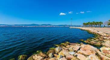 T&uuml;rkiye&rsquo;nin en gelişmiş sanayi şehirlerinden biri olan Kocaeli; hem İzmit K&ouml;rfezi hem de Karadeniz kıyılarında uzanan tertemiz plajları, yemyeşil milli parkları ve kaliteli kayak merkezleriyle aynı zamanda Marmara B&ouml;lgesi&rsquo;nin en kendine &ouml;zg&uuml; turistik şehirlerinden biri. Kartepe Kayak Merkezi&rsquo;nde her yıl binlerce yerli ve yabancı turisti misafir eden şehir, Maşukiye&rsquo;nin alabalık &ccedil;iftlikleri, Kerpe ve Kefken&rsquo;in benzersiz kaya oluşumları, Kandıra&rsquo;nın Akdeniz&rsquo;i aratmayan sahilleriyle de yaz tatillerinin sevilen adreslerinden biri. B&uuml;y&uuml;k şehirlere yakınlığıyla da karşımıza &ccedil;ıkan Kocaeli'de gezilecek yerlere ge&ccedil;meden &ouml;nce bize en &ccedil;ok sorulan soruları yanıtlayarak işe koyuluyoruz. Kocaeli&rsquo;nde ne yenir? Kocaeli seyahatin sırasında mancarlı Kandıra pidesi, hindi dolması, dartı, ciğerli kavurma, uma&ccedil; ve kesme &ccedil;orbası ve Kandıra yoğurdunun mutlaka tadına bakmalısın. Pişmaniyenin de tadına bakmadan ise d&ouml;nmemelisin. Kocaeli hangi illere yakın? Doğu ve g&uuml;neydoğusunda Sakarya, g&uuml;neyinde Bursa, batısında Yalova ve İstanbul yakın olduğu iller arasında. Kocaeli- Sabiha G&ouml;k&ccedil;en havalimanı arası ka&ccedil; dakika? Kocaeli- Sabiha G&ouml;k&ccedil;en havalimanı arası 52 kilometre olup yaklaşık olarak 1 saat s&uuml;rer. 1. Başiskele Sahili İzmit K&ouml;rfezi&rsquo;nin en g&uuml;zel manzaralarını izlemek ve harika fotoğraflarını &ccedil;ekmeye hazır mısın? İnce kumlu plajı, sahil boyunca uzanan y&uuml;r&uuml;y&uuml;ş, koşu ve bisiklet yolları ile &ccedil;ok sevilen bir dinlenme alanı olan sahilde &ccedil;ocuklar i&ccedil;in eğlence merkezleri, parklar ve oyun alanları da bulunuyor. Yaz aylarında denizin tadını &ccedil;ıkarabileceğin ve serin deniz havasında akşam y&uuml;r&uuml;y&uuml;şlerine &ccedil;ıkabileceğin Başiskele sahili, gece aydınlatıldığında sunduğu &ccedil;arpıcı manzaralarıyla da g&ouml;r&uuml;lmeye değer. Konum Linki 2. Seka Park Sadece Kocaeli'nin değil, T&uuml;rkiye&rsquo;nin de en b&uuml;y&uuml;k şehir i&ccedil;i parklarından biri olan ve denize sıfır konumda inşa edilen Seka Park, eski Seka Kağıt Fabrikası arazisinde 580 d&ouml;n&uuml;ml&uuml;k bir yeşil alana yayılıyor. Etkileyici deniz manzaraları eşliğinde y&uuml;r&uuml;y&uuml;şlere &ccedil;ıkabileceğin parkurların yanı sıra kır bah&ccedil;eleri, kafeler, balık restoranları, mesire alanları ile ilgi &ccedil;eken devasa parkta &ccedil;ocuklar i&ccedil;in geniş oyun merkezleri, kaykay pisti, sergi salonları, sanat at&ouml;lyeleri, a&ccedil;ık ve kapalı spor sahaları gibi pek &ccedil;ok olanak bulunuyor. Konum Linki 3. Kocaeli Kent Ormanı Kalabalık ve g&uuml;r&uuml;lt&uuml;den uzaklaşıp doğada zaman ge&ccedil;irmek i&ccedil;in gidebileceğin en g&uuml;zel yerlerden biri olan Kocaeli Kent Ormanı, şehir merkezine sadece 17 kilometre uzaklıkta. 300 d&ouml;n&uuml;ml&uuml;k geniş bir yeşil alanı yayılan ve aynı zamanda Kocaeli&rsquo;nin en b&uuml;y&uuml;k yeşil alanlarından biri olan kent ormanı; &ccedil;am ve meşe ağa&ccedil;larıyla s&uuml;sl&uuml; y&uuml;r&uuml;y&uuml;ş parkurları, mesire alanları, tenis kortları, futbol sahaları ve panoramik fotoğraflar &ccedil;ekebileceğin seyir terasları ile g&ouml;r&uuml;lmeye değer g&uuml;zellikte. Konum Linki 4. Seka Kağıt M&uuml;zesi &Uuml;lkemizin en eski sanayi kuruluşlarından biri olan Seka Kağıt Fabrikasının belirli b&ouml;l&uuml;mleri d&uuml;zenlenerek 2016 yılında m&uuml;ze haline getirildi. 12.000 m2 alana yayılan ve etkileyici koleksiyonlarıyla ilgi g&ouml;ren Seka Kağıt M&uuml;zesinde kağıttan &uuml;retilmiş sanat eserleri, heykeller ve birbirinden ilgin&ccedil; &uuml;r&uuml;nler arasında keyifli bir gezi yapabilirsin. Cumhuriyet tarihi boyunca kağıt &uuml;retmek i&ccedil;in kullanılan makineleri ve kağıt &uuml;retim s&uuml;re&ccedil;lerini de yakından g&ouml;rebileceğin Seka Kağıt M&uuml;zesi, Avrupa'nın en b&uuml;y&uuml;k kağıt m&uuml;zesi ve T&uuml;rkiye'nin en b&uuml;y&uuml;k end&uuml;striyel miras m&uuml;zesi olarak g&ouml;r&uuml;lmeye değer. Konum Linki {calismasaatleri}Giriş &uuml;creti &Uuml;cretsiz A&ccedil;ık olduğu saatler Pazartesi g&uuml;nleri kapalı Diğer g&uuml;nler 09.00-17.30{/calismasaatleri} 5. Derince Harikalar Sahili Kocaeli merkezine sadece 14 kilometre uzaklıktaki Derince il&ccedil;esinin sahil şeridinin bir b&ouml;l&uuml;m&uuml;, 2007 yılında yeniden d&uuml;zenlenerek şehrin en b&uuml;y&uuml;k temalı parklarından biri haline getirildi. &Ccedil;ocuklu ailelerin kesinlikle uğramasını &ouml;nerdiğimiz Derince Harikalar Sahili; birbirinden g&uuml;zel mantar evler, masal ve &ccedil;izgi roman kahramanlarının heykelleri, &ccedil;ocuklar i&ccedil;in lunaparklar, devasa şatolar, gezi trenleri ve g&uuml;n boyu s&uuml;ren eğlenceli aktiviteleri ile &ccedil;ok pop&uuml;ler. Yetişkinlerin de b&uuml;y&uuml;leyici deniz manzaraları eşliğinde yorgunluk atabileceği kır bah&ccedil;eleri ve restoranların hizmet verdiği park, Denizciler Caddesi &uuml;zerinde yer alıyor. Konum Linki {insightBoxStart}Yazar Notu: Merkezden veya otogardan kalkan Derince minib&uuml;slerini kullanarak ulaşım sağlayabilirsin.{insightBoxEnd} 6. Selim Sırrı Paşa Konağı Mimari ve tarih meraklılarının Kocaeli gezisinde kesinlikle g&ouml;rmesini &ouml;nerdiğimiz başka bir etkileyici mimari yapı da 19. y&uuml;zyılda inşa edilen ve Osmanlı d&ouml;neminin en g&uuml;zel sivil mimari &ouml;rneklerinden biri olarak g&ouml;sterilen Sırrı Paşa Konağı. İzmit K&ouml;rfezine hakim bir konumda, 4 katlı olarak inşa edilen ve etkileyici ahşap s&uuml;slemelerle dikkat &ccedil;eken konak; haremlik ve selamlık b&ouml;l&uuml;mleri, bitki motifleriyle s&uuml;sl&uuml; tavanı ve d&ouml;nem mobilyalarıyla dekore edilmiş odalarıyla seni tarihte bir yolculuğa &ccedil;ıkaracak. Kocaeli&rsquo;nin en g&ouml;rkemli ve etkileyici yapılarından olan Selim Sırrı Paşa Konağı, İzmit il&ccedil;esinde Sırrıpaşa Caddesi &uuml;zerinde kısa bir y&uuml;r&uuml;y&uuml;şle ulaşılabilecek g&uuml;zel bir konumda yer alıyor. Konum Linki {calismasaatleri}Giriş &uuml;creti &Uuml;cretsiz A&ccedil;ık olduğu saatler Haftanın her g&uuml;n&uuml; 09.00-17.30{/calismasaatleri} {insightBoxStart}Yazar Notu: Her yarım saatte bir rehber turu başlıyor.{insightBoxEnd} 7. Gayret Gemi M&uuml;zesi Kore ile Vietnam savaşlarında g&ouml;rev alan ve 1972 yılından beri T&uuml;rk Deniz Kuvvetleri&rsquo;ne hizmet veren Gayret Gemisi, &uuml;lkemizin &ouml;nemli tersanelerinde G&ouml;lc&uuml;k Tersanesi&rsquo;nde i&ccedil; b&ouml;l&uuml;mleri yenilenerek halkın ziyaretine a&ccedil;ıldı. Savaş komuta merkezi ile komutanların kamaralarının yanı sıra geminin mutfak, yatakhane, &ccedil;amaşırhane b&ouml;l&uuml;mlerini de gezebilir ve ilgin&ccedil; fotoğraflar &ccedil;ekebilirsin. T&uuml;rkiye'nin ilk m&uuml;ze gemisi olarak ayrı bir &ouml;nemi de sahip. Konum Linki {calismasaatleri}Giriş &uuml;creti 0-6 yaş &uuml;cretsiz 90 TL A&ccedil;ık olduğu saatler Haftanın her g&uuml;n&uuml; 09.00-17.30{/calismasaatleri} {insightBoxStart}Yazar Notu: Kapıda beklememek i&ccedil;in &ouml;nceden rezervasyon yaptırabilirsin.{insightBoxEnd} 8. U&ccedil;urtma Tepesi İzmit K&ouml;rfezi'ne hakim y&uuml;ksek bir tepede uzanan U&ccedil;urtma Tepesi, hem keyifli bir gezi yapabileceğin hem de &ccedil;ocuklarınla eğlenebileceğin sevilen yerler arasında. &Ouml;zellikle hafta sonları &ccedil;ocuklarıyla u&ccedil;urtma u&ccedil;urmak isteyen ailelerle dolan tepede İzmit K&ouml;rfezi&rsquo;nin panoramik fotoğraflarını &ccedil;ekebileceğin seyir terasları, y&uuml;r&uuml;y&uuml;ş yolları, peyzajlı &ccedil;i&ccedil;ek bah&ccedil;eleri ve &ccedil;ocuk parkları gibi pek &ccedil;ok imkan bulunuyor. Konum Linki 9. İzmit Saat Kulesi Kocaeli'nin simgesel yapılarından biri olan ve halk arasında Kocaeli Saat Kulesi olarak da bilinen 16 metre y&uuml;kseklikteki 4 katlı İzmit Saat Kulesi, 1902 yılında Padişah II. Abd&uuml;lhamit&rsquo;in anısına inşa edilmiş etkileyici bir mimari şaheser. Şehrin her yerinden g&ouml;r&uuml;necek şekilde &ouml;zel bir konuma yerleştirilen ve &ccedil;arpıcı neoklasik mimarisiyle Kocaeli&rsquo;nin en &ccedil;ok fotoğraflanan yapılarından biri olan saat kulesi, 2010 yılında aslına uygun olarak restore edildi. &Ccedil;evresindeki kafeler, restoranlar, hediyelik eşya d&uuml;kkanları, y&uuml;r&uuml;y&uuml;ş yolları ve &ccedil;ocuk oyun alanlarıyla sevilen bir gezi alanı da olan İzmit Saat Kulesi&rsquo;ne kısa bir y&uuml;r&uuml;y&uuml;şle kolayca ulaşım sağlayabilirsin. Konum Linki 10. Kocaeli Bilim Merkezi Şehri gezen &ccedil;ocuklu ailelerin kesinlikle uğramasını &ouml;nerdiğimiz Kocaeli Bilim Merkezi, Kocaeli B&uuml;y&uuml;kşehir Belediyesi ve T&Uuml;BİTAK'ın katkılarıyla 2015 yılında hizmete a&ccedil;ıldı. Her yaştan &ccedil;ocuğa bilim ile teknolojiyi eğlenceli bir şekilde anlatmayı ama&ccedil;layan ve 8.500 metrekarelik geniş bir alana yayılan bilim merkezinin i&ccedil;erisinde 250'den fazla deney alanı, sergi salonları, k&uuml;t&uuml;phaneler ve ilgin&ccedil; at&ouml;lyeler bulunuyor. 1934 yılında a&ccedil;ılan ve &uuml;lkemizin en eski sanayi kuruluşlarından biri olan Seka Kağıt Fabrikasının alanında yer alan Kocaeli Bilim Merkezi&rsquo;nde yılın her d&ouml;nemi d&uuml;zenlenen konferanslar, eğitimler, workshoplar ve bilim g&ouml;sterilerine de katılabilirsin. Konum Linki {calismasaatleri}Giriş &uuml;creti &Uuml;cretsiz A&ccedil;ık olduğu saatler Haftanın her g&uuml;n&uuml; 09.00-17.30{/calismasaatleri} {{campaignsSlider}} 11. Kocaeli Arkeoloji ve Etnografya M&uuml;zesi Uzun bir tarihe sahip olarak pek &ccedil;ok medeniyetten izler taşıyan Kocaeli'nin tarihi ve k&uuml;lt&uuml;rel hazineleri g&ouml;rmek i&ccedil;in Kocaeli Arkeoloji ve Etnografya M&uuml;zesi'ne uğrayabilirsin. İzmit'in tarihi tren garının restore edilmesiyle ziyarete a&ccedil;ılan m&uuml;zenin koleksiyonlarında Kaba Taş Devrinden Helenistik, Roma Bizans ve Osmanlı d&ouml;nemine kadar uzanan binlerce eseri yakından g&ouml;rebilirsin. 21 d&ouml;n&uuml;m gibi geniş bir alana yayılan m&uuml;zenin bah&ccedil;esinde ise Roma d&ouml;nemine ait lahitler, taş ve mermer heykeller bulunuyor. Konum Linki {calismasaatleri}Giriş &uuml;creti M&uuml;zeKart ge&ccedil;erli Tam 60 TL &Ouml;ğrenci 30 TL A&ccedil;ık olduğu saatler Pazartesi g&uuml;nleri kapalı Diğer g&uuml;nler 09.00-17.30{/calismasaatleri} {insightBoxStart}Yazar Notu: Navigasyon yanlış yere &ccedil;ıkarabiliyor. Harita ile gitmeni &ouml;neriyoruz.{insightBoxEnd} 12. Atat&uuml;rk, Redif ve Etnografya M&uuml;zesi 1800'l&uuml; yılların sonlarında inşa edilen etkileyici bir konakta hizmet veren Atat&uuml;rk, Redif ve Etnografya M&uuml;zesi, Kocaeli'nin en &ccedil;ok ziyaret edilen m&uuml;zelerinden biri. Osmanlı redif subayları i&ccedil;in inşa edilen ve ismini de buradan alan m&uuml;zede 18. ve 19. y&uuml;zyıl d&ouml;nem mobilyaları, askeri malzemeler, &uuml;niformalar, madalyalar, tarihi belgeler ve savaş fotoğrafları gibi pek &ccedil;ok obje sergileniyor. Konum Linki {calismasaatleri}Giriş &uuml;creti M&uuml;zeKart ge&ccedil;erli 60 TL A&ccedil;ık olduğu saatler Pazartesi g&uuml;nleri kapalı Diğer g&uuml;nler 09.00-17.30{/calismasaatleri} 13. Doğu Kışla Gen&ccedil;lik Parkı Spor yapmak isteyenlerin Kocaeli&rsquo;nde en sık uğradığı yerlerden biri olan Doğu Kışla Gen&ccedil;lik Parkı; &ccedil;im halı sahaları, spor salonları, tenis kortları, y&uuml;r&uuml;y&uuml;ş ve koşu yolları ile spor yapmak i&ccedil;in ilk uğraman gereken yerler arasında. &Ccedil;ocuklar ve gen&ccedil;ler i&ccedil;in spor eğitimlerinin de verildiği gen&ccedil;lik parkı, &ouml;zellikle sabahları ve hafta sonları temiz havada spor yapmak isteyen insanlarla doluyor. Konum Linki 14. Ormanya Doğal Yaşam Parkı Hem &ccedil;ocuklu ailelerin hem de doğa severlerin Kocaeli&rsquo;nde mutlaka uğradığı yerlerden biri olan Ormanya Doğal Yaşam Parkı; 189 hektarlık orman alanı, benzersiz mantar evleri, donanımlı kamp ve karavan alanlarıyla dinlendirici bir g&uuml;n sunuyor. Binlerce hayvan t&uuml;r&uuml;ne ev sahipliği yapan alanda &ccedil;ocukların &ccedil;ok sevdiği deve kuşları, ceylanlar, midilli atlar ve karacaların harika fotoğraflarını &ccedil;ekebilirsin. Organik &uuml;r&uuml;nlerle hazırlanan kahvaltılar ve y&ouml;resel lezzetler sunan restoranları, temiz havada dinlenebileceğin kır bah&ccedil;eleri, &ccedil;ocuk oyun parkları, orman boyunca uzanan y&uuml;r&uuml;y&uuml;ş ve bisiklet parkurları ile hem eğlenceli hem de huzurlu bir g&uuml;n ge&ccedil;irebileceğin Ormanya Doğal Yaşam Parkı mutlaka g&ouml;rmen gereken yerler arasında. Konum Linki {calismasaatleri}Giriş &uuml;creti &Uuml;cretsiz Otopark 50 TL{/calismasaatleri} {insightBoxStart}Yazar Notu: Hafta sonu ve &ouml;zel g&uuml;nlerde &ccedil;ok kalabalık olabiliyor. Keyif almak ve g&uuml;zel zaman ge&ccedil;irmek i&ccedil;in hafta i&ccedil;ini tercih etmelisin.{insightBoxEnd}&nbsp; 15. Kartepe Kayak Merkezi Sadece Kocaeli&rsquo;nin değil, İstanbul ve Bursa gibi komşu şehirlerin de en sevilen kış tatili merkezlerinden biri olan Kartepe Kayak Merkezi, şehre sadece 32 kilometre uzaklıkta. Kartepe Dağı eteklerinde deniz seviyesinden yaklaşık 1600 metre y&uuml;kseklikte kurulan kayak merkezi; d&uuml;nya standartlarındaki pistleri, kayak ekipmanları kiralayabileceğin tesisleri, d&uuml;nya mutfaklarından lezzetler sunan restoranları ve kaliteli otelleriyle her kış binlerce insanı ağırlıyor. Her yaş grubu i&ccedil;in kayak ve snowboard eğitimleri alabileceğin Kartepe Kayak Merkezi&rsquo;nde &ccedil;ocuklara &ouml;zel pistler ve geniş oyun alanları da bulunuyor. G&uuml;zel bir kayak tatili i&ccedil;in Kartepe kayak merkezi rehberi yazısına mutlaka g&ouml;z atmalısın. Konum Linki 16. Ballıkayalar Kanyonu ve Tabiat Parkı Sadece Kocaeli'nde değil, Marmara B&ouml;lgesi'nde d&uuml;zenlenen doğa gezileri ve fotoğraf safarilerinin en sevilen adreslerinden biri olan Ballıkayalar Kanyonunun &ccedil;evresi 1995 yılında milli parkı ilan edilerek koruma altına alındı. 500'e yakın vahşi hayvan t&uuml;r&uuml; ve y&uuml;zlerce kuş t&uuml;r&uuml;ne ev sahipliği yapan Ballıkayalar Kanyonu ve Tabiat Parkı, 850 hektarlık geniş bir alana yayılıyor. 1,5 kilometre boyunca uzanan devasa sarp kaya duvarları ve zengin bitki &ccedil;eşitliliği ile T&uuml;rkiye'nin en g&uuml;zel y&uuml;r&uuml;y&uuml;ş parkurlarından biri olarak g&ouml;sterilen kanyon, her zorluk derecesine g&ouml;re d&uuml;zenlenmiş parkurları ile profesyonel y&uuml;r&uuml;y&uuml;şleri de yılın her mevsimi kendine &ccedil;ekiyor. Konum Linki {calismasaatleri}Giriş &uuml;creti Ara&ccedil; başı 150 TL{/calismasaatleri} {insightBoxStart}Yazar Notu: Kanyon i&ccedil;erisinde bulunan bazı parkur zeminleri kaygan olabiliyor. Ayağına kaydırmayan outdoor ayakkabı giymeni &ouml;neriyoruz.{insightBoxEnd}&nbsp; 17. Kumcağız Plajı Kocaeli merkezine yaklaşık 1 saat uzaklıktaki Kandıra il&ccedil;esinde yer alan Kumcağız Plajı, yaz aylarında Karadeniz'in serin ve tertemiz suların tadını &ccedil;ıkarmak i&ccedil;in gidebileceğiniz en g&uuml;zel plajlardan. Huzurlu tatil arayanların sık&ccedil;a ziyaret ettiği Kerpe ile Kefken arasında uzanan plaj, berrak denizi ve altın renkli kumlarla s&uuml;sl&uuml; sahiliyle &ccedil;ok seviliyor. Turizm olanakları bakımından da gelişmiş olan Kumcağız Plajı&rsquo;nın &ccedil;evresinde her b&uuml;t&ccedil;eye uygun apart oteller, butik oteller ve pansiyonlar hizmet veriyor. Balık ge&ccedil;iş noktasında yer alan plaj, hem olta balık&ccedil;ılığı yapmak hem de teknelerle balık avlama turlarına &ccedil;ıkmak i&ccedil;in de ideal noktalar arasında. Kocaeli'nde her saat bulabileceğiniz Kandıra minib&uuml;sleriyle kolayca gidebileceğiniz Kumcağız Plajında dinlendirici bir deniz g&uuml;n&uuml; ge&ccedil;irebilir, plajın arkasını saran &ccedil;am ormanlarında ise kamp yapabilirsiniz. Konum Linki {calismasaatleri}Giriş &uuml;creti 2 şezlong + 1 şemsiye 200TL{/calismasaatleri} {insightBoxStart}Yazar Notu: Plaj alanı &ccedil;evresinde herhangi bir ATM bulunmuyor.{insightBoxEnd}&nbsp; 18. Kerpe Kartal Kayaları Milyonlarca yılda sert dalgalar ve r&uuml;zg&acirc;rlarla şekillenmiş birbirinden ilgin&ccedil; kayalarıyla t&uuml;m d&uuml;nyadan fotoğraf&ccedil;ıların ilgisini &ccedil;eken Kerpe Kartal Kayalar, Kocaeli seyahatin sırasında mutlaka g&ouml;rmen gereken yerler arasında. Kartalı andırmasından ismini alan Kerpe Kartal Kayaları ise b&ouml;lgede en &ccedil;ok fotoğraflanan kaya oluşumları arasında. &Ouml;zellikle kızıl g&uuml;n doğumu ve g&uuml;n batımlarında inanılmaz manzaralara şahit olabileceğin devasa kayaların g&ouml;letlerinin tertemiz sularında da unutulmaz bir y&uuml;zme deneyimi yaşayabilirsin. Doğa gezileri ve fotoğraf&ccedil;ılık turlarının yanı sıra tekne gezileriyle de Kerpe Kartal Kayalarına uğrayabilir ve gezinizin en g&uuml;zel fotoğraflarını burada &ccedil;ekebilirsin. Konum Linki {insightBoxStart}Yazar Notu: Kocaeli&rsquo;nde sık aralıklarla bulabileceğin minib&uuml;slerle 1 saat i&ccedil;erisinde buraya ulaşabilirsin.{insightBoxEnd}&nbsp; 19. Sardala Koyu Kocaeli'nde g&ouml;rmen gereken tabiat harikalarından biri olan ve gizli cennet olarak adlandırılan Sardala Koyu; binlerce yılda r&uuml;zg&acirc;r ve dalgalarla şekillenmiş etkileyici kaya oluşumları, kristal berraklığındaki denizi ve el değmemiş yemyeşil doğasıyla dinlendirici bir g&uuml;n ge&ccedil;irmek i&ccedil;in ilk uğraman gereken yerlerden. Sadece T&uuml;rkiye'den değil t&uuml;m d&uuml;nyadan doğalseverlerin ve kamp&ccedil;ıların ilgisini &ccedil;eken bakir koy, arkası &ccedil;am ormanları &ouml;n&uuml; ise turkuaz denizle &ccedil;evrili ince kumlu sahili ile Ege ve Akdeniz&rsquo;i aratmıyor. Konum Linki 20. Beşkayalar Tabiat Parkı Kocaeli'nde keşfe &ccedil;ıkabileceğin başka bir sevilen gezi alanı olan Beşkayalar Tabiat Parkı, şehir merkezinde yaklaşık 27 kilometre uzaklıkta. Devasa Kanyon duvarları, metrelerce y&uuml;kseklikten d&ouml;k&uuml;len şelaleleri ve irili ufaklı dereleri ile &ccedil;am ormanları arasında dinlendirici bir g&uuml;n yaşayabileceğin tabiat parkında binlerce yıllık mağaraları da rehberlerle birlikte keşfe &ccedil;ıkabilirsin. Donanımlı kamp alanları ve iyi işaretlenmiş y&uuml;r&uuml;y&uuml;ş yollarıyla yılın her mevsimi ilgi g&ouml;ren Beşkayalar Tabiat Parkı; Bursa İstanbul ve Ankara gibi b&uuml;y&uuml;k şehirlere yakın olduğu i&ccedil;in b&ouml;lgenin &ouml;nemli doğa sporu merkezlerinden. Konum Linki 21. Cebeci Plajı ve Sahili Mavinin her tonunu g&ouml;rebileceğin, b&uuml;y&uuml;leyici Karadeniz manzaraları eşliğinde keyifli y&uuml;r&uuml;y&uuml;şler yapmak ve yaz aylarında denizin tadını &ccedil;ıkarmak i&ccedil;in gidebileceğin en pop&uuml;ler yerlerden biri de Cebeci sahili. Altın renkli kumlarıyla &uuml;nl&uuml; mavi bayraklı Cebeci Plajına da ev sahipliği yapan sahilin &ccedil;evresinde her b&uuml;t&ccedil;eye uygun apart ve butik oteller yer alıyor. Her yıl binlerce kişi tarafından ziyaret edilen Cebeci sahilinde akşam y&uuml;r&uuml;y&uuml;şlerine &ccedil;ıkabilir, balık restoranlarında mevsimlik Karadeniz balıkları ve y&ouml;resel mezeler tadabilirsin. Cebeci, aynı zamanda İstanbul'a en yakın mavi bayraklı plaja sahip olmasından dolayı da b&uuml;y&uuml;k şehirlerden en &ccedil;ok ziyaret edilen Kocaeli&rsquo;nin turistik noktaları arasında. Konum Linki 22. Kuzuyaylası Tabiat Parkı Kocaeli'nde doğa y&uuml;r&uuml;y&uuml;şleri ve yayla turlarının &ouml;nemli merkezlerinden biri olan Kuzu Yaylası&rsquo;nın &ccedil;evresi, el değmemiş g&uuml;zelliklerin korunması i&ccedil;in 2011 yılında milli park ilan edildi. Şehrin en pop&uuml;ler doğaya ka&ccedil;ış noktalarından biri olan ve Maşukiye sınırlarında yer alan Kuzuyayla Tabiat Parkı; Sapanca G&ouml;l&uuml; manzaralı y&uuml;r&uuml;y&uuml;ş yolları, oksijen seviyesi y&uuml;ksek temiz havası, mesire alanları, seyir terasları ve kır lokantalarıyla yılın yorgunluğunu atmak i&ccedil;in ilk uğraman gereken yerlerden. Kış aylarında kar manzaraları eşliğinde de geziler yapabileceğin Kuzuyaylası Tabiat Parkı&rsquo;nda ahşap yayla evleri ve orman k&ouml;şklerinde konaklayabilir veya &ccedil;adırını kurarak doğa i&ccedil;erisinde dinlenebilirsin. Kamp yapmak i&ccedil;in &ccedil;ok tercih edilen Kuzuyayla Tabiat Parkı i&ccedil;erisinde tuvalet ve mescit bulunuyor. G&uuml;venliğin son derece y&uuml;ksek olduğu alanda herhangi bir market bulunmadığı i&ccedil;in t&uuml;m istek ve ihtiya&ccedil;larını yanına almanda fayda var. Konum Linki {calismasaatleri}Giriş &uuml;creti Ara&ccedil; 90 TL{/calismasaatleri} {insightBoxStart}Yazar Notu: Ateş yakmak yasak.{insightBoxEnd}&nbsp;&nbsp; 23. Seyrek Plajı Turistik tatil beldesi Kandıra'nın başka bir sevilen plajı olan Seyrek Plajı 400 metre uzunluğunda ince kumlu sahili ve harika manzaraları ile hem b&ouml;lge halkı hem de &ccedil;evre illerden gelenler tarafından &ccedil;ok seviliyor. Balık ge&ccedil;iş noktasında yer aldığı i&ccedil;in dalışlar yaparak onlarca balık t&uuml;r&uuml;n&uuml; yakından g&ouml;rebileceğin plajda k&uuml;&ccedil;&uuml;k balık&ccedil;ı kayıklarıyla d&uuml;zenlenen balık avlama etkinliklerine katılarak da farklı deneyimler yaşayabilirsin. Az sayıda işletme ve turistik tesisin bulunduğu plajda mevsimlik balıklar tadabileceğin deniz manzaralı balık restoranları da &ccedil;ok ilgi g&ouml;r&uuml;yor. Konum Linki 24. Serindere Kanyonu Kocaeli'nin turistik il&ccedil;esi Kartepe sınırlarında uzanan ve doğa sporları yapmak i&ccedil;in en sevilen adreslerinden olan Serindere Kanyonu, hem doğaseverler hem de kamp&ccedil;ıların keşfetmesi gereken tabiat harikalarından. Birbirinden g&uuml;zel şelaleleri, buz gibi dereleri ve onlarca ağa&ccedil; &ccedil;eşidiyle s&uuml;sl&uuml; doğasıyla &uuml;nl&uuml; Serindere Kanyonu, aynı zamanda Marmara B&ouml;lgesindeki en zorlu y&uuml;r&uuml;y&uuml;ş parkurlarına da ev sahipliği yapıyor. Bahar ve yaz aylarında kar sularının erimesiyle buz gibi olan şelale g&ouml;letlerinde serinleyebileceğini ve y&uuml;zlerce metrelik devasa kanyon duvarları arasında rehberli y&uuml;r&uuml;y&uuml;şlere katılabileceğin Serindere Kanyonu; dağ bisikleti gezileri, ATV turları, kamp&ccedil;ılık, kaya tırmanma ve dağcılık gibi onlarca etkinlik i&ccedil;in ideal. Konum Linki 25. Ayrı Gezegen Cam Terası Kocaeli&rsquo;nin oksijen deposu Kartepe&rsquo;nin eteklerinde uzanan Ayrı Gezegen Cam Terası, Kocaeli&rsquo;de mutlaka uğraman gereken yerler arasında. 2019 yılında hizmete a&ccedil;ıldığından beri binlerce yerli ve yabancı turist tarafından ziyaret edilen, 185 metre y&uuml;ksekliğindeki Ayrı Gezegen Cam Terasında Sapanca G&ouml;l&uuml; ve Saman Dağlarına kadar uzanan benzersiz doğa manzaralarına şahit olacaksın. Manzarayı tamamlayan akarsuların &ccedil;evresindeki kır bah&ccedil;elerinde ve balık &ccedil;iftliklerinde dinlenebileceğin gezinde macera parkı ve &ccedil;ocuk oyun alanlarında da g&uuml;zel zaman ge&ccedil;irebilirsin. Konum Linki {calismasaatleri}Giriş &uuml;creti 150 TL A&ccedil;ık olduğu saatler Haftanın her g&uuml;n&uuml; 09.00-22.00{/calismasaatleri} {insightBoxStart}Yazar Notu: Tuvalet i&ccedil;in yanında nakit para bulundurmalısın. Restoranın fiyatları biraz y&uuml;ksek, oturmadan &ouml;nce fiyatlara g&ouml;z atmanda fayda var.{insightBoxEnd}&nbsp;&nbsp; 26. Kandıra Kocaeli merkezine yaklaşık 45 kilometre uzaklıktaki Kandıra il&ccedil;esi, tarihi yapıları ve doğal g&uuml;zellikleri ile g&uuml;n&uuml;birlik gezilere &ccedil;ıkmak i&ccedil;in en ideal yerlerden. Kristal berraklığındaki denizi, birbirinden g&uuml;zel plajları, milyonlarca yılda oluşmuş etkileyici kaya oluşumları ile ilgi g&ouml;ren Kandıra sahili, el değmemiş g&uuml;zellikleri ile &uuml;nl&uuml; Sardala Koyu gibi bir&ccedil;ok gizli koya da ev sahipliği yapıyor. Kocaeli&rsquo;nin sevilen tatil cennetlerinden Kerpe, tekne gezilerinin değişmez adreslerinden Kefken Adası, t&uuml;m d&uuml;nyadan fotoğrafları kendine &ccedil;eken Pembe Kayalar, Karadeniz'in en g&uuml;zel plajlarından biri olarak g&ouml;sterilen Cebeci Plajı, T&uuml;rkiye'nin en b&uuml;y&uuml;k 6. g&ouml;leti olan Tahtalı G&ouml;leti, doğal atmosferini korumayı başarmış Bağırganlı K&ouml;y&uuml; ve Babalı K&ouml;y&uuml; gibi pek &ccedil;ok gezi alanı bulabileceğin Kandıra&rsquo;da hem denizin hem de doğanın tadını &ccedil;ıkarabilirsin. Konum Linki {insightBoxStart}Yazar Notu: Kocaeli Otogarında sık aralıklarla bulabileceğin minib&uuml;slerle yaklaşık 45 dakikada ulaşabilirsin.{insightBoxEnd}&nbsp;&nbsp; 27. Bayramoğlu Adası Kocaeli'nin en batı ucunda Darıca il&ccedil;esi sınırlarında yer alan Bayramoğlu Adası, tertemiz plajı ve yaz aylarında bile sakin kalan uzun sahiliyle &ccedil;ok sevilen bir tatil cenneti. Temiz sularında doyasıya y&uuml;zebileceğin ve şnorkelli dalışlar yapabileceğin ada da g&uuml;n&uuml;birlik ve saatlik tekne turlarıyla İzmit K&ouml;rfezi koylarını keşfe &ccedil;ıkabilirsin. Bayramoğlu Adasında apart oteller, butik oteller, pansiyonlar, balık restoranları ve kafeler gibi pek &ccedil;ok imkan da bulunuyor. Konum Linki 28. Kandıra Sarısu Plajı Kocaeli'nde denize girebileceğin en sevilen plajlardan biri de Kandıra il&ccedil;esi sınırlarında yer alan Sarısu Plajı. Kandıra&rsquo;ya sadece 8 kilometre uzaklıkta yer alan ve &ouml;zellikle &ccedil;evresini saran donanımlı kamp alanları ile b&ouml;lgenin en sevilen kamp merkezlerinden biri haline gelen Sarısu Plajı; tertemiz denizi, sessiz ve huzurlu atmosferiyle keyifli bir deniz g&uuml;n&uuml; sunuyor. Yaz aylarında bile olduk&ccedil;a sakin olan plaj, kalabalıklardan uzakta denize girmek isteyen aileler i&ccedil;in de ideal. Konum Linki {insightBoxStart}Yazar Notu: Kocaeli Otogarından sık aralıklarla bulabileceğin Kandıra minib&uuml;sleriyle kolaylıkla ulaşım sağlayabilirsin.{insightBoxEnd}&nbsp; &nbsp; 29. Bağırganlı Koyu Hem doğa y&uuml;r&uuml;y&uuml;şlerine &ccedil;ıkmak hem de denizin tadını &ccedil;ıkarmak ve kamp yapmak i&ccedil;in ziyaret edebileceğin Bağırganlı Koyu, Kandıra il&ccedil;esi sınırlarında yer alıyor. &Ccedil;evresi b&uuml;y&uuml;leyici kaya oluşumları ile s&uuml;sl&uuml; olan ve bakir doğal g&uuml;zelliğinden dolayı sit alanı olarak koruma altına alınan yemyeşil koy, Karadeniz&rsquo;in en g&uuml;zel koylarından biri olarak g&ouml;steriliyor. Hi&ccedil;bir yapılaşma bulunmayan Bağırganlı Koyu&rsquo;nun kristal berraklığındaki denizinde şnorkel dalışlar yaparak b&uuml;y&uuml;leyici su altı g&uuml;zelliklerine de şahit olabilirsin. Konum Linki 30. Pişman &Ccedil;ocuk Aquapark Yaz aylarında &ccedil;ocuklarınla eğlenceli zaman ge&ccedil;irebileceğin pop&uuml;ler tesislerden biri de İzmit il&ccedil;esinde yer alan Pişman &Ccedil;ocuk Aquapark. Şehre hakim y&uuml;ksek bir noktada konumlanan ve yılın 12 ayı kapalı havuzda &ccedil;ocuklar i&ccedil;in y&uuml;zme eğitimleri verilen su parkında hem yetişkinler hem de &ccedil;ocuklar i&ccedil;in kaydıraklar, a&ccedil;ık ve kapalı y&uuml;zme havuzları, &ccedil;ocuk oyun alanları, kafeteryalar ve g&uuml;neşlenme terasları gibi pek &ccedil;ok olanak bulunuyor. Konum Linki {calismasaatleri}Giriş &uuml;creti 0-3 yaş &uuml;cretsiz 4 yaş &uuml;st&uuml; &ccedil;ocuk hafta i&ccedil;i 250 TL 4 yaş &uuml;st&uuml; &ccedil;ocuk hafta sonu 300 TL A&ccedil;ık olduğu saatler Haftanın her g&uuml;n&uuml; 11.00-17.00{/calismasaatleri}&nbsp; 31. Kapri Koyu Karadeniz kıyısında sıralanan birbirinden g&uuml;zel koylarıyla b&ouml;lgenin en &ouml;nemli tatil cennetlerinden biri olan Kocaeli&rsquo;nde Ağva ile Cebeci arasında yer alan Kapri Koyu, turizm olanakları bakımından en gelişmiş koylardan biri olarak ilgi g&ouml;r&uuml;yor. Masmavi denizi ile &uuml;nl&uuml; koy, aynı zamanda kızıl g&uuml;n batımı eşliğinde romantik akşam yemekleri tadabileceğin restoranlarıyla da &ccedil;ok seviliyor. Her b&uuml;t&ccedil;eye uygun butik oteller, apart oteller ve pansiyonların hizmet verdiği Kapri Koyu&rsquo;na tekne gezilerinin yanı sıra Kefken minib&uuml;sleriyle de kısa s&uuml;rede ulaşabilirsin. Konum Linki {insightBoxStart}İpucu: Otob&uuml;s biletini ENUYGUN'dan kolayca alabileceğini unutma! Otob&uuml;s biletinde değişiklik ve iptal işlemlerini tek tıkla yapabilir, farklı firma ve seferleri karşılaştırabilirsin. Yola &ccedil;ıkmaya hazırsan Kocaeli otob&uuml;s bileti almak i&ccedil;in tıkla!{insightBoxEnd} {bus_search_form_banner} 32. Uzunkum Tabiat Parkı T&uuml;rkiye'nin en kuzeybatı ucunda yer alan 80 hektar b&uuml;y&uuml;kl&uuml;ğ&uuml;ndeki Uzunkum Tabiat Parkı, el değmemiş doğal g&uuml;zelliklerinden dolayı 2014 yılında koruma altına alındı. Karadeniz kıyısında kilometrelerce uzanan sahilinde kalabalıktan uzakta denizin tadını &ccedil;ıkarmak isteyen aileler tarafından da sık&ccedil;a ziyaret edilen park, onlarca &ccedil;eşit bitki &ccedil;eşidi ve vahşi yaşam zenginliğiyle doğa safarilerinin de ana merkezlerinden biri konumunda. Konum Linki 33. Samanlı Dağları Doğa severler i&ccedil;in adeta bir cennet olan Kocaeli'nde keşfe &ccedil;ıkabileceğin başka bir yeşil alan da Samanlı Dağları. İzmit K&ouml;rfezi, İznik G&ouml;l&uuml; ve Gemlik K&ouml;rfezi arasında uzanan Samanlı Dağları, 1699 metre y&uuml;kseklikteki Kartepe&rsquo;yi de i&ccedil;ine alan olduk&ccedil;a b&uuml;y&uuml;k bir alana yayılıyor. İlkbahar ve sonbahar aylarında sarıdan yeşile doğanın her tonunu g&ouml;rebileceğin b&uuml;y&uuml;leyici manzaralarından dolayı d&uuml;nyanın her yerinden doğa fotoğraf&ccedil;ılarının ilgisini &ccedil;eken Samanlı Dağları&rsquo;nda kış aylarında da kartpostal g&uuml;zelliğindeki kar manzaraları arasında keyifli bir gezi yapabilirsin. Konum Linki 34. Yeni Cuma Camii (Pertev Mehmet Paşa Camii ve K&uuml;lliyesi) Kocaeli'nde gezebileceğin Osmanlı d&ouml;neminden kalan etkileyici yapılarından biri de 1579 yılında inşa edilen Pertev Mehmet Paşa Camii ve K&uuml;lliyesi. Halk arasında Yeni Cuma Camii olarak da bilinen ve ismini II. Selim'in veziri Pertev Mehmet Paşa&rsquo;dan alan k&uuml;lliyenin i&ccedil;erisinde s&uuml;byan mektebi, şifahane, cami, hamam ve &ccedil;eşme gibi farklı b&ouml;l&uuml;mler bulunuyor. Mimar Sinan'ın etkileyici eserlerinden biri olmasıyla dikkat &ccedil;eken ve klasik Osmanlı mimarisine sahip olan g&ouml;rkemli Pertev Mehmet Paşa Camii ve K&uuml;lliyesi, g&ouml;r&uuml;lmeye değer Kocaeli yapılarından biri. Konum Linki 35. N&uuml;zhetiye Şelalesi Kocaeli'nin en &ouml;nemli trekking parkurlarından biri olan ve bakir doğal g&uuml;zelliğiyle hafta sonları ve yaz aylarının değişmez adreslerinden biri haline gelen N&uuml;zhetiye Şelalesi, Kocaeli merkezine yaklaşık 22 kilometre uzaklıkta yer alıyor. Sarp kayalar &uuml;st&uuml;nden d&ouml;k&uuml;len bembeyaz suları, buz gibi g&ouml;letleri, şelale &ccedil;evresinde hizmet veren kır bah&ccedil;eleri ve balık restoranlarıyla yaz sıcaklarında serinlemek i&ccedil;in de uğrayabileceğin N&uuml;zhetiye Şelalesi, her zorluk derecesine g&ouml;re d&uuml;zenlenmiş y&uuml;r&uuml;y&uuml;ş parkurlarıyla da yılın her d&ouml;nemi t&uuml;m &uuml;lkeden doğa y&uuml;r&uuml;y&uuml;ş&ccedil;&uuml;lerini misafir ediyor. Konum Linki 36. Hızır Reis Denizaltı M&uuml;zesi Sadece Kocaeli'nin değil, T&uuml;rkiye'nin de en ilgin&ccedil; etkileyici m&uuml;zelerinden biri olan ve 2. D&uuml;nya Savaşı D&ouml;neminden kalma bir denizaltıda hizmet veren Hızır Reis M&uuml;zesi, gezmeni &ouml;nerdiğimiz ilgin&ccedil; Kocaeli m&uuml;zelerinden biri. 30 yıldan uzun zaman ABD Deniz Kuvvetleri'nde yer alan ve sonrasında T&uuml;rk Deniz Kuvvetleri tarafından kullanılan denizaltı, 2004 yılından beri İzmit sahilinde m&uuml;ze olarak halka a&ccedil;ık. İsmini &uuml;nl&uuml; Osmanlı denizcisi Hızır Reis&rsquo;ten alan 95 metre uzunluğundaki denizaltının 80 kişilik m&uuml;rettebat odalarını, komuta b&ouml;l&uuml;mlerini, mutfağını, silah ve cephanelik b&ouml;l&uuml;mlerini inceleyebilirsin. Konum Linki {calismasaatleri}Giriş &uuml;creti 90 TL A&ccedil;ık olduğu saatler Haftanın her g&uuml;n&uuml; 09.00-16.00{/calismasaatleri}&nbsp; 37. İzmit Sahili Kocaeli'ni keşfetmeye başlamak i&ccedil;in en ideal noktalardan biri olan İzmit sahili, bir&ccedil;ok &ouml;nemli turistik tesise de ev sahipliği yapıyor. Deniz kenarı boyunca uzanan y&uuml;r&uuml;y&uuml;ş, bisiklet ve koşu yolları, peyzajlı &ccedil;i&ccedil;ek bah&ccedil;eleri, &ccedil;ocuk oyun alanları ve &ccedil;ardakları ile s&uuml;sl&uuml; sahile hem hafta sonları hem de yaz aylarında deniz havası almak veya spor yapmak isteyen y&uuml;zlerce insan uğruyor. İzmit sahili, aynı zamanda T&uuml;rkiye'nin b&uuml;y&uuml;k şehir parklarından biri olan Seka Park ve şehrin en ilgin&ccedil; m&uuml;zelerinden olan Hızır Reis Denizaltı M&uuml;zesi i&ccedil;in de sık&ccedil;a ziyaret ediliyor. &Ccedil;ay bah&ccedil;eleri, kafeler ve restoranlarla &ccedil;evrili İzmit sahilinde akşam y&uuml;r&uuml;y&uuml;şlerine &ccedil;ıkarak b&uuml;y&uuml;leyici g&uuml;n batımı manzaraları izlemeyi de unutma. Konum Linki 38. Eskihisar Kalesi Kocaeli gezisinde yakından g&ouml;rebileceğin &ouml;nemli bir tarihi hazinede İzmit K&ouml;rfezi&rsquo;nin g&uuml;ney b&ouml;l&uuml;m&uuml;n&uuml; kontrol etmek i&ccedil;in b&ouml;lgeye hakim bir tepeye 1241 yılında yapılan Eskihisar Kalesi. Bizans d&ouml;neminde inşa edilen ve Osmanlı d&ouml;neminde de genişletilerek kullanılmaya devam eden etkileyici kale, 1998 yılında aslına uygun olarak restore edilerek turizme kazandırıldı. Devasa g&ouml;zetleme kuleleri ve g&uuml;n&uuml;m&uuml;ze kadar ayakta kalmış surlarıyla b&uuml;y&uuml;leyici bir manzaraya sahip olan Eskihisar Kalesi&rsquo;nin hem i&ccedil; b&ouml;l&uuml;mlerini gezebilir hem de surlardan İzmit K&ouml;rfezi'nin en g&uuml;zel manzaralarının panoramik fotoğraflarını &ccedil;ekebilirsin. Konum Linki 39. Karam&uuml;rsel Sahili Eşsiz deniz manzaraları karşısında keyifli bir gezi yapabileceğin sevilen gezi alanı olan Karam&uuml;rsel Sahili, Kocaeli&rsquo;ne sadece 35 kilometre uzaklıkta. Yaz aylarında yerli ve yabancı turistlerle dolan sahil; ince kum plajı, kilometrelerce uzanan y&uuml;r&uuml;y&uuml;ş parkuru, bisiklet yolları ve k&uuml;&ccedil;&uuml;k yat limanıyla &ccedil;ok ilgi g&ouml;r&uuml;yor. Piknik yapmak isteyenler i&ccedil;in deniz manzaralı mesire alanları ve geniş &ccedil;ocuk oyun alanları da bulunan Karam&uuml;rsel Sahilinin &ccedil;evresinde ise oteller, restoranlar, kafeler ve eğlence merkezleri sıralanıyor. Konum Linki 40. Babalı Plajı Kocaeli&rsquo;nin tatil cenneti Kandıra'nın en g&uuml;zel sahil şeridine ev sahipliği yapan Babalı Plajı, Kocaeli'ne 70 kilometre, Kandıra&rsquo;ya ise sadece 30 kilometre uzaklıkta yer alıyor. Kilometrelerce uzanan altın kumlu sahilinde denizin tadını &ccedil;ıkarabileceğin plaj, aynı zamanda &ccedil;evresini saran &ccedil;arpıcı kaya oluşumları ile benzersiz fotoğraf&ccedil;ılar &ccedil;ekmek i&ccedil;in de sık&ccedil;a ziyaret ediliyor. Donanımlı kamp alanları ile Marmara'nın kamp yapmak i&ccedil;in en g&uuml;zel noktalarından biri olan Babalı Plajı ve &ccedil;evresini yılın her d&ouml;neminde d&uuml;zenlenen fotoğraf&ccedil;ılık gezileri, tekne turları ve bisiklet gezileri ile keşfe &ccedil;ıkılabilirsin. Konum Linki 41. Darıca Hobbit K&ouml;y&uuml; &Ccedil;ocuklu ailelerin Kocaeli'nde mutlaka uğramasını &ouml;nerdiğimiz ilgin&ccedil; yerlerden biri de Darıca il&ccedil;esi sınırlarında yer alan Hobbit K&ouml;y&uuml;. Doğayla uyumlu olarak tasarlanmış taş ve ahşap mimarili şirin Hobbit evlerinin s&uuml;slediği k&ouml;y, seni modern d&uuml;nyadan alıp fantastik bir d&uuml;nya yolculuğa &ccedil;ıkaracak. &Ccedil;ocukların &ccedil;ok eğlenceli zaman ge&ccedil;irebileceği Darıca Hobbit K&ouml;y&uuml;&rsquo;nde birbirinden g&uuml;zel fotoğraflar &ccedil;ekebilir, evlerin bah&ccedil;elerinde piknik yaparak keyifli zaman ge&ccedil;irebilirsin. T&uuml;rkiye'nin en b&uuml;y&uuml;k Hobbit k&ouml;y&uuml; olan ve İstanbul'a yakınlığından dolayı hafta sonları olduk&ccedil;a kalabalık olan Darıca Hobbit K&ouml;y&uuml;&rsquo;nde 4 kilometrelik bisiklet yolu, spor sahaları, y&uuml;r&uuml;y&uuml;ş parkurları, kır bah&ccedil;eleri ve &ccedil;ocuk oyun alanları gibi pek &ccedil;ok olanak bulunuyor. Konum Linki 42. Kavaklı Sahili Kocaeli merkezine sadece 16 kilometre uzaklıktaki G&ouml;lc&uuml;k il&ccedil;esi sınırlarında yer alan Kavaklı sahili, 81 d&ouml;n&uuml;ml&uuml;k arazi &uuml;zerinde inşa edilmiş &ccedil;ok sevilen bir dinlenme alanı. İ&ccedil;erisinde lunapark, &ccedil;ocuk oyun alanları, konserlerin d&uuml;zenlendiği etkinlik alanları, tenis kortları, basketbol ve voleybol sahaları bulunan sahil, &ouml;zellikle yaz akşamlarında serin havada y&uuml;r&uuml;y&uuml;şe &ccedil;ıkmak isteyen yerli ve yabancı turistlerle doluyor. Yıl boyu pek &ccedil;ok &ouml;nemli etkinlik, kutlama ve t&ouml;renin ger&ccedil;ekleştirildiği Kavaklı sahilinin koşu, y&uuml;r&uuml;y&uuml;ş ve bisiklet yollarında spor yaparak da keyifli bir g&uuml;n ge&ccedil;irebilirsin. Konum Linki 43. Değirmendere Sahili Kocaeli'nin G&ouml;lc&uuml;k il&ccedil;esi sınırlarında yer alan ve b&uuml;y&uuml;leyici deniz manzaraları eşliğinde y&uuml;r&uuml;y&uuml;şler yapmak i&ccedil;in mutlaka uğramanı &ouml;nerdiğimiz Değirmendere sahili, İzmit K&ouml;rfezi'nin incisi olarak kabul ediliyor. Huzurlu sahil kasabası; otelleri, balık&ccedil;ı restoranları, deniz kenarında sıralanan &ccedil;ay bah&ccedil;eleri, y&uuml;r&uuml;y&uuml;ş ve koşu yollarıyla g&uuml;n&uuml;birlik geziler yapmak i&ccedil;in en ideal yerler arasında. Yılın her d&ouml;nemi d&uuml;zenlenen balık avlama turlarına katılabileceğin veya asırlık &ccedil;ınar ağa&ccedil;larının g&ouml;lgesinde b&uuml;y&uuml;leyici deniz manzaraları eşliğinde mola verebileceğin Değirmendere Sahilinde huzurlu bir g&uuml;n ge&ccedil;irebilirsin. Konum Linki 44. Kumyalı Plajı Kocaeli'nde denizin ve g&uuml;neşin tadını &ccedil;ıkarmak i&ccedil;in gidebileceğin en g&uuml;zel plajlardan biri olan Kumyalı Plajı, şehir merkezine yaklaşık 30 kilometre uzaklıktaki Kordonboyu Caddesi &uuml;zerinde yer alıyor. 600 metre uzunluğundaki altın renkli kumlarla s&uuml;sl&uuml; sahili ve sanayi b&ouml;lgesine yakın olmasına rağmen tertemiz kalmış deniziyle Akdeniz sahillerini andıran Kumyalı Plajı, Marmara b&ouml;lgesindeki mavi bayrak &ouml;d&uuml;l&uuml; adayı iki plajdan biri. Yaz aylarında turistlerle dolan plajın sığ denizinde ve ince kumlu sahilinde &ccedil;ocuklu aileler de keyifli zaman ge&ccedil;irebilir. Konum Linki 45. Hannibal Anıt Mezarı Kocaeli'nde ziyaret edebileceğin başka bir ilgin&ccedil; yer de &uuml;nl&uuml; komutan Kartacalı Hannibal anısına 1981 yılında inşa edilen etkileyici taş anıt. 900 metrekarelik alanda 5 farklı b&ouml;l&uuml;mden oluşan anıt, T&Uuml;BİTAK arazisi i&ccedil;erisinde Hannibal Tepesi &uuml;zerinde y&uuml;kseliyor. Atat&uuml;rk'&uuml;n Hannibal&rsquo;ın b&ouml;lgede olduğu d&uuml;ş&uuml;n&uuml;len mezarının bulunması ve anıtının dikilmesi isteğinden dolayı 1981 yılında inşa edilen Hannibal Anıt Mezarı, antik d&uuml;nyanın en b&uuml;y&uuml;k komutanlarından biri olan Hannibal&rsquo;ın y&uuml;z&uuml;n&uuml;n kabartma tekniğiyle oyulduğu kayaları ve komutanın hayat hikayesini anlatan kitabesi ile yabancı turistlerin de &ccedil;ok ilgisini &ccedil;ekiyor. Konum Linki {calismasaatleri}A&ccedil;ık olduğu saatler Hafta sonu kapalı Hafta i&ccedil;i her g&uuml;n 08.00-17.00{/calismasaatleri} 46. Bayraktepe Denize Sevgi Parkı B&uuml;y&uuml;leyici deniz manzaralarına şahit olabileceğin Bayraktepe Denize Sevgi Parkı, seyir terasları ile &uuml;nl&uuml; Bayraktepe boyunca uzanıyor. Kır bah&ccedil;eleri ve dinlenme alanlarında temiz havada yorgunluk atabileceğin veya yaz akşamlarında serin havada y&uuml;r&uuml;y&uuml;şlere &ccedil;ıkabileceğin Bayraktepe Denize Sevgi Parkı&rsquo;nda b&uuml;y&uuml;leyici g&uuml;n batımı manzaraları eşliğinde romantik yemekler tadabileceğin restoranlar, kafeler ve &ccedil;ocuk oyun alanları gibi olanaklar da bulabilirsin. Konum Linki {calismasaatleri}A&ccedil;ık olduğu saatler Haftanın her g&uuml;n&uuml; 09.00-21.00{/calismasaatleri}&nbsp; 47. Seyrek Kalesi Kandıra il&ccedil;esinde Karadeniz'e hakim bir konumda inşa edilmiş olan Seyrek Kalesi, g&uuml;n doğumu ve g&uuml;n batımlarında sunduğu b&uuml;y&uuml;leyici manzarasıyla doğa gezileri ve fotoğraf&ccedil;ılık turlarının sevilen adresleri arasında. Bizans d&ouml;neminde yenilendiği d&uuml;ş&uuml;n&uuml;len etkileyici kalenin antik d&ouml;nemlerden beri kullanıldığı tahmin ediliyor. K&uuml;&ccedil;&uuml;k bir yarımadanın &uuml;zerinde yer alan ve antik d&ouml;nemlerde liman olarak da kullanılan Seyrek Kalesi&rsquo;nin &ccedil;evresindeki sakin koylar ve b&uuml;y&uuml;leyici kaya oluşumları arasında g&uuml;zel bir g&uuml;n ge&ccedil;irebilir; doğa y&uuml;r&uuml;y&uuml;şleri veya kamp yaparak b&ouml;lgeyi keşfe &ccedil;ıkabilirsin. Konum Linki 48. Fevziye Camii Kocaeli'nin merkez il&ccedil;esi İzmit'te H&uuml;rriyet Caddesi &uuml;zerinde yer alan Fevziye Camii, 16. y&uuml;zyılda inşa edilmiş tarihi hazinelerimizden biri. Klasik Osmanlı mimarisinin yansıtan ve Osmanlı d&ouml;neminin en b&uuml;y&uuml;k ustası Mimar Sinan'ın yapıtlarından biri olmasıyla ilgi &ccedil;eken Fevziye Camii, hem tarih ve k&uuml;lt&uuml;r hem de mimarlık meraklılarının sık&ccedil;a ziyaret ettiği tarihi yapılar arasında. 450 yılı aşkın zamandır sağlam kalan ve g&uuml;n&uuml;m&uuml;zde de hizmet vermeye devam eden etkileyici cami; i&ccedil; mekanlarını saran b&uuml;y&uuml;leyici s&uuml;slemeleri, renkli vitray pencereleri ve huzurlu atmosferiyle Kocaeli&rsquo;nin en g&uuml;zel camilerinden biri olarak g&ouml;r&uuml;lmeye değer. Konum Linki 49. Osman Hamdi Bey Evi ve M&uuml;zesi Kocaeli'nin Gebze il&ccedil;esine bağlı Eskihisar beldesinde yer alan ve T&uuml;rk m&uuml;zeciliğinin kurucusu kabul edilen Osman Hamdi Bey'in 1884 yılı yapımı yazlık konağında hizmete a&ccedil;ılan Osman Hamdi Bey M&uuml;zesi, hem dış mimarisi hem de antika mobilyalarla s&uuml;sl&uuml; salonlarıyla g&ouml;r&uuml;lmeye değer g&uuml;zellikte. Osman Hamdi Bey'in balmumu heykeli, sanat eserleri ve kişisel eşyalarının sergilendiği m&uuml;zenin konağı da &ccedil;am ormanları arasında tabloyu andıran &ccedil;arpıcı bir manzaraya sahip. 19. y&uuml;zyıl d&ouml;nem mobilyaları ile s&uuml;sl&uuml; Osman Hamdi Bey Evi ve M&uuml;zesi, Kocaeli gezisinde g&ouml;rmen gereken yerlerden. Konum Linki {insightBoxStart}Yazar Notu: Ge&ccedil;ici olarak kapalı.{insightBoxEnd}&nbsp;&nbsp; 50. Pembe Kayalar Kocaeli&rsquo;nin t&uuml;m d&uuml;nyada doğa fotoğraf&ccedil;ılarını kendine &ccedil;eken &uuml;nl&uuml; tabiat harikalarından biri olan Pembe Kayalar, Kandıra il&ccedil;esinde Karadeniz kıyısı boyunca uzanıyor. Milyonlarca yılda r&uuml;zg&acirc;rlar ve dalgalarla şekillenen benzersiz jeolojik yapılar olan pembe renkli kayalardan antik &ccedil;ağlarda yapı malzemesi olarak faydalanılmış. Suyun i&ccedil;inde yumuşak bir halde bulunan ve sudan &ccedil;ıkarıldığı zaman sertleşen pembe renkli kayalar, Osmanlı d&ouml;neminde de İstanbul'un pek &ccedil;ok simgesel yapısında kullanılmış. &Ouml;zellikle g&uuml;n doğumu ve g&uuml;n batımlarında Karadeniz sahili ile b&uuml;y&uuml;leyici fotoğraflarını &ccedil;ekebileceğin Pembe Kayaları kendi başına veya doğa y&uuml;r&uuml;y&uuml;şleri ve fotoğraf&ccedil;ılık gezileri ile keşfe &ccedil;ıkabilirsin. Konum Linki {insightBoxStart}Yazar Notu: Bu doğa harikası yere gitmeden &ouml;nce t&uuml;m istek ve ihtiya&ccedil;larını yanına aldığından emin ol.{insightBoxEnd}&nbsp;&nbsp; 51. Arastapark Alışveriş ve Yaşam Merkezi İzmit il&ccedil;esinde Paşalar Caddesi &uuml;zerinde yer alan ve Kocaeli&rsquo;nin en b&uuml;y&uuml;k alışveriş merkezinden biri olan Arastapark Alışveriş ve Yaşam Merkezi hem alışveriş yapmak hem de eğlenceli bir g&uuml;n ge&ccedil;irmek i&ccedil;in uğrayabileceğin yerler arasında. İ&ccedil;erisinde bowling salonu, sinema salonları, hipermarket, d&uuml;nya mutfaklarından lezzetler tadabileceğin restoranlar, kafeler, ulusal ve uluslararası markaların satıldığı onlarca mağaza bulabileceğiniz Arastapark&rsquo;ta &ccedil;ocukların g&uuml;zel zaman ge&ccedil;irebileceğin &ccedil;ocuk oyun parkları da bulunuyor. Konum Linki {calismasaatleri}A&ccedil;ık olduğu saatler Haftanın her g&uuml;n&uuml; 10.00-22.00{/calismasaatleri}&nbsp; 52. &Ccedil;oban Mustafa Paşa K&uuml;lliyesi Kocaeli'nin 16. y&uuml;zyıldan kalma başka bir &ouml;nemli tarihi hazinesi de Gebze il&ccedil;esinde yer alan &Ccedil;oban Mustafa Paşa K&uuml;lliyesi. Mimar Sinan'ın tasarladığı k&uuml;lliye, 1523 yılında Yavuz Sultan Selim'in damadı adına inşa edilmiş. İ&ccedil;erisindeki cami, medrese, t&uuml;rbe, k&uuml;t&uuml;phane, imaret, dar&uuml;şşifa, paşa odaları ve kervansaray b&ouml;l&uuml;mlerini gezebileceğin devasa k&uuml;lliye, 2012 yılında restore edildi ve 2015 yılında tekrar ibadete a&ccedil;ıldı. Konum Linki {calismasaatleri}A&ccedil;ık olduğu saatler Haftanın her g&uuml;n&uuml; 07.00-19.30{/calismasaatleri}&nbsp; {insightBoxStart}Yazar Notu: Park problemi yaşandığı i&ccedil;in araba ile gelmemeni &ouml;neriyoruz.{insightBoxEnd}&nbsp;&nbsp; 53. Ncity AVM Kocaeli Fuar Alanı&rsquo;nın hemen yanı başında g&uuml;zel bir konumda bulunan Ncity AVM, 2006 yılından beri hizmet veren şehrin en b&uuml;y&uuml;k alışveriş merkezleri arasında. Tekstil, teknoloji ve kozmetik gibi farklı kategorilerde mağazalar bulabileceğin, restoranlarında y&ouml;resel ve d&uuml;nya mutfaklarından lezzetler tadabileceğin alışveriş merkezinde kafeler, &ccedil;ocuk oyun alanları ve sinema salonları da yer alıyor. Konum Linki {calismasaatleri}A&ccedil;ık olduğu saatler Haftanın her g&uuml;n&uuml; 10.00-22.00{/calismasaatleri}&nbsp; 54. İzmit 41 AVM Kocaeli gezisinde hem alışveriş yapabileceğin hem de keyifli zaman ge&ccedil;irebileceğin başka bir pop&uuml;ler alışveriş merkezi de İzmit il&ccedil;esinde &Ouml;mer T&uuml;rk&ccedil;akal Bulvarı &uuml;zerinde yer alan İzmit 41 AVM. İ&ccedil;erisinde 30 farklı kategoride 150'ye yakın mağazanın bulunduğu alışveriş merkezi; restoranları, sinema salonları, &ccedil;ocuk oyun alanları, kafeleriyle yerli ve yabancı turistler tarafından da sık&ccedil;a ziyaret ediliyor. Konum Linki {calismasaatleri}A&ccedil;ık olduğu saatler Haftanın her g&uuml;n&uuml; 10.00-22.00{/calismasaatleri}&nbsp; 55. Kasr-ı H&uuml;mayun Saray M&uuml;zesi Sultan Abd&uuml;laziz'in Kocaeli&rsquo;ndeki av k&ouml;şk&uuml; olduğu i&ccedil;in Av K&ouml;şk&uuml; Sarayı olarak da bilinen Kasr-ı H&uuml;mayun Sarayı, ilk olarak 4. Murat d&ouml;neminde ahşap olarak inşa edilmiş ve yangından sonra 1800 yılların sonunda Sultan Abd&uuml;laziz d&ouml;neminde kesme taşlarla yeniden yapılmış. Mustafa Kemal Atat&uuml;rk tarafından uluslararası toplantılar i&ccedil;in de kullanılan etkileyici yapı, aynı zamanda Osmanlı İmparatorluğu'nun İstanbul dışındaki en g&uuml;zel saraylarından biri olmasıyla ilgi &ccedil;ekiyor. Konum Linki {calismasaatleri}Giriş &uuml;creti 40 TL A&ccedil;ık olduğu saatler Pazartesi g&uuml;nleri kapalı Diğer g&uuml;nler 09.00-17.30{/calismasaatleri}&nbsp; 56. Altınkemer Plajı Kocaeli'nin mavi bayraklı plajlarından biri olan Altınkemer Plajı, Karam&uuml;rsel il&ccedil;e merkezine yaklaşık 1 kilometre uzaklıkta yer alıyor. Sanayi kuruluşlarının atıklarından etkilenmeyen g&uuml;zel bir konumda yer alan ve mavinin her tonunu g&ouml;rebileceğin berrak deniziyle Akdeniz sahillerini aratmayan Altınkemer Plajı, olduk&ccedil;a k&uuml;&ccedil;&uuml;k olmasına rağmen &ccedil;ok seviliyor. &Ccedil;evresinde &ccedil;ocuk oyun alanları, &ccedil;ardaklar, &ccedil;ay bah&ccedil;eleri, restoran ve kafeler bulabileceğin plaj, yaz aylarında Kocaeli&rsquo;nde denizin tadını &ccedil;ıkarmak i&ccedil;in gidebileceğin en g&uuml;zel yerler arasında Konum Linki 57. Maşukiye Son yıllarda Marmara B&ouml;lgesi&rsquo;nin en &ccedil;ok ilgi g&ouml;ren tatil cennetlerinden biri haline gelen Maşukiye, Kocaeli&rsquo;ne sadece 20 kilometre uzaklıkta. Kartepe Kayak Merkezi yolunda Derbent&rsquo;e olduk&ccedil;a yakın bir konumda bulunan Maşukiye, dere kenarlarında sıralanan alabalık restoranlarıyla ve kır bah&ccedil;eleriyle her yıl binlerce insanı kendine &ccedil;ekiyor. Endemik bitki t&uuml;rleriyle s&uuml;sl&uuml; bakir doğasından dolayı y&uuml;r&uuml;y&uuml;şlerin sevilen adreslerinden olan Maşukiye&rsquo;de derelerde sandallarla balık avlama turlarına katılarak da dinlendirici bir g&uuml;n ge&ccedil;irebilirsin. Konum Linki 58. Maşukiye Şelalesi Kocaeli'nin en pop&uuml;ler doğaya ka&ccedil;ış noktalarından biri olan Maşukiye'nin simgesi haline gelen b&uuml;y&uuml;leyici Maşukiye Şelalesi, hem doğa gezileri hem de fotoğraf&ccedil;ılık gezileriyle yakından g&ouml;rebileceğin bir doğal g&uuml;zelliğimiz. Metrelerce y&uuml;kseklikten geniş bir alanda d&ouml;k&uuml;len bembeyaz suları, şelale &ccedil;evresini saran y&uuml;r&uuml;y&uuml;ş parkurları, alabalık &ccedil;iftlikleri ve kır bah&ccedil;elerinin hizmet verdiği Maşukiye Şelalesi&rsquo;nde yaz aylarında serin sularda da doyasıya y&uuml;zebilirsin. Konum Linki 59. Yarhisar M&uuml;ze Gemisi Kocaeli'nde keyifle gezebileceğin başka bir &ouml;nemli m&uuml;zesi de G&ouml;lc&uuml;k il&ccedil;esinde yer alan Yarhisar M&uuml;ze Gemisi, 1965 yılında hizmete başlayan ve 2005 yılında emekliye ayrılan devasa savaş gemisinin m&uuml;zeye &ccedil;evrilmesiyle hizmete başladı. T&uuml;rkiye'nin ilk ve tek karaya yerleştirilmiş savaş gemisi m&uuml;zesi olan Yarhisar M&uuml;ze Gemisi, g&uuml;zel konumuyla yerli ve yabancı turistler tarafından sık&ccedil;a ziyaret ediliyor. Silahlar, cephanelikler, salonlar, yemekhaneler ve yaşam alanlarını gezebileceğin devasa savaş gemisi, geceleri aydınlatıldığında sunduğu &ccedil;arpıcı manzarasıyla da ilgi &ccedil;ekiyor. Konum Linki {calismasaatleri}A&ccedil;ık olduğu saatler Salı g&uuml;nleri kapalı Diğer g&uuml;nler 09.00-17.00{/calismasaatleri}&nbsp; 60. Hereke Kocaeli'nin en eski yerleşim b&ouml;lgelerinden biri olan ve el yapımı halılarıyla d&uuml;nya &ccedil;apında bir &uuml;ne kavuşan Hereke, İzmit K&ouml;rfezi&rsquo;nin b&uuml;y&uuml;leyici manzaralar arasında keyifli bir g&uuml;n&uuml;birlik gezi sunuyor. Dağ eteklerinde sıralanan tarihi evleri, kaliteli otelleri, kafeleri ve restoranlarıyla turizm olanakları a&ccedil;ısında olduk&ccedil;a gelişmiş olan Hereke, Roma d&ouml;neminde inşa edilen etkileyici Hereke Kalesi&rsquo;yle de yerli ve yabancı turistleri kendine &ccedil;ekiyor. B&uuml;y&uuml;leyici g&uuml;n batımı manzaraları eşliğinde romantik akşam yemekleri tadabileceğin restoranları i&ccedil;in sık&ccedil;a ziyaret edilen Hereke&rsquo;de Kocaeli'nin simgelerinden biri olan &ccedil;arpıcı Kaiser Wilhelm K&ouml;şk&uuml;&rsquo;n&uuml; gezebilir, seyir teraslarından k&ouml;rfez manzaralarının panoramik fotoğraflarını &ccedil;ekebilir, otantik &ccedil;arşılarda ise el yapımı Hereke halı ve kilimlerin satın alarak g&uuml;zel bir tatil alışverişi yapabilirsin. Konum Linki 61. Hereke Kalesi Kocaeli'nde gezebileceğin en etkileyici tarihi yapılardan biri de M.S. 640 yıllarında Roma İmparatorluğu d&ouml;neminde inşa edilen g&ouml;rkemli Hereke Kalesi. İzmit K&ouml;rfezi'ne hakim bir konumda deniz kenarında y&uuml;kselen kale, 1326 yılında Osmanlılara bağlanmış ve Osmanlılar d&ouml;neminde de aktif olarak kullanılmış. Evliya &Ccedil;elebi'nin kitaplarında &ouml;vg&uuml;yle bahsettiği kale, yıkıcı depremlerle zarar g&ouml;rd&uuml;kten sonra defalarca yenilenmiş. 2007 yılında aslına uygun olarak restore edilerek turizme kazandırılan Hereke Kalesi, b&uuml;y&uuml;leyici İzmit K&ouml;rfezi manzaralarını izleyebileceğin surları ve i&ccedil; kale b&ouml;l&uuml;mleriyle g&ouml;r&uuml;lmeye değer g&uuml;zellikte. Konum Linki 62. Ak&ccedil;akoca Bey Anıt Mezarı Osmanlı Devleti kurucularından Orhan Bey d&ouml;neminde yaşayan ve Kocaeli Fatihi olarak bilinen Ak&ccedil;akoca Bey anısına inşa edilen etkileyici anıt, Kandıra il&ccedil;esi Babadağ mevkiinde etkileyici bir manzara sunuyor. Osmanlı'nın ilk d&ouml;nemlerinin &uuml;nl&uuml; bir komutanı ve Ertuğrul Gazi, Osman Gazi, Orhan Gazi'nin silah arkadaşı olan Ak&ccedil;akoca Bey, Kocaeli şehrine de ismini veren tarihi bir kişilik. Ak&ccedil;akoca Bey Anıt Mezarı&rsquo;nı ziyaret ederek hem &uuml;nl&uuml; komutanı anabilir hem de &ccedil;arpıcı anıtı inceleyerek b&ouml;lgenin panoramik manzaralarını izleyebilirsin. Konum Linki 63. Yuvacık Barajı Kocaeli&rsquo;nin en pop&uuml;ler y&uuml;r&uuml;y&uuml;ş parkurlarından biri olan ve aynı zamanda şehrin su ihtiyacının neredeyse %80'ini karşılayan Yuvacık Barajı, doğaseverlerin keşfetmesi gereken yeşil alanlardan biri. Baraj g&ouml;l&uuml; manzaralı mesire alanları, iyi d&uuml;zenlenmiş y&uuml;r&uuml;y&uuml;ş ve bisiklet yolları ile 258 kilometrelik bir alanı kapsayan Yuvacık Barajı&rsquo;nın &ccedil;evresinde paintball sahaları, donanımlı kamp alanları, kır bah&ccedil;eleri ve alabalık tesisleri gibi pek &ccedil;ok imkan da bulabilirsin. Konum Linki {insightBoxStart}İpucu: En iyi otel fiyatlarını tek bir yerde g&ouml;rmek, se&ccedil;eceğin otel hakkında bilgi almak ve saniyeler i&ccedil;inde rezervasyon yapmak i&ccedil;in ENUYGUN'da Kocaeli otelleri araştırmasına başlayabilirsin.{insightBoxEnd} {hotel_search_form_banner} 64. Kerpe Kandıra il&ccedil;esinin huzurlu tatil cenneti Kerpe, Kocaeli&rsquo;ne sadece 60 kilometre uzaklıkta dinlendirici bir g&uuml;n&uuml;birlik gezi sunuyor. İstanbul&rsquo;a yakın olmasından dolayı hem hafta sonları hem de yaz aylarında olduk&ccedil;a hareketli olan belde; masmavi denizi, &ccedil;am ormanlarıyla sarılı doğası ve tertemiz havasıyla yorgunluk atmak veya doğa y&uuml;r&uuml;y&uuml;şlerine &ccedil;ıkmak i&ccedil;in b&ouml;lgedeki en ideal yerlerden biri. Uzun yıllar k&uuml;&ccedil;&uuml;k bir balık&ccedil;ı k&ouml;y&uuml; olan ve son yıllarda turizmin geliştiği belde, sakin ve huzurlu atmosferini g&uuml;n&uuml;m&uuml;ze kadar korumayı başarmış. &Ouml;zel olarak yapılmış gibi g&ouml;r&uuml;nen devasa kaya oluşumlarının s&uuml;slediği ıssız sahilleri, M.&Ouml;. 5. y&uuml;zyıla kadar uzanan tarihi hazineleri ve Romalılardan Cenevizlilere kadar pek &ccedil;ok medeniyet tarafından kullanılan doğal limanıyla &uuml;nl&uuml; Kerpe, balık ge&ccedil;iş noktasında ve balık bolluğundan dolayı b&ouml;lgenin en &ouml;nemli balık avlama alanlarında da biri. Konum Linki 65. Kefken Kocaeli&rsquo;ne yaklaşık 60 kilometre uzaklıkta Kandıra il&ccedil;esine bağlı tatil cenneti olan Kefken, benzersiz g&uuml;zelliğiyle yılın her mevsimi insanların ilgisini &ccedil;ekiyor. Karadeniz kıyısında uzanan belde; tertemiz plajları, plajların &ccedil;evresini saran devasa kaya oluşumları, balık avlama alanları ve gelişmiş turizm olanaklarıyla g&uuml;n&uuml;birlik geziler i&ccedil;in ideal bir adres. Her saat bulabileceğin Kandıra ve Kefken minib&uuml;slerinin yanı sıra doğa gezileri ve fotoğraf safarileriyle de keşfe &ccedil;ıkabileceğin Kefken&rsquo;de Yeşil Koy, Kapri Koyu, Kumcağız Koyu, Cebeci Koyu ve Midye Koyu&rsquo;nun masmavi sularında denizin tadını &ccedil;ıkarabilir; Pembe Kayalar, Kerpe Kartal Kayaları ve ıssız Kefken Adası&rsquo;nın doğal g&uuml;zellikleri arasında kaybolarak unutulmaz bir g&uuml;n yaşayabilirsin. Konum Linki 66. G&ouml;lkay Park Hem su sporları yapabileceğin hem de yemyeşil bir ortamda dinlenebileceğin &ccedil;ok sevilen bir dinlenme alanı olan G&ouml;lkay Park, &ouml;zellikle yaz aylarında d&uuml;zenlenen su kayağı etkinlikleriyle de &ccedil;ok pop&uuml;ler. Bisiklet parkurları, y&uuml;r&uuml;y&uuml;ş yolları, a&ccedil;ık hava spor sahaları, &ccedil;ocuk oyun alanları ve seyir terasları bulabileceğin parkta kısa bir eğitimle sen de su kayağı yaparak eğlenceli bir g&uuml;n ge&ccedil;irebilirsin. İzmit il&ccedil;esi sınırlarında yer alan ve Kocaeli merkezine sadece 8 kilometre uzaklıkta g&uuml;zel bir konumda bulunan G&ouml;lkay Park, şehrin kalabalığından uzaklaşmak i&ccedil;in gidebileceğin en yakın yeşil alanlardan biri. Konum Linki {calismasaatleri}A&ccedil;ık olduğu saatler Haftanın her g&uuml;n&uuml; 09.00-20.00{/calismasaatleri}&nbsp; 67. İn&ouml;n&uuml; Yaylası Kocaeli&rsquo;nin el değmemiş g&uuml;zellikleriyle &uuml;nl&uuml;, mutlaka g&ouml;rmeni &ouml;nerdiğimiz yaylalardan biri de deniz seviyesinden 1050 metre y&uuml;kseklikte yer alan İn&ouml;n&uuml; Yaylası. Onlarca &ccedil;eşit ağa&ccedil;la s&uuml;sl&uuml; geniş bir alanı kapsayan ve yılın her mevsimi kartpostal g&uuml;zelliğindeki doğa manzaraları izleyebileceğin İn&ouml;n&uuml; Yaylası; &ccedil;am, k&ouml;knar ve meşe ağa&ccedil;ları arasında uzanan y&uuml;r&uuml;y&uuml;ş parkurları, ahşap yayla evleri, y&ouml;resel lezzetler tadabileceğin kır lokantaları ve mesire alanlarıyla &ccedil;ok ilgi g&ouml;r&uuml;yor. Oksijen seviyesi y&uuml;ksek tertemiz havasının solunum yolu rahatsızlıklarına da iyi geldiği bilinen İn&ouml;n&uuml; Yaylası&rsquo;nda her yaz d&uuml;zenlenen şenliklere katılarak da hem y&ouml;resel Karadeniz ve yayla lezzetleri tadabilir hem de eğlenceli etkinliklerle g&uuml;zel zaman ge&ccedil;irebilirsin. Konum Linki 68. Yarımca Sahili Kocaeli merkezine 20 dakikalık mesafede yer alan ve toplu taşıma ara&ccedil;larıyla rahatlıkla ulaşabileceğin Yarımca sahili, b&uuml;y&uuml;leyici deniz manzaraları eşliğinde spor ve y&uuml;r&uuml;y&uuml;ş yapmak i&ccedil;in tercih edebileceğin pop&uuml;ler yerler arasında. Balık bolluğundan dolayı olta balık&ccedil;ılığı yapmak i&ccedil;in de Kocaeli&rsquo;ndeki en ideal yer olan Yarımca&rsquo;nın sahili; yorgunluk atabileceğin deniz manzaralı &ccedil;ardaklar, y&uuml;r&uuml;y&uuml;ş parkurları, bisiklet yolları, spor sahaları ve &ccedil;ocuk oyun alanları ile hem hafta sonları hem de yaz aylarında olduk&ccedil;a hareketli. Dinlendirici deniz havası eşliğinde &ccedil;ay bah&ccedil;eleri, kafeler ve restoranların hizmet verdiği sahilde &ccedil;arpıcı g&uuml;n batımı manzaralarının fotoğraflarını da &ccedil;ekebilirsin. Konum Linki 69. Kaiser Wilhelm K&ouml;şk&uuml; Kocaeli'nin etkileyici mimari eserlerinden bir diğeri de İstanbul'un en g&uuml;zel saraylarından biri olan ve Yıldız Sarayı'nda inşa edilip Kocaeli'ne taşınan Kaiser Wilhelm K&ouml;şk&uuml;. 1884 yılında Osmanlı İmparatorluğu'nun ziyaret eden Alman İmparatoru Kaiser II. Wilhelm adına tasarlanan k&ouml;şk, deniz kenarında &ccedil;arpıcı bir manzaraya sahip. Tekne gezileriyle de g&ouml;rebileceğiniz veya kısa bir y&uuml;r&uuml;y&uuml;şle ulaşarak i&ccedil; mekanlarını gezebileceğiniz tarihi k&ouml;şkte d&ouml;nem mobilyaları, antikalar, Hereke dokuması halılar, ipek d&ouml;şemeler ve &ouml;zel yapım perdelikler arasında unutulmaz bir gezi yapabilirsiniz. Tekne yapım teknikleri ile hi&ccedil;bir metal &ccedil;ivi kullanılmadan tasarlanmasıyla da &uuml;nl&uuml; olan Kaiser Wilhelm K&ouml;şk&uuml;, bu &ouml;zelliğiyle mimari meraklılarının da ilgisini &ccedil;ekiyor. K&ouml;rfez il&ccedil;esinde Hereke Cumhuriyet Caddesi &uuml;zerinde g&uuml;zel bir konumda yer alan k&ouml;şke Hereke halk otob&uuml;sleri ile kolayca ulaşabilirsiniz Konum Linki 70. Mevlevi Evi Kocaeli'nin en b&uuml;y&uuml;k şehri parkı olan Seka Park i&ccedil;erisinde uğrayabileceğin başka bir etkileyici yer de Mevlevi dervişlerin balmumu heykelleri ile dikkat &ccedil;eken Mevlevi Evi. İki farklı b&ouml;l&uuml;mden oluşan Mevlevi Evi&rsquo;nde Mevlevi k&uuml;lt&uuml;r&uuml;n&uuml; yansıtan ebru ve hat &ccedil;alışmaları, antika m&uuml;zik aletleri, &ccedil;arpıcı balmumu heykeller, d&ouml;nem mobilyaları, şark k&ouml;şeleri ve antikalar arasında modern d&uuml;nyadan uzaklaşarak unutulmaz bir g&uuml;n ge&ccedil;irebilirsin. Konum Linki 71. &Ccedil;amlıtepe İzmit K&ouml;rfezi&rsquo;nin panoramik manzaralarını izlemek i&ccedil;in yerli ve yabancı turistlerin mutlaka uğradığı &Ccedil;amlıtepe, şehir merkezine yaklaşık 18 kilometre uzaklıkta yer alıyor. B&uuml;y&uuml;leyici dağ, g&ouml;l ve Kocaeli manzaraları eşliğinde tertemiz havada yılın b&uuml;t&uuml;n yorgunluğunu atabileceğin &Ccedil;amlıtepe, aynı zamanda Kocaeli'nde d&uuml;zenlenen doğa y&uuml;r&uuml;y&uuml;şleri ve fotoğraf&ccedil;ılık gezilerinin de en sevilen adreslerinden biri. Panoramik manzaralar eşliğinde tadabileceğin organik &uuml;r&uuml;nlerle hazırlanan serpme kahvaltılarıyla &uuml;nl&uuml; kır bah&ccedil;elerinin de hizmet verdiği &Ccedil;amlıtepe&rsquo;ye toplu taşıma ara&ccedil;larıyla 15-20 dakika i&ccedil;inde ulaşabilirsin. Konum Linki 72. Kapanca Sokak Kocaeli'nde harika fotoğraflar &ccedil;ekmek ve tarihi konaklar arasında g&uuml;zel bir g&uuml;n ge&ccedil;irmek i&ccedil;in tarihi Kapancı Sokak&rsquo;a uğramalısın. 19. y&uuml;zyıl mimarisini yansıtan, ahşap ve taş mimarili 18 tane koruma altına alınmış konağın sıralandığı sokaklar denize kadar uzanıyor. Şehirde d&uuml;zenlenen fotoğraf safarilerinin değişmez adreslerinden biri haline gelen Kapanca Sokak&rsquo;ta bazıları butik otel ve kafe olarak hizmet veren konakların i&ccedil; b&ouml;l&uuml;mlerini gezebilir, d&ouml;nem mobilyaları ile s&uuml;sl&uuml; odalarda harika fotoğraflar &ccedil;ekebilirsin. Kış aylarında kar yağdığında da b&uuml;y&uuml;leyici manzaralara şahit olabileceğin Kapanca Sokak, Kocaeli'nin tarihi ruhunu hissetmek i&ccedil;in ilk uğraman gereken yerler arasında. Konum Linki 73. Dikili Plajı Kandıra il&ccedil;esinin Babalı K&ouml;y&uuml; mevkiinde yer alan Dikili Plajı, sessiz ve sakin bir ortamda kalabalıklardan uzakta denizin tadını &ccedil;ıkarmak i&ccedil;in tercih edebileceğin g&uuml;zel Kocaeli plajlarından biri. Deniz kenarında doğal yollarla oluşmuş kaya g&ouml;letlerinin turkuaz sularında da y&uuml;zebileceğin Dikili Plajı, doğa y&uuml;r&uuml;y&uuml;şlerine &ccedil;ıkarak yeşil ve mavinin buluştuğu b&uuml;y&uuml;leyici mağazaların fotoğraflarını &ccedil;ekmek i&ccedil;in de ziyaret edilmeye değer. Konum Linki 74. Kovanağzı Plajı Kocaeli&rsquo;nin sevilen turistik beldelerinden Kandıra'ya bağlı Kefken il&ccedil;esinde yer alan Kovanağzı Plajı hem yazlık&ccedil;ılar hem de turistlerle yaz aylarında olduk&ccedil;a hareketli. Kıyısında k&uuml;&ccedil;&uuml;k balık&ccedil;ı teknelerinin sıralandığı masmavi denizi, altın renkli ince kumlu sahili ve sert dalgaları &ouml;nleyen doğal kaya oluşumlarıyla &uuml;nl&uuml; plaj, sakin sularıyla acemi y&uuml;z&uuml;c&uuml;ler ve &ccedil;ocuklu ailelere de g&uuml;venli bir y&uuml;zme deneyimi sunuyor. Berrak ve tertemiz denizinde şnorkelli, t&uuml;pl&uuml; ve t&uuml;ps&uuml;z dalışlarda yapabileceğin Kovanağzı Plajı&rsquo;nın &ccedil;evresinde kiralık yazlıklar, aile pansiyonları, butik oteller, apart oteller, restoranlar ve kafeler de bulunuyor. Konum Linki {insightBoxStart}Yazar Notu: Engelli bireylerin rahat edebilmesi i&ccedil;in denize kadar platformda bulunuyor. Tekerlekli sandalye ile deniz kenarına kadar gerebilirsin.{insightBoxEnd}&nbsp;&nbsp; 75. Kefken Adası Cebeci sahilinin hemen karşısında Karadeniz &uuml;zerinde yer alan k&uuml;&ccedil;&uuml;k Kefken Adası, el değmemiş doğası ve defne ağa&ccedil;ları ile sarılı tertemiz koyları ile g&ouml;r&uuml;lmeye değer bir tabiat cenneti. &Uuml;zerinde Cenevizliler d&ouml;neminden kalan kalenin sularını da gezebileceğiniz yaklaşık 1.7 kilometre uzunluğunda Kefken Adası, aynı zamanda somon balığı &ccedil;iftlikleriyle de &uuml;nl&uuml;. Zengin balık &ccedil;eşitlerinden dolayı balık avlama turlarının &ouml;nemli merkezlerinden biri haline gelen ve 1. derece sit alanı olarak koruma altına alınan Kefken Adası'na tekne gezileri ve balık avlama turlarıyla uğrayabilirsiniz. Konum Linki 76- Tahtalı G&ouml;leti TEMA Vakfı'nın &ouml;nemli &ccedil;alışma alanlarından biri ve T&uuml;rkiye'nin en b&uuml;y&uuml;k 6. g&ouml;leti olan Tahtalı G&ouml;leti, hem piknik yapmak hem de doğa gezilerine &ccedil;ıkmak i&ccedil;in sevilen adresler arasında. İyi d&uuml;zenlenmiş y&uuml;r&uuml;y&uuml;ş parkurları, mesire alanları ve seyir terasları ile &ccedil;evrili g&ouml;let, zengin balık &ccedil;eşitliliğinden dolayı olta balık&ccedil;ılığı yapmak veya k&uuml;&ccedil;&uuml;k sandallarla balık avlama turlarına katılmak i&ccedil;in de sık&ccedil;a ziyaret ediliyor. Kocaeli'nin en g&uuml;zel trekking parkurlarına ve kamp alanına ev sahipliği yapan Tahtalı G&ouml;leti, Kocaeli merkezine 25 kilometre gibi olduk&ccedil;a yakın bir mesafede ve g&ouml;lete minib&uuml;slerle kısa s&uuml;rede ulaşmak m&uuml;mk&uuml;n. Konum Linki 77. Babalı K&ouml;y&uuml; Kandıra il&ccedil;esinin el değmemiş doğal g&uuml;zellikleri ve otantik atmosferi bozulmamış en g&uuml;zel k&ouml;ylerinden biri olan Babalı K&ouml;y&uuml;, g&uuml;n&uuml;birlik dinlendirici bir gezi yapmak i&ccedil;in en ideal yerlerden. Hem doğal g&uuml;zellikleri hem de Karadeniz kıyısında sıralanan balık restoranlarıyla son yıllarda huzurlu tatil arayanların tercih ettiği adreslerinden biri haline gelen Babalı K&ouml;y&uuml;'nde apart oteller ve aile pansiyonları gibi olanaklar da bulabilirsin. Balık &ccedil;eşitliliği bakımından &ccedil;ok zengin olan denizinde yılın her d&ouml;nem bir balık avlama turlarına katılabileceğin Babalı K&ouml;y&uuml;&rsquo;nde tertemiz havada meyve bah&ccedil;eleri i&ccedil;inde doğa gezilerine &ccedil;ıkabilir ve sahilde &ccedil;arpıcı g&uuml;n batımı manzaraları eşliğinde hizmet veren balık restoranlarında g&uuml;zel bir akşam ge&ccedil;irebilirsin. Konum Linki 78. Karakaya Piknik Alanı 2019 yılında hizmete a&ccedil;ıldığından beri hem ailelerin hem de yerli ve yabancı turistlerin ilgisini &ccedil;eken Karakaya Piknik Alanı, dere kenarında sıralana ahşap &ccedil;ardakları, kır bah&ccedil;eleri, y&uuml;r&uuml;y&uuml;ş parkurları ve mangal yapabileceğin mesire alanlarıyla tertemiz havada dinlendirici bir g&uuml;n sunuyor. Seyir teraslarından harika fotoğraflar &ccedil;ekebileceğin Karakaya Piknik Alanı&rsquo;nda zipline ve paintball gibi olanaklarla bulabilir, b&ouml;lgeyi ATV veya bisiklet gezileriyle de keşfe &ccedil;ıkabilirsin. Konum Linki {calismasaatleri}Giriş &uuml;creti Masa 400 TL{/calismasaatleri}&nbsp; 79. Darıca Hayvanat Bah&ccedil;esi Faruk Yal&ccedil;ın Hayvanat Bah&ccedil;esi olarak da bilinen ve 1991 yılından beri hizmet veren Darıca Hayvanat Bah&ccedil;esi, hem hayvan severlerin hem de &ccedil;ocuklu ailelerin uğrayabileceği &ccedil;ok sevilen gezi alanlarından biri. İ&ccedil;erisinde onlarca farklı t&uuml;rden vahşi hayvanı g&ouml;rebileceğin hayvanat bah&ccedil;esi, y&uuml;zlerce kuş t&uuml;r&uuml;ne ev sahipliği yapan kuş cenneti ve binlerce farklı bitki ile s&uuml;sl&uuml; botanik parkı bulunan Darıca Hayvanat Bah&ccedil;esi, aynı zamanda nesli t&uuml;kenmekte olan hayvanların bakım ve koruma hizmetlerini de sağlıyor. Konum Linki {calismasaatleri}Giriş &uuml;creti 595 TL Otopark 100 TL A&ccedil;ık olduğu saatler Haftanın her g&uuml;n&uuml; 10.00-18.00{/calismasaatleri}&nbsp; {insightBoxStart}Yazar Notu: Hafta i&ccedil;i indirimli fiyatlar sadece gişede ge&ccedil;erli.{insightBoxEnd}&nbsp;&nbsp; 80. Cephanelik Mesire Alanı Şehir merkezine sadece 3 kilometre uzaklıktaki Cephanelik Mesire Alanı, toplu taşıma ara&ccedil;ları veya y&uuml;r&uuml;yerek kolayca ulaşabileceğin en yakın yeşil alanlardan biri. &Ccedil;am, meşe ve g&uuml;rgen ağa&ccedil;ları ile &ccedil;evrili y&uuml;r&uuml;y&uuml;ş parkurları, piknik yaparak dinlenebileceğin g&uuml;zel mesire alanları, buz gibi dereleri, ahşap k&ouml;pr&uuml;leri, seyir terasları ve &ccedil;ocuk oyun alanlarıyla &ouml;zellikle hafta sonları ailelerle dolan Cephanelik Mesire Alanı, şehrin g&uuml;r&uuml;lt&uuml;s&uuml;nden uzaklaşabileceğin en yakın yeşil alanlardan biri olarak ziyaret edilmeye değer. Konum Linki 81. Kaya &Uuml;st&uuml; Yaylası Tertemiz yaylalar konusunda adeta bir cennet olan Kocaeli'nde hem dağcılık hem de doğa y&uuml;r&uuml;y&uuml;şleri yapmak i&ccedil;in en &ccedil;ok tercih edilen yerlerden biri de panoramik doğa manzaraları sunan Kaya &Uuml;st&uuml; Yaylası. 15 kilometrelik bir y&uuml;r&uuml;y&uuml;ş parkuruna sahip olan, &ouml;zellikle ilkbahar, sonbahar yaz aylarında T&uuml;rkiye'nin her yerinden doğa y&uuml;r&uuml;y&uuml;şlerinin ziyaret ettiği yaylada dağ eteklerinde sıralanan ahşap evler, sapsarı yayla &ccedil;i&ccedil;ekleri arasında oksijen seviyesi y&uuml;ksek tertemiz havada yenilenebilirsin. Deniz seviyesinden 900 ile 1000 metre y&uuml;kseklikteki seyir teraslarında b&uuml;y&uuml;leyici manzaralara şahit olabileceğin ve g&uuml;n batımlarında benzersiz fotoğraflar &ccedil;ekebileceğin Kaya &Uuml;st&uuml; Yaylası&rsquo;nda dağ bisiklet parkurları, kamp ve kaya tırmanma alanları gibi olanaklar da bulabilirsin. Konum Linki 82. Maşukiye Kirazlı Yaylası Maşukiye Yaylası olarak da bilinen ve endemik bitki t&uuml;rleriyle s&uuml;sl&uuml; b&uuml;y&uuml;leyici g&uuml;zelliğiyle yaz aylarının pop&uuml;ler doğaya ka&ccedil;ış noktalarından biri olan Kirazlı Yaylası, İstanbul gibi b&uuml;y&uuml;k şehirlere olduk&ccedil;a yakın olduğu i&ccedil;in de yaz d&ouml;nemlerinde olduk&ccedil;a hareketli. Turizm olanakları a&ccedil;ısından olduk&ccedil;a gelişmiş olan yaylada piknik yapabileceğin mesire alanları, konaklayabileceğin orman k&ouml;şkleri, y&ouml;resel et ve sebze yemekleri tadabileceğin kır lokantaları gibi pek &ccedil;ok olanak bulabilirsin. Konum Linki 83. Yuvacık Menekşe Yaylası Kocaeli'nin en sevilen ve sık ziyaret edilen yaylalarından biri de Yuvacık Yaylası olarak bilinen Menekşe Yaylası. Şehir merkezine yaklaşık 21 kilometre uzaklıkta yer alan yayla, &ccedil;am ormanları arasında uzanan donanımlı kamp alanları ve macera parkıyla gen&ccedil;lerin de &ccedil;ok ilgisini &ccedil;ekiyor. Kayın, g&uuml;rgen ve &ccedil;am ormanları ile sarılı her zorluk derecesine g&ouml;re d&uuml;zenlenmiş y&uuml;r&uuml;y&uuml;ş parkurları, kır bah&ccedil;eleri ve y&ouml;resel yayla yemekleri bulabileceğin k&uuml;&ccedil;&uuml;k restoranlarıyla g&uuml;zel bir g&uuml;n ge&ccedil;irebileceğin Menekşe Yaylası, Kocaeli&rsquo;nde doğa gezilerine &ccedil;ıkmak veya kamp yapmak isteyenlerin ilk uğradığı yerler arasında. Konum Linki 84. Parsık Mağarası Doğaseverlerin yanı sıra arkeoloji meraklılarının da sık&ccedil;a ziyaret ettiği bir tabiat harikamız olan binlerce yıllık Parsık Mağarası, Başiskele il&ccedil;esinde Kazandere K&ouml;y&uuml; mevkiinde yer alıyor. &Ouml;zellikle i&ccedil;indeki etkileyici damlataş havuzları ve devasa sarkıtlarıyla ziyaret&ccedil;ilerini b&uuml;y&uuml;leyen mağara, soğan şekilli damlataşlarıyla da dikkat &ccedil;ekiyor. &Ccedil;evresindeki sarp kaya duvarlarından dolayı kaya tırmanma, dağcılık ve kamp&ccedil;ılık gibi faaliyetlerin de yapıldığı Parsık Mağarası&rsquo;nı rehberli mağaracılık turları ve doğa y&uuml;r&uuml;y&uuml;şleriyle ziyaret edebilirsin. Konum Linki 85. Yazlık ılıcası Kocaeli; sadece g&uuml;zel plajları, kayak merkezleri ve milli parkları ile değil, y&uuml;zlerce yıldır şifa dağıtan kaplıcalarıyla da ilgi &ccedil;eken bir şehir. Yorgunluk atmak ve şifa bulmak i&ccedil;in ziyaret edebileceğiz en pop&uuml;ler Kocaeli kaplıcalardan biri de G&ouml;lc&uuml;k il&ccedil;esinde yer alan Yazlık ılıcası. Bizans İmparatorluğu d&ouml;neminden beri aktif olarak kullanılan kaplıcanın şifalı sularının başta cilt ve mide sorunları olmak &uuml;zere onlarca rahatsızlığa iyi geldiği biliniyor. Turizm olanakları a&ccedil;ısında olduk&ccedil;a gelişen kaplıca b&ouml;lgesinde T&uuml;rk hamamlarında masaj odalarına, buhar banyolarından şok havuzlarına kadar pek &ccedil;ok olanak sağlanıyor. Tertemiz havada y&ouml;resel &uuml;r&uuml;nler tadabileceğin restoranları, &ccedil;am ormanları i&ccedil;inde ilerleyen y&uuml;r&uuml;y&uuml;ş yolları ve s&uuml;s bah&ccedil;eleriyle de insanları kendine &ccedil;eken Yazlık Ilıcası, yılın her d&ouml;neminde şifa bulmak isteyen yerli ve yabancı turistler tarafından ziyaret ediliyor. Konum Linki {calismasaatleri}Giriş &uuml;creti 0-4 yaş &uuml;cretsiz Termal havuz 12 yaş &uuml;creti 180 TL 5-11 90 TL Aile odası (2 saat) 450 TL VİP aile odası (2 saat) 600 TL Aile odası extra 90 TL A&ccedil;ık olduğu saatler Haftanın her g&uuml;n&uuml; 08.323.00{/calismasaatleri}&nbsp; 86. Orhan Camii (Gazi S&uuml;leyman Paşa Camii) Kocaeli'nin tarihi ve doğal g&uuml;zellikleri ile &uuml;nl&uuml; G&ouml;yn&uuml;k il&ccedil;esinde yer alan Orhan Camii, halk arasında Gazi S&uuml;leyman Paşa Camii olarak da biliniyor. Osmanlı Devleti'nin kurucularından Orhan Gazi'nin oğlu Gazi S&uuml;leyman Paşa tarafından 1331 ile 1335 yılları arasında inşa ettirilen yapı, Kocaeli'nin en eski camilerinden biri ve ilk olarak ahşap malzemelerle inşa edilip yandıktan sonra ise 2. Abd&uuml;lhamit d&ouml;neminde kesme taşlarla tekrar inşa edilmiş. Orhan Camii, 2000 yılında da aslına uygun olarak restore edildi ve tekrar halka a&ccedil;ıldı. Klasik Osmanlı mimarisini yansıtan dış cephesi, etkileyici ahşap s&uuml;slemeli tavanı, kemerli pencereleri ve bah&ccedil;esindeki asırlık &ccedil;ınar ağa&ccedil;larıyla keyifle ziyaret edebileceğin tarihi Orhan Camii, Akşemsettin Caddesi &uuml;zerinde g&uuml;zel bir konumda bulunuyor. Konum Linki 87. Valide Sultan K&ouml;pr&uuml;s&uuml; 1912 yılında inşa edilen ve g&uuml;n&uuml;m&uuml;zde de kullanılmaya devam eden Valide Sultan K&ouml;pr&uuml;s&uuml;, Kocaeli'nde yer alan etkileyici Osmanlı d&ouml;nemi yapılarından biri. Kesme taşlarla ve klasik Osmanlı k&ouml;pr&uuml; mimarisiyle inşa edilen k&ouml;pr&uuml;n&uuml;n 4. Murat'ın annesi K&ouml;sem Sultan tarafından yaptırıldığı tahmin ediliyor. Kervansaray yolu &uuml;zerine yer alan ve g&uuml;n&uuml;m&uuml;zde restore edilerek turizme kazandırılan 64 metre uzunluğundaki Valide Sultan K&ouml;pr&uuml;s&uuml;&rsquo;n&uuml; tarih gezilerinin yanı sıra fotoğraf&ccedil;ılık turları ve doğa gezileriyle de g&ouml;rme şansın var. Konum Linki 88. Konca Lahdi G&ouml;lc&uuml;k il&ccedil;esinin &ouml;nemli tarihi hazinelerinden biri olan ve Roma Mezarı olarak da bilinen Konca Lahdi, M.S 2. y&uuml;zyılda Roma İmparatorluğu d&ouml;neminde inşa edilmiş etkileyici bir lahit. Denize hakim bir konumda inşa edilen anıt mezarın kitabesinin yanı sıra kayaya kabartma y&ouml;ntemiyle oyulmuş insan y&uuml;zleri, erkek ve kadın fig&uuml;rleri de g&ouml;r&uuml;lmeye değer g&uuml;zellikte. G&uuml;n&uuml;m&uuml;ze kadar sağlam kalmayı başarmış ve etkileyici tasarımıyla il&ccedil;eyi gezen turistlerin mutlaka ziyaret ettiği eserlerden biri olan Konca Lahdi, asırlardır gemileri selamlayan gizli kalmış antik yapılarımızdan biri. Konum Linki 89. H&uuml;nk&acirc;r &Ccedil;ayırı ve H&uuml;nk&acirc;r &Ccedil;eşmesi Kocaeli&rsquo;nde uğrayabileceğin başka bir &ouml;nemli tarihi gezi alanı da Fatih Sultan Mehmet'in 1481 yılında İtalya seferi sırasında &ccedil;adır kurduğu yer olan H&uuml;nk&acirc;r &Ccedil;ayırı ve burada inşa edilen tarihi H&uuml;nk&acirc;r &Ccedil;eşmesi. H&uuml;nk&acirc;r &Ccedil;ayırı'nda son otağını kuran Fatih Sultan Mehmet'in anısına inşa edilen etkileyici &ccedil;eşme, hemen yanındaki Fatih Sultan Mehmet Anıtı ile etkileyici bir manzara sunuyor. 1659 yılında inşa edilen ve klasik Osmanlı &ccedil;eşme mimarisinin en g&uuml;zel &ouml;rneklerinden biri kabul edilen yansıtan H&uuml;nk&acirc;r &Ccedil;eşmesi ve b&ouml;lgeye hakim bir konumda yer alan H&uuml;nkar &Ccedil;ayırı, tarih meraklıları tarafından sık&ccedil;a ziyaret ediliyor. Konum Linki 90. Saraylı K&ouml;y&uuml; Evleri Kocaeli merkezine yaklaşık 20 kilometre uzaklıktaki Saraylı K&ouml;y&uuml;, Roma d&ouml;neminden kalan tarihi yapıları ve y&uuml;zlerce yıllık Osmanlı konaklarıyla unutulmaz bir g&uuml;n&uuml;birlik gezi deneyimi sunuyor. 19. y&uuml;zyılda inşa edilen iki katlı, taş ve ahşap mimarili konaklarla s&uuml;sl&uuml; sokaklarıyla ziyaret&ccedil;ilerini b&uuml;y&uuml;leyen Saraylı K&ouml;y&uuml;, sit alanı olarak koruma altına da alındı. K&ouml;y &ccedil;evresinde Roma d&ouml;nemine ait lahitler ve mezarlık alanları bulunuyor, bu alanlar da arkeolojik sit alanı olarak korunuyor. Konum Linki 91. Kartepe Altıoluk Yaylası Kartepe yama&ccedil;larında &ccedil;am ve meşe ormanları arasında uzanan Altıoluk Yaylası, 5000 d&ouml;n&uuml;ml&uuml;k geniş bir yeşil alana yayılıyor. Kartepe Kayak Merkezi yolu &uuml;zerinde yer alan ve b&ouml;lgenin en eski yaylalarından biri olan Altınoluk Yaylası; sunduğu b&uuml;y&uuml;leyici doğa manzaraları, şelaleleri, dereleri, ilkbahar ve yaz aylarında a&ccedil;an sapsarı yayla &ccedil;i&ccedil;ekleriyle s&uuml;sl&uuml; doğasıyla harika fotoğraflar &ccedil;ekmek i&ccedil;in ideal bir yer. Yaylada yetiştirilen organik &uuml;r&uuml;nleri alabileceğin veya kır bah&ccedil;elerinde organik &uuml;r&uuml;nlerle hazırlanan kahvaltılar tadabileceğin Altınoluk Yaylası&rsquo;nda ahşap yayla evleri, bungalovlar ve orman k&ouml;şklerinde konaklayabilir veya yaz aylarında tertemiz havada kamp yapabilirsin. Konum Linki 92. Derbent Kocaeli merkezine sadece 18 kilometre uzaklıkta yer alan ve Kartepe il&ccedil;esi sınırlarında bulunan Derbent, hem tatil yapmak hem de g&uuml;n&uuml;birlik gezilere &ccedil;ıkmak i&ccedil;in ziyaret edilen tabiat cennetlerimizden biri. El değmemiş doğal g&uuml;zelliklerini koruyan belde; kar sularıyla beslenen buz gibi dereleri, dere kenarlarında ahşap iskelelerde hizmet veren balık restoranları, yemyeşil ormanlar i&ccedil;inde ilerleyen y&uuml;r&uuml;y&uuml;ş yolları ve doğaya uyumlu olarak tasarlanmış otelleriyle yılın her mevsimi ilgi g&ouml;r&uuml;yor. Derbent, b&uuml;y&uuml;k şehirlere yakın olduğu i&ccedil;in &ouml;zellikle hafta sonları doğayla i&ccedil; i&ccedil;e zaman ge&ccedil;irmek isteyen y&uuml;zlerce insanı misafir ediyor. Konum Linki {insightBoxStart}Yazar Notu: Kocaeli Otogarı&rsquo;nda sık aralıklarla bulabileceğin Kartepe ve Derbent minib&uuml;sleri ile ulaşım sağlayabilirsin.{insightBoxEnd}&nbsp;&nbsp; 93.&nbsp; Hikmetiye Camii Kocaeli gezisinde ziyaret edebileceğin g&uuml;zel mimarili tarihi camilerden biri olan Hikmetiye Camii, Kartepe il&ccedil;esine bağlı Derbent beldesinde yer alıyor. Osmanlı Padişahı II. Abd&uuml;lhamid tarafından 1899 yılında inşa ettirilen cami, etkileyici kesme taş mimarisi ve yemyeşil doğal g&uuml;zellikler i&ccedil;indeki konumuyla dikkat &ccedil;ekiyor. Y&uuml;z yılı aşkın zamandır hizmet vermeye devam eden, bayramlar ve kutsal g&uuml;nlerde tamamen dolan Hikmetiye Camii&rsquo;ni ziyaret ederek Osmanlı d&ouml;neminin son yapıtlarından birini yakından g&ouml;rebilirsin. Konum Linki 94. Kocaeli Fuar Alanı 400.000 metrekarelik geniş alanıyla hem Kocaeli halkının hem de şehri gezen yerli ve yabancı turistlerin sık uğradığı bir dinlenme alanı olan Kocaeli Fuar Alanı, 1980'li yıllardan beri hizmet veriyor. İlk olarak 1966 yılında Kocaeli&rsquo;nde &uuml;retilen sanayi ve end&uuml;stri &uuml;r&uuml;nlerinin sergilenmesi amacıyla a&ccedil;ılan fuar alanı, son yıllarda eklenen s&uuml;s g&ouml;letleri, y&uuml;r&uuml;y&uuml;ş yolları, kır bah&ccedil;eleri, &ccedil;ocuklar i&ccedil;in eğlenceli parklar ve oyun alanlarıyla &ccedil;ok ilgi g&ouml;r&uuml;yor. Konum Linki 95. Portakal Hafız Konağı Tarihi konakları gezmeyi seviyorsan, Kocaeli&rsquo;nde uğraman gereken etkileyici yapılardan biri de Portakal Hafız Konağı. 1860 yılında 3 katlı olarak inşa edilmiş etkileyici konak, iki kere yangınlarla tamamen yıkılmış ve aslına uygun olarak tekrar yapılmış. Portakal Hafız Konağı; Mustafa Kemal Atat&uuml;rk'&uuml;n 1922 yılında &ccedil;eşitli uluslararası g&ouml;r&uuml;şmeler i&ccedil;in kullandığı salonlar, d&ouml;nem mobilyalar, antikalar, fotoğraflar ve d&ouml;nem belgeleriyle tarih ve k&uuml;lt&uuml;rel gezilerin sevilen mola noktalarından biri. Konum Linki {calismasaatleri} A&ccedil;ık olduğu saatler Haftanın her g&uuml;n&uuml; 09.00-17.00{/calismasaatleri}&nbsp; 96. İzmit K&uuml;lt&uuml;r Tepesi Şehrin en yeni cazibe merkezlerinden biri olan ve İzmit Saat Kulesi, Kocaeli Atat&uuml;rk Heykeli, Kasr-ı H&uuml;mayun Sarayı, İmaret Camii, Atat&uuml;rk ve Redif M&uuml;zesi gibi pek &ccedil;ok turistik noktayı kapsayan İzmit K&uuml;lt&uuml;r Tepesi, ziyarete a&ccedil;ıldığı g&uuml;nden beri &ccedil;ok ilgi g&ouml;r&uuml;yor. Y&uuml;r&uuml;y&uuml;ş yolları, kafeleri ve bah&ccedil;eleriyle keyifli bir gezi yapabileceğin İzmit K&uuml;lt&uuml;r Tepesi, geceleri aydınlatıldığında da b&uuml;y&uuml;leyici manzaralar sunuyor. Yıl boyu m&uuml;zik dinletileri, tiyatro g&ouml;sterileri, konserler ve sanatsal etkinliklere ev sahipliği yapan, şehrin en &ouml;nemli sanat merkezi olması ama&ccedil;lanan İzmit K&uuml;lt&uuml;r Tepesi&rsquo;ni gezerken pek &ccedil;ok turistik yeri bir arada gezme şansı bulacaksın. Konum Linki 97. &Uuml;&ccedil; Tepeler T&uuml;m&uuml;l&uuml;s&uuml; Kocaeli&rsquo;nde tarih ve k&uuml;lt&uuml;r turlarıyla keşfe &ccedil;ıkabileceğin &Uuml;&ccedil; Tepeler T&uuml;m&uuml;l&uuml;s&uuml;, şehir merkezine sadece 3 kilometre uzaklıkta İstanbul yolu &uuml;zerinde yer alıyor. Antik kral mezarları olan ve Erken Roma &Ccedil;ağı&rsquo;nda yapıldığı tahmin edilen etkileyici t&uuml;m&uuml;l&uuml;sler, Efeler K&ouml;y&uuml; &ccedil;evresinde farklı alanlarda sıralanıyor. &Ccedil;arpıcı el yapımı taş oymalarıyla ilgi &ccedil;eken &Uuml;&ccedil; Tepeler T&uuml;m&uuml;l&uuml;s&uuml;, Aytepe T&uuml;m&uuml;l&uuml;s&uuml; olarak da biliniyor ve arkeoloji turlarının yanı sıra doğa gezilerinin de &ouml;nemli duraklarından biri. Konum Linki 98. &Ccedil;ınarlıdere Mesire Alanı Yaz aylarının sıcaklarından ve hafta sonu şehrin g&uuml;r&uuml;lt&uuml;s&uuml;nden uzaklaşarak doğada zaman ge&ccedil;irmek i&ccedil;in gidebileceğin en sevilen yerlerden biri de Derince il&ccedil;esi sınırlarında yer alan &Ccedil;ınarlıdere Mesire Alanı. Kar sularından beslenen buz gibi dereler etrafında kurulmuş kır bah&ccedil;eleri, piknik alanları, y&uuml;r&uuml;y&uuml;ş yolları ve alabalık restoranlarıyla dinlendirici bir g&uuml;n yaşayabileceğin &Ccedil;ınarlıdere Mesire Alanı&rsquo;nda yılın her mevsimi seyir teraslarından harika fotoğraflar da &ccedil;ekebilirsin. Kocaeli merkezine sadece 12 dakika uzaklıkta yer aldığı i&ccedil;in toplu taşıma ara&ccedil;ları ile kolayca ulaşabileceğin &Ccedil;ınarlıdere Mesire Alanı, tertemiz havada spor yapmak i&ccedil;in de şehirde en &ccedil;ok tercih edilen yerler arasında. Konum Linki 99. &Ccedil;enedağ Şelalesi Kocaeli'nde yılın her mevsimi d&uuml;zenlenen rehberli doğa y&uuml;r&uuml;y&uuml;şleriyle keşfe &ccedil;ıkabileceğin tabiat g&uuml;zelliklerinden biri de Derince il&ccedil;esi sınırlarında yer alan &Ccedil;enedağ Şelalesi. Onlarca &ccedil;eşit bitki t&uuml;r&uuml;n&uuml;n s&uuml;slediği sarp kayalar arasından d&ouml;k&uuml;len bembeyaz suları, gizli mağaraları ve tertemiz şelale g&ouml;letiyle s&uuml;sl&uuml; şelale, kalabalıklardan uzakta keyifle zaman ge&ccedil;irmek i&ccedil;in ideal. &Ccedil;enedağ Şelalesi&rsquo;nde yaz aylarında buz gibi g&ouml;letlerde serinleyebilir, seyir teraslarından harika fotoğraflar &ccedil;ekebilir, &ccedil;am ormanları arasında kamp yapabilir veya kaya tırmanma, dağ bisikleti, mağaracılık, dağcılık gibi pek &ccedil;ok etkinliğe katılabilirsin. Konum Linki 100. Demirciler Konağı Kocaeli'nin Dilovası İl&ccedil;esi'nde yer alan ve 19. y&uuml;zyılın etkileyici sivil mimari &ouml;rneklerinden biri olarak kabul edilen Demirciler Konağı, 190 metrekarelik bir alanda 3 katlı tasarlanmış g&ouml;r&uuml;lmeye değer g&uuml;zellikte bir yapı. Ahşap ve taş iş&ccedil;ilikleriyle dikkat &ccedil;eken konak, aslına uygun olarak restore edilerek turizme kazandırıldı. İ&ccedil; b&ouml;l&uuml;mlerindeki etkileyici duvar s&uuml;slemeleri, &ccedil;arpıcı dış mimarisi ve el yapımı ahşap oymalarıyla ilgi &ccedil;eken Demirciler Konağı, tarih ve mimarlık meraklarının g&ouml;rmesi gereken Kocaeli yapıları arasında. Konum Linki {insightBoxStart}Yazar Notu: Ge&ccedil;ici olarak kapalı.{insightBoxEnd} 101. &Ouml;merağzı Koyu Kefken ile Kerpe arasında uzanan &Ouml;merağzı Koyu, &ccedil;am ormanları arasında uzanan ince kumlu sahili ve masmavi deniziyle Kocaeli&rsquo;nin gizli k&ouml;şelerinden biri. Kıncıllı K&ouml;y&uuml;ne kısa bir y&uuml;r&uuml;y&uuml;ş mesafesinde yer alan koy, donanımlı &ccedil;adır ve karavan alanlarıyla &ouml;zellikle yaz aylarında alternatif tatil arayanların tercih edebileceği adreslerden biri. Mesire alanları, y&uuml;r&uuml;y&uuml;ş parkurları, bisiklet yolları ve panoramik orman fotoğrafları &ccedil;ekebileceğin seyir terasları, &ccedil;am ormanı i&ccedil;inde hizmet veren kır bah&ccedil;eleriyle s&uuml;sl&uuml; &Ouml;merağzı Koyu, bahar ve yaz aylarında yoga ve meditasyon eğitimlerine de ev sahipliği yapıyor. Konum Linki 102. Aytepe Diriliş Kampı Aytepe Park olarak da bilinen ve Kocaeli'nin en sevilen kamp alanlarından biri olan Aytepe Diriliş Kampı, Başiskele il&ccedil;esinde doğayla i&ccedil; i&ccedil;e dinlendirici bir g&uuml;n sunuyor. Kış aylarında sevdiklerinle eğlenceli zaman ge&ccedil;irebileceğin kızak pistinin yanı sıra trekking parkurları, zipline ve paintball sahalarıyla da yılın her mevsimi ilgi &ccedil;eken kampta, iki katlı ahşap evler ve kamp alanlarında da konaklama olanağı bulunuyor. Bahar ve yaz aylarında organik &uuml;r&uuml;nlerle hazırlanan k&ouml;y kahvaltılar i&ccedil;in sık&ccedil;a ziyaret edilen Aytepe Diriliş Kampı mutlaka zaman ge&ccedil;irmen gereken yerler arasında. Konum Linki 103. Pembe K&ouml;şk Kocaeli, pek &ccedil;ok tarihi k&ouml;şk ve konağa ev sahipliği yapıyor, bu yapılar arasında etkileyici olanlardan biri ise 20. y&uuml;zyılın başlarında inşa edilen Pembe K&ouml;şk. Aslına uygun olarak restore edilerek halka a&ccedil;ılan tarihi k&ouml;şk; &ouml;zel tasarımlı pencereleri, etkileyici taş ve ahşap mimarisi ile g&ouml;r&uuml;lmeye değer g&uuml;zellikte. 3 katlı olarak tasarlanan ve klasik Osmanlı mimarisini yansıtan Pembe K&ouml;şk&rsquo;&uuml;n bir b&ouml;l&uuml;m&uuml;, panoramik İzmit K&ouml;rfezi manzaraları eşliğinde geleneksel Osmanlı yemekleri tadabileceğin bir restoran olarak da hizmet veriyor. Konum Linki 104. Başdeğirmen Aşıklar Tepesi Kocaeli&rsquo;ne yaklaşık 40 dakika uzaklıktaki Karam&uuml;rsel il&ccedil;esi sınırlarında yer alan Başdeğirmen Aşıklar Tepesi, bulunduğu konumdan izleyebileceğin b&uuml;y&uuml;leyici İzmit G&ouml;l&uuml; manzaraları ile &uuml;nl&uuml;. Tepede yer alan restoranlar ve kafeler ise sundukları d&uuml;nya mutfaklarından lezzetlerle romantik bir akşam ge&ccedil;irmek isteyen kişilerin &ccedil;ok ilgisini &ccedil;ekiyor. G&uuml;n doğumu ve g&uuml;n batımlarında harika fotoğraflar &ccedil;ekebileceğin veya sıcak yaz aylarında serin havada keyifli y&uuml;r&uuml;y&uuml;şler yapabilirsin. Konum Linki {insightBoxStart}Yazar Notu:&nbsp;Başdeğirmen Aşıklar Tepesine Karam&uuml;rsel minib&uuml;sleri ile yaklaşık 1 saat i&ccedil;erisinde ulaşabilirsin.{insightBoxEnd}&nbsp;&nbsp; 105. Palamar Koyu Hem tekne gezileri hem de balık&ccedil;ılık turları ve doğa y&uuml;r&uuml;y&uuml;şleri ile keşfe &ccedil;ıkabileceğin Kocaeli'nin en g&uuml;zel koylarından biri olan Palamar Koyu, Karadeniz kıyısı boyunca yeşil ve mavi manzaralarıyla uzanıyor. Kocaeli merkezine yaklaşık 57 kilometre uzaklıkta Kandıra il&ccedil;esi sınırlarında bulunan koyun tertemiz denizinde t&uuml;m g&uuml;n y&uuml;zebilir, bisiklet gezilerine &ccedil;ıkabilir, kamp yapabilir veya zengin balık bolluğuyla &uuml;nl&uuml; sularda balık avlama turlarına katılarak yorgunluk atabilirsin. Konum Linki 106. Veysel Candan Mağarası Cirbin Ali Mağarası olarak da bilinen Başiskele il&ccedil;esinde Soğuksu mevkiinde yer alan Veysel Candan Mağarasını hem mağaracılık turları hem de doğa y&uuml;r&uuml;y&uuml;şleri ile keşfedebilirsin. Binlerce yılda şekillenen 200 metre uzunluğundaki mağara devasa sarkıtları, damlataş havuzları ve dikitleriyle unutulmaz bir gezi deneyimi sunuyor. Rehberli gezilere katılaraK mağaranın 100 metre derinliğindeki g&ouml;letinİ ve 200 metre derinliğindeki 8 metrelik şelalenin de fotoğraflarını &ccedil;ekebilirsin. Konum Linki 107. Symbol Alışveriş ve Yaşam Merkezi Başiskele il&ccedil;esinde merkezi bir konumda yer alan Symbol Alışveriş ve Yaşam Merkezi, Kocaeli'nin en b&uuml;y&uuml;k alışveriş merkezlerinden biri. Y&uuml;zlerce mağazanın hizmet verdiği ve 62.000 metrekarelik bir alışveriş alanına sahip merkez, aynı zamanda 5000 m2 konferans merkeziyle de ulusal ve uluslararası pek &ccedil;ok etkinliğe ev sahipliği yapıyor. İ&ccedil;erisinde sinema salonları, y&uuml;zlerce marka bulabileceğin mağazalar, &ccedil;ocuk oyun parkları, kafeler ve restoranlar sıralanan Symbol Alışveriş ve Yaşam Merkezi&rsquo;nde bayramlar, yılbaşı ve &ouml;zel g&uuml;nlerde de pek &ccedil;ok &ouml;zel etkinliğe katılabilirsin. Konum Linki {calismasaatleri}A&ccedil;ık olduğu saatler Haftanın her g&uuml;n&uuml; 10.00-22.00{/calismasaatleri}&nbsp; 108. Kınalı Asker&nbsp;Parkı İzmit il&ccedil;esinde Demokrasi Caddesi &uuml;zerinde yer alan Kınalı Asker Parkı; Atat&uuml;rk Heykeli, Kınalı Asker Heykeli, Seyit Onbaşı Heykeli, &Ccedil;anakkale Savaşı'na hayatını kaybeden Kocaeli şehitlerinin isimlerinin yazılı olduğu kitabeler, &Ccedil;anakkale Savaşı cephelerinin g&ouml;sterildiği haritalar ve savaşta kullanılan toplar gibi b&ouml;l&uuml;mleriyle dikkat &ccedil;ekiyor. Kocaeli&rsquo;ni gezerken mutlaka uğraman gereken yerler arasında bulunan park, g&ouml;rsel ve işitsel sergileriyle de seni &Ccedil;anakkale Savaşı d&ouml;nemine geri g&ouml;t&uuml;recek. Kınalı Asker Parkı&rsquo;nı gezerken Seyit Onbaşı'nın kullandığı efsanevi topun bir &ouml;rneğini yakından g&ouml;rme şansı da bulacaksın. Konum Linki 109. Mi&ccedil;o Koyu Gizli Cennet Koyu olarak da bilinen Mi&ccedil;o Koyu, Kerpe&rsquo;nin yanı başında uzanıyor ve b&uuml;y&uuml;leyici g&uuml;zelliğiyle en sevilen doğa y&uuml;r&uuml;y&uuml;ş&uuml; rotalarından biri haline gelmiş durumda. Arkası &ccedil;am ve meşe ağa&ccedil;ları, &ouml;n&uuml; ise masmavi Karadeniz manzaralarıyla &ccedil;evrili koy, her iki tarafından sarp kayalarla &ccedil;evrildiği i&ccedil;in sert r&uuml;zg&acirc;rlardan korunuyor. Binlerce yılda doğal yollarla oluşmuş kaya g&ouml;letlerinde &ccedil;ocuklarınızla eğlenceli zaman ge&ccedil;irebileceğin Mi&ccedil;o Koyu&rsquo;nda şnorkelli, t&uuml;pl&uuml; ve t&uuml;ps&uuml;z dalışlar yapabilir, kanolarla gezebilir, sığ ve dalgasız sularda y&uuml;zerek veya koy &ccedil;evresinde kamp yaparak kalabalıklardan uzakta g&uuml;zel bir g&uuml;n ge&ccedil;irebilirsin. Konum Linki 110. Brisa M&uuml;zesi Otomobil meraklılarının ilgisini &ccedil;ekecek başka bir ilgin&ccedil; Kocaeli m&uuml;zesi de tekerleğin icadının g&uuml;n&uuml;m&uuml;zdeki son teknoloji lastiklere kadar y&uuml;zlerce &uuml;r&uuml;n&uuml;n sergilendiği Brisa M&uuml;zesi. &Ouml;nemli otomotiv sanayi kuruluşlarına ev sahipliği yapan m&uuml;ze, aynı zamanda kendi enerjisini &uuml;reten ve yağmur sularıyla ara&ccedil; yıkama b&ouml;l&uuml;mleri bulunan &ccedil;evre dostu binasıyla da g&ouml;r&uuml;lmeye değer g&uuml;zellikte. Konum Linki {calismasaatleri}A&ccedil;ık olduğu saatler Haftanın her g&uuml;n&uuml; 08.00-17.30{/calismasaatleri} 111. Fethiye Caddesi Kocaeli&rsquo;nin en hareketli ve sevilen caddelerinden biri olan Fethiye Caddesi, trafiğe kapalı y&uuml;r&uuml;y&uuml;ş yoluyla İstanbul'un İstiklal Caddesi'ni andırıyor. Her iki tarafı restoranlar, kafeler, hediyelik eşya d&uuml;kkanları, kitap&ccedil;ılar ve eğlence mekanları ile &ccedil;evrili cadde, gen&ccedil;lerin de en sevdiği buluşma noktalarından biri. Hem akşam y&uuml;r&uuml;y&uuml;şlerine &ccedil;ıkmak ve alışveriş yapmak hem de bir yol &uuml;st&uuml; kafesinde mola vererek yorgunluk atmak i&ccedil;in Fethiye Caddesi&rsquo;ne kesinlikle uğramalısın. Konum Linki 112. Acısu Parkı Şehri gezerken kısa bir mola verebileceğiniz ve yemyeşil doğal g&uuml;zelliklerin i&ccedil;inde yorgunluk atabileceğiniz en yakın noktalardan biri olan Acısu Parkı, İzmit il&ccedil;esinde Tepecik Mahallesi&rsquo;nde yer alıyor. 1996 yılından beri hizmet veren parkın i&ccedil;erisinde y&uuml;r&uuml;y&uuml;ş parkurları, &ccedil;ardaklar, &ccedil;ay bah&ccedil;eleri, &ccedil;ocuk oyun parkları ve s&uuml;s havuzları gibi b&ouml;l&uuml;mler bulabilirsin. Yıl boyu &ccedil;eşitli t&ouml;ren, d&uuml;ğ&uuml;n, kutlamalara ev sahipliği yapan ve son yıllarda yenilenen Acısu Parkı&rsquo;na kısa bir y&uuml;r&uuml;y&uuml;şle ulaşım sağlayabilirsin. Konum Linki 113. G&ouml;zlementepe Mesire Alanı B&uuml;y&uuml;leyici G&ouml;lc&uuml;k ve İzmit K&ouml;rfezi manzaraları sunmasının yanı sıra mesire alanlarıyla da &ccedil;ok ilgi g&ouml;ren G&ouml;zlementepe Mesire Alanı, Kocaeli&rsquo;nde hem temiz havada yenilenmek hem de panoramik fotoğraflar &ccedil;ekmek i&ccedil;in uğrayabileceğin yerler arasında. G&ouml;lc&uuml;k il&ccedil;esinden toplu taşıma ara&ccedil;larıyla kolayca ulaşabileceğin mesire alanında temiz havada geziler yaptıktan sonra kır bah&ccedil;elerinde de &ccedil;ayını yudumlayarak yorgunluk atabilirsin. &Ouml;zellikle sonbahar aylarında sararmış yapraklar arasında bisiklet s&uuml;rmek ve yaz aylarının sıcaklarında serinlemek i&ccedil;in de uğrayabileceğin G&ouml;zlementepe Mesire Alanı, şehrin en sevilen kamp alanlarına da ev sahipliği yapıyor. Konum Linki 114. 17 Ağustos Deprem Anma ve Farkındalık M&uuml;zesi Cephanelik Mesire Alanı i&ccedil;erisinde ziyaret edebileceğin 17 Ağustos Deprem Anma ve Farkındalık M&uuml;zesi, fay hatları &uuml;st&uuml;nde bulunduğu i&ccedil;in tarihi boyunca pek &ccedil;ok yıkıcı deprem yaşayan Kocaeli'nde deprem farkındalığı yaratmak i&ccedil;in inşa edilmiş etkileyici bir m&uuml;ze. 1740 metrekarelik bir alana yayılan m&uuml;zede &uuml;&ccedil; boyutlu sergilerden dijital g&ouml;sterim merkezlerini kadar pek &ccedil;ok farklı b&ouml;l&uuml;m hizmet veriyor. &Ccedil;ocuklar, gen&ccedil;ler ve yetişkinlere depremle ilgili eğitimlerin verildiği m&uuml;zenin sergilerinde 17 Ağustos 1999 yılında yaşayan yıkıcı depremin fotoğraflarını da inceleyebilirsin. Konum Linki {calismasaatleri} A&ccedil;ık olduğu saatler Cumartesi ve pazar kapalı Hafta i&ccedil;i 08.30-17.30{/calismasaatleri}&nbsp; Bonus:&nbsp;Sapanca G&ouml;l&uuml; Kocaeli ile Sakarya arasında yer alan 45 km2 b&uuml;y&uuml;kl&uuml;ğ&uuml;ndeki Sapanca G&ouml;l&uuml;, Kocaeli gezilerinde en &ccedil;ok ziyaret edilen tabiat cennetlerinden biri. Y&uuml;zlerce su kuşu ve g&ouml;&ccedil;men kuşun b&uuml;y&uuml;leyici manzaralarıyla s&uuml;sl&uuml; g&ouml;l&uuml;n &ccedil;evresini saran iyi d&uuml;zenlenmiş y&uuml;r&uuml;y&uuml;ş yolları, balık restoranları, kuş seyir terasları ve kamp alanları, yılın her mevsimi doğa severler tarafından ilgi g&ouml;r&uuml;yor. G&ouml;l manzaralı butik otelleri, &ccedil;am ormanları arasında gizlenmiş bungalov otelleri ve yorgunluk atabileceğin kır bah&ccedil;eleriyle unutulmaz bir gezi deneyimi sunan Sapanca G&ouml;l&uuml;&rsquo;nde sevdiklerinle g&uuml;zel bir g&uuml;n ge&ccedil;irebilirsin. Donanımlı kamp alanlarıyla d&uuml;nyanın her k&ouml;şesinden kampseverleri de misafir eden Sapanca G&ouml;l&uuml;&rsquo;ne Kocaeli Otogarı&rsquo;nda her saat bulabileceğiniz minib&uuml;slerle veya doğa gezileriyle yaklaşık 30 dakikalık bir yolculukla gidebilirsin. Konum Linki Sana bir sonraki rota &ouml;nerimiz b&uuml;y&uuml;leyici bir g&uuml;zelliğe sahip olan Sakarya. Sakarya gezilecek yerler yazısına tıklayarak rota oluşturabilirsin.