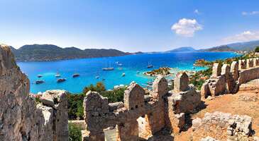 Antalya&rsquo;nın &ccedil;ok sevilen turistik cennetlerinden biri olan Demre, şehir merkezine yaklaşık 2,5 saat uzaklıkta yer alıyor. M&Ouml;. 5. y&uuml;zyıla uzanan etkileyici tarihi hazinelerinin yanı sıra Demre, el değmemiş doğası ve tertemiz deniziyle de &ccedil;ok &uuml;nl&uuml;. Likya d&ouml;neminin liman kentlerinden olan il&ccedil;e, aynı zamanda Noel Baba olarak bilinen Aziz Nikolaos&rsquo;ın yaşadığı yer olmasıyla da d&uuml;nya &ccedil;apında biliniyor. Gezinde sahil kenarında sıralanan salaş balık restoranlarında taze deniz &uuml;r&uuml;nleri ve y&ouml;resel mezeler tadarak da yorgunluk atabilirsin. Dilersen tekne gezileri ile dalış turlarına da katılabilirsin. Hazırsan Demre&rsquo;de gezilecek yerleri keşfedelim ve &ccedil;ok sorulan soruları yanıtlayalım. Demre nereye yakın? Antalya&rsquo;da yer alan Demre Kaş ve Finike il&ccedil;elerine yakın. Antalya-Demre arası ka&ccedil; kilometre? Antalya-Demre arası yaklaşık 142 kilometre. Yani ortalama 2 saat 20 dakika. Demre neyi ile meşhur? Demre &Uuml;&ccedil;ağız K&ouml;y&uuml;, Kekova Adası ve Kalek&ouml;y gibi turistik noktaları, Noel Baba Kilisesi, uygarlıkları ve denizi ile &uuml;nl&uuml;. 1. St. Nicholas Kilisesi Antalya'nın Demre il&ccedil;esinin en &ccedil;ok ziyaret edilen yerlerinden olan Noel Baba Kilisesi, Noel Baba olarak da bilinen Aziz Nikolaos'a adanmış tarihi bir yapı. M.S. 4. y&uuml;zyılda inşa edilen kilise, Hristiyanlar i&ccedil;in de &ccedil;ok &ouml;nemli bir hac yeri. Kilise, ayrıca &ccedil;ok pop&uuml;ler bir turistik destinasyon olarak binlerce insanı kendine &ccedil;ekiyor. M.S. 3. y&uuml;zyılda g&uuml;n&uuml;m&uuml;zde Demre olan Myra kentinde doğan piskopos ve din adamı Aziz Nikolaos, Noel Baba olarak d&uuml;nya &ccedil;apında bir &uuml;ne sahip oldu. C&ouml;mertliği ve yardımseverliği ile tanınan Aziz Nikolaos, zamanla efsanevi Noel Baba olarak bilinmeye başladı. Aziz Nikolaos'un &ouml;l&uuml;m&uuml;n&uuml;n ardından inşa edilen Noel Baba Kilisesi ise 11. y&uuml;zyılda Bizanslılar tarafından restore edilmiş bir tarihi hazinemiz. &Uuml;&ccedil; nefli olarak tuğla ve taştan &ouml;r&uuml;len kilisenin zemini, etkileyici mozaiklerle s&uuml;slenmiş. Kilisenin fresklerle s&uuml;sl&uuml; apsisi de g&ouml;r&uuml;lmeye değer g&uuml;zellikte. G&uuml;n&uuml;m&uuml;zde Hristiyanlar i&ccedil;in &ouml;nemli bir hac yeri haline gelen Noel Baba Kilisesi, her yıl Aziz Nikolaos'un anısını yaşatmak isteyen binlerce Hristiyan hacıyı ağırlıyor. Yıl boyu kilisede d&uuml;zenlenen etkinliklere de katılman m&uuml;mk&uuml;n. Demre merkezinde de il&ccedil;enin simgesi haline gelen Noel Baba temalı bir&ccedil;ok &uuml;r&uuml;n&uuml; hediyelik eşya d&uuml;kkanlarında bulabilirsin. Konum Linki {calismasaatleri}Giriş &uuml;creti 250 TL M&uuml;zeKart ve &ouml;ğretmen kartı ile &uuml;cretsiz A&ccedil;ık olduğu saatler Haftanın her g&uuml;n 08.00-17.30 saatleri arasında ziyaret edilebilir.{/calismasaatleri} {insightBoxStart}Yazar Notu: &Ouml;zellikle yaz aylarında pazar g&uuml;nleri kilise &ccedil;ok kalabalık olabiliyor. &Ouml;zel ayin ve etkinliklerde kilise ziyarete kapatılabiliyor.{insightBoxEnd} 2. Kekova Adası Demre&rsquo;de mutlaka keşfetmeni &ouml;nerdiğim yerlerden biri de Demre sahili a&ccedil;ıklarında bulunan ve bir kısmı sular altında kalan Kekova Adası (Batık Şehir). Likya d&ouml;neminden kalma tarihi kalıntılara ev sahipliği yapan Kekova Adası, tekne gezilerinin değişmez adreslerinden biri haline gelmiş durumda. Doğal g&uuml;zelliği ve tarihi &ouml;nemi ile &uuml;nl&uuml; Kekova Adası, aynı zamanda T&uuml;rkiye'nin en pop&uuml;ler tekne destinasyonları arasında. Likya d&ouml;neminden beri yerleşim yeri olarak kullanılan adada tiyatro, agoralar, nekropoller ve kiliseler gibi bir&ccedil;ok antik yapı bulunuyor. M.S. 2. y&uuml;zyılda meydana gelen bir deprem sonucu bir kısmı sular altında kalan Kekova Adası, bu nedenle Batık Şehir olarak da biliniyor. Yıl boyu d&uuml;zenlenen dalışlara katılarak da batık şehrin antik yapıları arasında y&uuml;zerek muhteşem fotoğraflar &ccedil;ekebilirsin. Turkuaz renkli denizi ve kayalık kıyı şeridiyle &ccedil;ok g&uuml;zel olan Kekova Adası&rsquo;nın etrafındaki k&uuml;&ccedil;&uuml;k koylar y&uuml;zmek ve g&uuml;neşlenmek i&ccedil;in ideal. Adanın en y&uuml;ksek noktası olan Teke Dağı'ndan ise &ouml;zellikle g&uuml;n batımlarında Akdeniz&rsquo;in muhteşem manzaralarını izleyebilirsin. Kekova Adası'na Demre'den kalkan ve genellikle 1-2 saat s&uuml;ren tekne turları ile kolayca ulaşabilirsin. Antalya&rsquo;da denize girilecek yerler i&ccedil;in de linke tıklayabilirsin. Konum Linki {insightBoxStart}Yazar Notu: Kekova Adası&rsquo;nı gezmek i&ccedil;in en az 2 saat ayırmak gerekiyor. Kayalık b&ouml;l&uuml;mleri &ccedil;ok olan ada sahilinde yanına deniz ayakkabısı almanı &ouml;neririm.{insightBoxEnd} 3. Myra Antik Kenti Likya uygarlığının en &ouml;nemli şehirlerinden biri olan Myra Antik Kenti, Demre gezilerinin değişmez adresleri arasında. M.&Ouml;. 5. y&uuml;zyılda kurulan Myra, Roma ve Bizans d&ouml;nemlerinde de b&ouml;lgedeki en &ouml;nemli kentler arasındaydı. Romalılar tarafından M.&Ouml;. 43 yılında ele ge&ccedil;irilen antik kent, uzun d&ouml;nem Likya'nın başkenti de oldu. G&uuml;n&uuml;m&uuml;zde kazı &ccedil;alışmalarının hala yapıldığı Myra Antik Kenti&rsquo;nde kaya mezarları, antik tiyatro ve Roma hamamı gibi tarihi yapıları keşfe &ccedil;ıkabilirsin. G&uuml;n&uuml;m&uuml;zde Myra Antik Kenti, &ouml;zellikle psikopos olan Noel Baba (Aziz Nikolaos) i&ccedil;in yaptırılan Noel Baba Kilisesi i&ccedil;in binlerce turisti kendine &ccedil;ekiyor. Likya d&ouml;neminde kayalara oyulan ve &ccedil;eşitli fig&uuml;rlerle s&uuml;slenmiş etkileyici kaya mezarları da antik kentin en &ccedil;ok ziyaret edilen yerleri arasında. M.S. 1. y&uuml;zyılda Romalılar tarafından inşa edilmiş 13.000 kişilik antik tiyatro ve M.S. 1. y&uuml;zyıldan kalma etkileyici Roma hamamını da antik kentte mutlaka g&ouml;rmeni &ouml;neririm. Konum Linki {calismasaatleri}Giriş &uuml;creti Kişi başı giriş 90 TL M&uuml;zeKart ile &uuml;cretsiz. A&ccedil;ık olduğu saatler Haftanın her g&uuml;n 10.00-20.00 saatleri arasında ziyaret edilebilir.{/calismasaatleri} {insightBoxStart}Yazar Notu: Myra Antik Kentini yaz aylarında gezeceksen havanın &ccedil;ok sıcak olabileceğini unutma. Ayrıca yanına mutlaka g&uuml;neş kremi, şapka ve yeterli miktarda su almanı &ouml;neririm.{insightBoxEnd} 4. Andriake Antik Kenti Demre&rsquo;de tarih ve k&uuml;lt&uuml;r meraklılarının mutlaka uğraması gereken yerlerden biri y&uuml;zlerce yıllık Andriake Antik Kenti. Myra Antik Kenti&rsquo;nin liman yerleşimi olan Andriake, ilk olarak M.&Ouml;. 5. y&uuml;zyılda kuruldu. Likya Birliği'nin en &ouml;nemli liman şehirlerinden biri olan Andriake&rsquo;de yapılan kazı &ccedil;alışmalarında ise binlerce paha bi&ccedil;ilmez tarihi eser bulundu. M.S. 1. y&uuml;zyılda Romalılar tarafından ele ge&ccedil;irilen Andriake Antik Kenti, Bizans d&ouml;neminde de &ouml;nemli bir liman kenti olarak hayatını s&uuml;rd&uuml;rd&uuml;. Antik kentte ilk g&ouml;rmen gereken yer ise Roma İmparatoru Hadrianus'un M.S. 130 yılında kenti ziyaretini anmak i&ccedil;in inşa edilmiş anıtsal Hadrian Kapısı. Kentin ticari ve sosyal merkezi olan agorada ise antik d&uuml;kkanlar, hamamlar ve stoalar arasında keyifli y&uuml;r&uuml;y&uuml;şler yapabilirsin. Roma d&ouml;neminden kalma en iyi korunmuş yapılardan olan tahıl ambarı Granarium ile Likya, Roma ve Bizans d&ouml;nemlerine ait anıt mezarları da gezinde yakından g&ouml;rebilirsin. Andriake Antik Kenti'ne hem Demre hem de Antalya şehir merkezinden otob&uuml;s veya minib&uuml;s ile rahat&ccedil;a ulaşabilirsin. Konum Linki {calismasaatleri}Giriş &uuml;creti Kişi başı giriş 90 TL M&uuml;zeKart ile &uuml;cretsiz. A&ccedil;ık olduğu saatler Haftanın her g&uuml;n 10.00-20.00 saatleri arasında ziyaret edilebilir.{/calismasaatleri} {insightBoxStart}İpucu: En iyi otel fiyatlarını tek bir yerde g&ouml;rmek, se&ccedil;eceğin otel hakkında bilgi almak ve saniyeler i&ccedil;inde rezervasyon yapmak i&ccedil;in ENUYGUN'da Demre otelleri araştırmasına başlayabilirsin.{insightBoxEnd} {hotel_search_form_banner} 5. Likya Uygarlıkları M&uuml;zesi Binlerce yıllık etkileyici bir ge&ccedil;mişi olan Demre&rsquo;nin tarihi hazinelerini g&ouml;rmek i&ccedil;in Likya Uygarlıkları M&uuml;zesi&rsquo;ne mutlaka uğramalısın. 2016 yılında a&ccedil;ılan m&uuml;ze, T&uuml;rkiye'nin en &ouml;nemli arkeoloji m&uuml;zelerinden biri olarak kabul ediliyor. M&uuml;zenin etkileyici koleksiyonlarında Likya uygarlığının tarihini ve eserlerini inceleme şansı bulabilirsin. Koleksiyonlarda Likya uygarlığına ait heykeller, kabartmalar, mozaikler, &ccedil;anak &ccedil;&ouml;mlekler ve sikkeler &ouml;zellikle &ccedil;ok ilgi g&ouml;r&uuml;yor. M&uuml;zenin başka bir &ouml;nemi de Likya uygarlığının sanatını, k&uuml;lt&uuml;r&uuml;n&uuml; ve g&uuml;nl&uuml;k yaşamını yansıtan etnografik eserler koleksiyonu. Likya Uygarlıkları M&uuml;zesi&rsquo;nde mutlaka g&ouml;rmeni &ouml;nerdiğim tarihi eser ise Myra Antik Kentinden getirilen ve Noel Baba olarak da bilinen Aziz Nikolaos'a ait ilgin&ccedil; lahit. Demre şehir merkezine yaklaşık 5 kilometre uzaklıktaki m&uuml;zeye taksi veya otob&uuml;sle kolayca ulaşabilir, Likya medeniyeti ile ilgili benzersiz bilgiler alabilirsin. Konum Linki {calismasaatleri}Giriş &uuml;creti Kişi başı giriş 75 TL M&uuml;zeKart ile &uuml;cretsiz. A&ccedil;ık olduğu saatler Haftanın her g&uuml;n 08.30-17.30 saatleri arasında ziyaret edilebilir.{/calismasaatleri} 6. Demre Taşdibi Plajı Demre&rsquo;de denize girmek i&ccedil;in en &ccedil;ok tercih edilen yerlerinden biri de her yıl bir&ccedil;ok yerli ve yabancı turisti kendine &ccedil;eken Taşdibi Plajı. Cam gibi berrak denizi ve ince kumlu sahiliyle &uuml;nl&uuml; plajda unutulmaz bir deniz g&uuml;n&uuml; yaşayabilirsin. Sakin ve huzurlu bir ortamda denize girmek isteyenler i&ccedil;in Taşdibi Plajı, en ideal adreslerden biri. Yaklaşık 3 kilometre uzunluğa bir kumsala sahip olan plajın denizi ise &ccedil;akıl ve kum karışımı. Sığ bir denizi olan plaj, acemi y&uuml;z&uuml;c&uuml;ler ve &ccedil;ocuklu ailelere de g&uuml;venli bir y&uuml;zme deneyimi sunuyor. Duş, tuvalet ve soyunma kabini gibi olanaklar bulabileceğin Taşdibi Plajı&rsquo;nda şezlong ve g&uuml;neş şemsiyesi de kiralayabilirsin. Plajda kano ve şnorkelli dalışlar gibi su sporları yaparak doyasıya eğlenebilir, g&uuml;zel bir g&uuml;n ge&ccedil;irebilirsin. Taşdibi Plajı'nda y&uuml;r&uuml;y&uuml;şlere katılarak ise Likya Yolu&rsquo;nda doğa y&uuml;r&uuml;y&uuml;şlerine &ccedil;ıkarak da etkileyici tarihi hazineleri keşfe &ccedil;ıkabilirsin. Plajın &ccedil;evresinde taze deniz &uuml;r&uuml;nlerinden Akdeniz mutfağından lezzetlere kadar &ccedil;eşitli se&ccedil;enekler bulabilirsin. Konum Linki 7. Kalek&ouml;y Tarihi hazinelerle doğal g&uuml;zelliklerin buluştuğu başka bir &ouml;zel yer olan Kalek&ouml;y (Simena) de Demre gezilerinin sevilen adresleri arasında. Hem masmavi denizi hem de tarihi hazineleri i&ccedil;in &ccedil;ok ziyaret edilen Kalek&ouml;y, Kekova Adası'nın hemen karşısında g&uuml;zel bir konumda uzanıyor. Sarp kayalıklar &uuml;zerine kurulu bir Rum k&ouml;y&uuml; ve antik Likya şehri olan Kalek&ouml;y, eşsiz atmosferiyle de her yıl binlerce turisti kendine &ccedil;ekiyor. İlk olarak M.&Ouml;. 4. y&uuml;zyılda kurulan ve d&ouml;neminde &ouml;nemli bir ticaret merkezi olan Kalek&ouml;y, Bizans d&ouml;neminden sonra terk edildikten sonra 19. y&uuml;zyılda Rumlar tarafından kullanıldı. Yemyeşil g&uuml;zellikler i&ccedil;inde gizlenen taş evleriyle &uuml;nl&uuml; k&ouml;y&uuml;n her k&ouml;şesinde tablo g&uuml;zelliğinde fotoğraflar &ccedil;ekebilirsin. Simena Kalesi&rsquo;nden b&ouml;lgenin panoramik manzaralarını izleyebileceğin gezinde Suna Suner Konağı gibi tarihi yapıları da yakından g&ouml;rebilirsin. Kekova Adası&rsquo;nın antik yapılarını gezebileceğin Kalek&ouml;y&rsquo;de batık şehre d&uuml;zenlenen t&uuml;pl&uuml; ve t&uuml;ps&uuml;z dalışlara katılarak da unutulmaz bir deneyim yaşayabilirsin. K&ouml;y&uuml;n sahilindeki restoranlarda ve kafelerde ise Akdeniz manzaraları eşliğinde b&uuml;y&uuml;leyici g&uuml;n batımı manzaralarının tadını &ccedil;ıkarabilirsin. Demre merkezine yaklaşık 25 kilometre uzaklıktaki Kalek&ouml;y&rsquo;e otob&uuml;sler ve taksilerle rahat&ccedil;a gitmek m&uuml;mk&uuml;n. Konum Linki {insightBoxStart}Yazar Notu: K&ouml;yde &ouml;zellikle yaz aylarında yiyecek ve i&ccedil;ecek fiyatları biraz y&uuml;ksek olabiliyor, bu nedenle yanında su ve atıştırmalık bulundurabilirsin. Ama buradayken mutlaka ke&ccedil;i s&uuml;t&uuml;nden yapılan dondurmanın tadına bakmalısın.{insightBoxEnd} 8. Demre Beymelek Lag&uuml;n&uuml; Sadece Demre&rsquo;nin değil, T&uuml;rkiye&rsquo;nin de g&ouml;r&uuml;lmeye değer tabiat g&uuml;zelliklerinden biri de Beymelek Lag&uuml;n&uuml;. Lag&uuml;n turkuaz renkli denizi, ince kumlu sahili ve el değmemiş g&uuml;zellikler arasında d&ouml;k&uuml;len şelalesiyle &uuml;nl&uuml;. Beymelek Lag&uuml;n&uuml;, her doğa tutkunu ve fotoğraf meraklısının mutlaka keşfetmesi gereken &ouml;zel yerler arasında. Yaklaşık 1 kilometre uzunluğundaki Beymelek Lag&uuml;n&uuml;, 500 metre genişliğe sahip. Tertemiz berrak sularına kendini bırakarak doyasıya y&uuml;zebileceğin lag&uuml;n&uuml;n denizi de &ccedil;ok sığ olduğu i&ccedil;in &ccedil;ocuklu aileler i&ccedil;in ideal. Hem lag&uuml;n hem de şelale etrafında muhteşem manzaraların tadını &ccedil;ıkarabileceğin y&uuml;r&uuml;y&uuml;ş yolları ve piknik alanları bulabilirsin. &Ccedil;evresinde kır bah&ccedil;eleri ve kafeler hizmet verdiği Beymelek Lag&uuml;n&uuml;, Demre merkezine ise yaklaşık 7 kilometre uzaklıkta yer alıyor. Konum Linki 9. Demre Kuş Cenneti Hem fotoğraf&ccedil;ılık hem de doğa meraklılarının Demre gezilerinde ilk uğraması gereken yer Demre Kuş Cenneti. 300'den fazla kuş t&uuml;r&uuml;ne ev sahipliği yapan kuş cenneti, aynı zamanda g&ouml;&ccedil;men kuşların da uğrak yerleri arasında yer alıyor. Doğa y&uuml;r&uuml;y&uuml;şlerinin değişmez adreslerinden olan Demre Kuş Cenneti, yıl boyunca kuş g&ouml;zlem gezilerine de ev sahipliği yapıyor. Yaklaşık 200 hektarlık geniş bir alana sahip olan Demre Kuş Cenneti i&ccedil;erisinde irili ufaklı bir&ccedil;ok k&uuml;&ccedil;&uuml;k g&ouml;l ve bataklık alanlar bulunuyor. Zengin su bitki &ccedil;eşitliliğine sahip kuş cennetinde flamingolar, pelikanlar, balık&ccedil;ılar, &ouml;rdekler ve kazlar gibi bir&ccedil;ok kuş t&uuml;r&uuml;n&uuml; yakından g&ouml;rerek kartpostal g&uuml;zelliğinde fotoğraflar &ccedil;ekebilirsin. Demre merkezinden otob&uuml;sler veya taksilerle 15 dakika i&ccedil;inde Demre Kuş Cenneti&rsquo;ne gitmen m&uuml;mk&uuml;n. Konum Linki {insightBoxStart}Yazar Notu: Demre Kuş Cenneti&rsquo;ni gezmek i&ccedil;in en g&uuml;zel zamanlar havanın serin ve kuş &ccedil;eşitliliğinin fazla olduğu ilkbahar ve sonbahar ayları. Gezinde yanına mutlaka d&uuml;rb&uuml;n ve fotoğraf makinesi almanı da &ouml;neririm. Kuş cennetine yiyecek ve i&ccedil;ecek sokmamaya, ayrıca &ccedil;evreye &ccedil;&ouml;p atmamaya da &ccedil;ok dikkat etmen gerekiyor.{insightBoxEnd} 10. Demre &Ccedil;ayağzı Demre&rsquo;nin en huzurlu cennet k&ouml;şelerinden biri de hem el değmemiş tabiatı hem de tarihi kalıntılarıyla dikkat &ccedil;eken &Ccedil;ayağzı. Deniz kaplumbağalarının az sayıdaki yuvalama alınlarından olan ince kumlu plajıyla da &uuml;nl&uuml; olan &Ccedil;ayağzı&rsquo;ın tertemiz mavi denizinde t&uuml;m g&uuml;n doyasıya y&uuml;zebilirsin. Myra'nın liman kenti olarak bilinen Andriake'nin kalıntıları &uuml;zerinde kurulan &Ccedil;ayağzı, antik d&ouml;nemde de &ouml;nemli bir limandı. Bizans d&ouml;neminden sonra terk edildikten sonra Rumların yerleştiği k&ouml;y&uuml;n her k&ouml;şesi birbirinden g&uuml;zel taş evlerle &ccedil;evrili. Gezinde Andriake ve Myra antik kentlerine kısa y&uuml;r&uuml;y&uuml;şlerle ulaşabilir, dağ eteklerine sıralanan antik yapıların fotoğraflarını &ccedil;ekebilirsin. Andriake Limanı kalıntıları ve Kalek&ouml;y Kalesi de &Ccedil;ayağzı gezinde mutlaka g&ouml;rmeni &ouml;nerdiğim yerler arasında. &Ccedil;ayağzı&rsquo;nda yaz aylarında her g&uuml;n d&uuml;zenlenen Kekova Adası tekne turlarına katılarak ise batık şehre unutulmaz dalışlar yapabilirsin. İstersen kilometrelerce uzanan Likya Yolu&rsquo;nda da tertemiz havada y&uuml;r&uuml;y&uuml;şlere &ccedil;ıkarak yılın b&uuml;t&uuml;n yorgunluğunu atabilirsin. Demre merkezine yaklaşık 5 kilometre uzaklıktaki &Ccedil;ayağzı'na hem ara&ccedil; kiralama hizmeti alarak hem de otob&uuml;sler veya taksilerle kolayca ge&ccedil;ebilirsin. Konum Linki {{campaignsSlider}} 11. Demre &Ccedil;ağıllı Plajı Finike ile Demre arasında gizlenen k&uuml;&ccedil;&uuml;k &Ccedil;ağıllı Plajı, kalabalıklardan uzakta denizin tadını &ccedil;ıkarmak isteyenlerin mutlaka uğraması gereken plajlardan biri. &Ccedil;oğunlukla aileler arasında tercih edilen plajın &ccedil;evresi yemyeşil &ccedil;am ormanlarıyla &ccedil;evrili. &Ccedil;akıl kum karışımı k&uuml;&ccedil;&uuml;k bir sahile sahip olan &Ccedil;ağıllı Plajı&rsquo;nın berrak denizinde balık s&uuml;r&uuml;leriyle birlikte doyasıya y&uuml;zebilirsin. Kalker kaya&ccedil;ların yay şeklinde uzandığı plajda tepelik alanlardan &ouml;zellikle g&uuml;n batımlarında muhteşem manzaralara şahit olabilirsin. Kamp yapmak i&ccedil;in de Demre&rsquo;deki en ideal adreslerden olan &Ccedil;ağıllı Plajı&rsquo;nda &ccedil;adırını kurarak yıldızlarla dolu g&ouml;ky&uuml;z&uuml;n&uuml; izleyebilirsin. &Ccedil;evresinde temel ihtiya&ccedil;larını alabileceğin k&uuml;&ccedil;&uuml;k turistik işletmelerin hizmet verdiği plaj, tekne ve yatların da sevilen mola noktalarından biri haline gelmiş durumda. En kalabalık yaz aylarında bile sakin atmosferini korumayı başaran &Ccedil;ağıllı Plajı&rsquo;nda yeşil ile mavinin buluştuğu b&uuml;y&uuml;leyici atmosferde yılın b&uuml;t&uuml;n yorgunluğunu atabilirsin. Konum Linki 12. S&uuml;l&uuml;kl&uuml; Plajı Demre&rsquo;nin saklı cennetlerinden biri olan S&uuml;l&uuml;kl&uuml; Plajı, Akdeniz&rsquo;in masmavi sularının tadını &ccedil;ıkarmak i&ccedil;in ideal bir adres. Turkuaz renkli denizi, kumsalı ve el değmemiş doğal g&uuml;zelliği ile &uuml;nl&uuml; olan S&uuml;l&uuml;kl&uuml; Plajı, yaklaşık 1 kilometre uzunluğunda bir kumsala sahip. İnce kumlu sahilinde t&uuml;m g&uuml;n g&uuml;neşlenebileceğin plajın denizi de sığ olduğu i&ccedil;in &ccedil;ocuklu aileler i&ccedil;in son derece g&uuml;venli. S&uuml;l&uuml;kl&uuml; Plajı&rsquo;nda duş, tuvalet ve soyunma kabini gibi temel ihtiya&ccedil;larını karşılayabileceğin tesisler hizmet veriyor. G&uuml;neş şemsiyesi ve şezlong kiralayabileceğin S&uuml;l&uuml;kl&uuml; Plajı&rsquo;nın berrak sularında şnorkelli dalışlar yaparak da b&uuml;y&uuml;leyici su altı manzaralarının tadını &ccedil;ıkarabilirsin. Plaj &ccedil;evresinde ilerleyen &uuml;nl&uuml; Likya Yolu&rsquo;nda da doğa y&uuml;r&uuml;y&uuml;şlerine &ccedil;ıkabilir, seyir alanlarından ise &ouml;zellikle g&uuml;n batımlarında tablo g&uuml;zelliğinde fotoğraflar &ccedil;ekebilirsin. Plajın etrafındaki restoranlarda ve kafelerde de &ccedil;arpıcı deniz manzarası eşliğinde romantik zamanlar ge&ccedil;irebilirsin. Konum Linki {insightBoxStart}Yazar Notu: Plajın kayalık alanlarında rahat etmek i&ccedil;in yanına deniz ayakkabısı alabilirsin. &Ccedil;ocuklu ailelerin de akıntılara karşı dikkat etmesi gerekiyor.{insightBoxEnd} 13. Kyaneai &Ouml;ren Yeri Likya medeniyetinin en gelişmiş şehirlerinden biri olan Kyaneai &Ouml;ren Yerini de Demre gezinde keşfe &ccedil;ıkabilirsin. M.&Ouml; 4.y&uuml;zyıldan g&uuml;n&uuml;m&uuml;ze kalan bir tarihi hazine olan Kyaneai, bulunduğu tepelik alanlardan sunduğu manzaralarla harika fotoğraflar &ccedil;ekme fırsatı sunuyor. Antik lahit ve kaya mezarlarını yakından g&ouml;rebileceğin antik kentin etkileyici kabartma fig&uuml;rleri de g&ouml;r&uuml;lmeye değer g&uuml;zellikte. Demre&rsquo;nin kuş bakışı manzaralarını izleyebileceğin Kyaneai &Ouml;ren Yeri&rsquo;nin g&uuml;n&uuml;m&uuml;ze kadar kalmayı başarmış antik tiyatrosunu da yakından inceleyebilirsin. Bizans ve Roma d&ouml;nemlerinde de aktif olarak kullanılan antik kent, hem doğa hem de fotoğraf&ccedil;ılık meraklılarının keyifle gezebileceği yerler arasında. Konum Linki {calismasaatleri}Giriş &uuml;creti &Uuml;cretsiz A&ccedil;ık olduğu saatler Haftanın her g&uuml;n 24 saat ziyaret edilebilir.{/calismasaatleri} 14. Tersane Koyu &Ccedil;ok sevilen tekne ve yat mola noktası olan Tersane Koyu&rsquo;nu Demre&rsquo;den her g&uuml;n hareket eden teknelerle keşfe &ccedil;ıkabilirsin. Tertemiz turkuaz denizi ve el değmemiş doğasıyla ilgi g&ouml;ren koy, yıl boyunca sakin ve huzurlu atmosferini korumayı başarıyor. T&uuml;m g&uuml;n denizin ve g&uuml;neşin tadını sessiz ortamda &ccedil;ıkarabileceğin Tersane Koyu&rsquo;nun ince kumlu sahilinde de &ccedil;adırını kurup kamp yapabilirsin. &Ccedil;evresi g&uuml;r &ccedil;am ormanlarla &ccedil;evrili koy, doğa y&uuml;r&uuml;y&uuml;şleri ve fotoğraf safarilerine &ccedil;ıkmak i&ccedil;in de ideal bir adres. Şnorkelli, t&uuml;pl&uuml; ve t&uuml;ps&uuml;z dalışlar yapmak i&ccedil;in sık&ccedil;a ziyaret edilen Tersane Koyu&rsquo;nun sularındaki antik kalıntıları da t&uuml;pl&uuml; ve t&uuml;ps&uuml;z dalışlar yaparak yakından g&ouml;rebilirsin. Konum Linki {insightBoxStart}Yazar Notu: Y&uuml;zerken veya dalışlar yaparken b&ouml;lgedeki sivri kayalık alanlara dikkat etmelisin.{insightBoxEnd} 15. Andrea Doria Koyu Demre&rsquo;de d&uuml;zenlenen tekne gezileri ve doğa y&uuml;r&uuml;y&uuml;şlerinin sevilen adreslerinden biri de b&uuml;y&uuml;leyici Andrea Doria Koyu. Berrak turkuaz deniziyle &uuml;nl&uuml; k&uuml;&ccedil;&uuml;k koy, Demre merkezine yaklaşık 25 kilometre uzaklıkta yer alıyor. Sarp kayalık alanlar ve &ccedil;am ormanlarıyla sarılı olan Andrea Doria Koyu, &ccedil;evresindeki tarihi kalıntıları i&ccedil;in de &ccedil;ok ziyaret ediliyor. İsmini 1956 yılında b&ouml;lgede batan Andrea Doria gemisinin batık kalıntılarından alan koy; şnorkelli, t&uuml;pl&uuml; ve t&uuml;ps&uuml;z dalışlar yapmak i&ccedil;in de Demre&rsquo;deki en g&uuml;zel noktalardan biri. &Ouml;zellikle koy &ccedil;evresindeki su altı mağaraları, g&ouml;r&uuml;lmeye değer g&uuml;zellikte. Andrea Doria Koyu&rsquo;nu Kekova batık şehir ile birlikte de keşfe &ccedil;ıkabilir, seyir alanlarından ise panoramik Akdeniz manzaraları izleyebilirsin. Sert dalga ve r&uuml;zgarlardan korunan koyun sakin dalgasız suları, &ccedil;ocuklu aileler i&ccedil;in de g&uuml;venli bir y&uuml;zme deneyimi sunuyor. Konum Linki 16. Kocakarı Koyu Demre merkezine sadece 40 kilometre uzaklıkta &Uuml;&ccedil;ağız K&ouml;y&uuml;&rsquo;n&uuml;n yanı başında saklanan k&uuml;&ccedil;&uuml;k Kocakarı Koyu, deniz tutkunlarının keşfetmesi gereken bir gizli cennet. Demre&rsquo;de yaz aylarında her sabah d&uuml;zenlenen doğa y&uuml;r&uuml;y&uuml;şleriyle koyu keşfe &ccedil;ıkabilirsin. Tekne gezileri ve dalış turlarıyla da sessiz ve huzurlu koya kolayca ulaşarak masmavi sulara kendini bırakarak doyasıya y&uuml;zebilirsin. Kamp yapmak i&ccedil;in de ideal bir nokta olan Kocakarı Koyu, &ccedil;evresindeki Aperlai Antik Kenti gibi tarihi hazineleriyle k&uuml;lt&uuml;r meraklılarına da keyifli bir gezi deneyimi yaşatıyor. Mavi yolculuk teknelerinin sık&ccedil;a mola verdiği Kocakarı Koyu, cam berraklığındaki denizi ile balık s&uuml;r&uuml;leri arasında t&uuml;pl&uuml; ve t&uuml;ps&uuml;z dalışlar yapmak i&ccedil;in de uğrayabileceğin yerler arasında. Konum Linki 17. Aperlai Antik Kenti Demre merkezine yaklaşık 27 kilometre uzaklıktaki Aperlai Antik Kenti, sadece Demre değil Kaş&rsquo;tan d&uuml;zenlenen doğa y&uuml;r&uuml;y&uuml;şleriyle de &ccedil;ok ziyaret ediliyor. Likya medeniyeti d&ouml;neminde b&ouml;lgenin &ouml;nemli yerleşim yerlerinden biri olan Aperlai Antik Kenti, d&ouml;neminde hareketli bir liman ve ticaret merkeziydi. Roma ve Bizanslılardan sonra terk edilen antik kentin deniz altında kalan tarihi harabeleri, t&uuml;pl&uuml; dalışlar yapmak i&ccedil;in ideal. Y&uuml;r&uuml;y&uuml;şlerin yanı sıra tekne gezileri ve dalış turlarıyla da keşfe &ccedil;ıkabileceğin Aperlai Antik Kenti&rsquo;nin sahilini kalabalıklardan uzakta doyasıya y&uuml;zerek yılın yorgunluğunu atabilirsin. B&ouml;lgedeki diğer antik kentlerle birlikte gezebileceğin Aperlai Antik Kenti&rsquo;nden g&uuml;n&uuml;m&uuml;ze kalan surlardan ise &ouml;zellikle g&uuml;n batımlarında benzersiz fotoğraflar &ccedil;ekebilirsin. Konum Linki {calismasaatleri}Giriş &uuml;creti &Uuml;cretsiz A&ccedil;ık olduğu saatler Haftanın her g&uuml;n 24 saat ziyaret edilebilir.{/calismasaatleri} 18. İsinda Antik Kenti Demre merkezine yaklaşık 40 kilometre uzaklıktaki Belenli K&ouml;y&uuml; sınırları i&ccedil;inde bulunan İsinda Antik Kenti, tarih ve k&uuml;lt&uuml;r meraklılarının ilgisini &ccedil;ekebilecek yerler arasında. Antik kent, tepelik bir alanda kurulmuş ve Likya medeniyetinin &ouml;nemli yerleşimleri arasında. Akropol&uuml;nde g&ouml;rebileceğin Likya dilinde yazılan yazıtlar ve lahit mezarlarıyla &ccedil;ok ilgi g&ouml;ren İsinda Antik Kenti&rsquo;nin M.&Ouml;. 4. y&uuml;zyılda kurulduğu tahmin ediliyor. Rehberli turlarla da gezebileceğin antik kentte hem İsinda hem de Likya medeniyetinin tarihini ve k&uuml;lt&uuml;r&uuml; hakkında ilgin&ccedil; bilgiler alabilirsin. &Ccedil;evresi el değmemiş g&uuml;zellikler ve &ccedil;am ormanlarıyla sarılı İsinda Antik Kenti&rsquo;ni doğa y&uuml;r&uuml;y&uuml;şleriyle de keyifle gezebilirsin. Tepelik alanlardan ise yeşil ormanların masmavi denizle birleştiği muhteşem manzaraları izleyerek gezinin en g&uuml;zel fotoğraflarını &ccedil;ekebilirsin. Konum Linki {calismasaatleri}Giriş &uuml;creti &Uuml;cretsiz A&ccedil;ık olduğu saatler Haftanın her g&uuml;n 24 saat ziyaret edilebilir.{/calismasaatleri} 19. Demre &Uuml;&ccedil;ağız K&ouml;y&uuml; Demre&rsquo;de tarih ve doğayla i&ccedil; i&ccedil;e benzersiz bir k&ouml;y olan &Uuml;&ccedil;ağız&rsquo;ı da mutlaka keşfe &ccedil;ıkmalısın. Binlerce yıllık tarihi kalıntılar, el değmemiş doğal g&uuml;zellikler ve masmavi deniziyle &uuml;nl&uuml; &Uuml;&ccedil;ağız&rsquo;da her b&uuml;t&ccedil;eye uygun oteller ve pansiyonlar hizmet veriyor. Likya d&ouml;neminden kalma kalıntılara ev sahipliği yapan k&ouml;y, Kekova Adası gezilerinin de değişmez mola noktalarından biri haline gelmiş durumda. Antik d&ouml;nemde Teimiussa adıyla bilinen bir Likya liman kenti olan &Uuml;&ccedil;ağız, uzun s&uuml;re de Myra Antik Kenti&rsquo;nin liman yerleşimi olarak kullanılmış. Likya d&ouml;neminden g&uuml;n&uuml;m&uuml;ze kalan tarihi hazineleriyle insanları kendine &ccedil;eken &Uuml;&ccedil;ağız&rsquo;da nekropoller, agoralar ve hamam kalıntıları arasında tarihte bir yolculuğa &ccedil;ıkabilirsin. &Uuml;&ccedil;ağız, tarihi hazinelerinin yanı sıra masmavi denizi ve yemyeşil doğasıyla ise yılın her mevsimi ruhunu dinlendirebileceğin &uuml;lkemizin gizli cennetlerinden biri. Tekne gezilerine &ccedil;ıkabileceğin k&ouml;yde Kekova Adası&rsquo;nı gezebilir ve batık şehrin antik hazinelerine dalışlar yapabilirsin. &Uuml;&ccedil;ağız doğa y&uuml;r&uuml;y&uuml;şleriyle ise dağ eteklerindeki antik yapıları keşfe &ccedil;ıkabilirsin. &Uuml;&ccedil;ağız gezinde sahil kenarında sıralanan salış balık restoranlarına uğrayarak b&uuml;y&uuml;leyici Akdeniz manzaraları eşliğinde taze deniz &uuml;r&uuml;nleri ve y&ouml;resel mezeler denemeyi de unutma. Konum Linki {insightBoxStart}İpucu:ENUYGUN&rsquo;da erken alınan biletler i&ccedil;in &ouml;zel fiyatlar bulunuyor. Bir sonraki sene i&ccedil;in tatilini ocak ayı sonuna kadar planlarsan u&ccedil;ak biletini &ccedil;ok daha uygun alabileceğini unutma! Seyahatinin ilk adımı olan&nbsp;Antalya u&ccedil;ak bileti&nbsp;almak i&ccedil;in tıkla.{insightBoxEnd} 20. Trysa Antik Kenti Demre&rsquo;nin saklı tarihi hazinelerinden olan Trysa Antik Kenti, Kaş ile Kale yolu &uuml;zerinde yer alıyor. M.&Ouml;. 2. y&uuml;zyılda kurulduğu tahmin edilen antik kent, &ccedil;ok az tarihi kaynakta kendine yer buluyor. Rehberli doğa y&uuml;r&uuml;y&uuml;şleriyle de gezebileceğin Trysa Antik Kenti, aynı zamanda antik Likya Yolu&rsquo;nun bir par&ccedil;ası. Likya Birliği &uuml;yelerinden biri olduğu bilinen antik kentin en ilgi &ccedil;eken b&ouml;l&uuml;m&uuml; ise dağ eteklerinde &ccedil;arpıcı bir manzara sunan Trysa Heroon. Tertemiz oksijeni y&uuml;ksek havada yenilenebileceğin Trysa Antik Kenti gezinde &ccedil;am ormanları arasında gizlenen kamp alanlarında da &ccedil;adırını kurarak yılın yorgunluğunu atabilirsin. Konum Linki {calismasaatleri}Giriş &uuml;creti &Uuml;cretsiz A&ccedil;ık olduğu saatler Haftanın her g&uuml;n 24 saat ziyaret edilebilir.{/calismasaatleri} Yaz tatili ile olduğu kadar k&uuml;lt&uuml;rel miraslarıyla da turizm cenneti olan Antalya&rsquo;da gezilecek yerler i&ccedil;in tıkla.