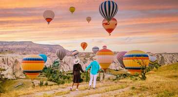 Kapadokya demek u&ccedil;suz bucaksız vadiler ve heybetli peribacalarının yanında muhteşem balon manzarası demek. G&uuml;neş doğmadan &ouml;nce havalanan devasa sıcak hava balonlarının kartpostalları aratmayan g&ouml;r&uuml;nt&uuml;s&uuml; karşısında b&uuml;y&uuml;leneceksin. Rengarenk balonlar y&uuml;kselirken birbirinden g&uuml;zel fotoğraflar &ccedil;ekerek bu anı &ouml;l&uuml;ms&uuml;zleştirebilirsin.&nbsp; Son yıllarda Kapadokya&rsquo;ya artan ilgi nedeniyle b&ouml;lgede neredeyse her t&uuml;rl&uuml; aktivite &uuml;cretli hale geldi. Bu eşsiz manzarayı izlemek i&ccedil;in bile giriş &uuml;creti istenen tepeler bulunuyor. Merak etme ENUYGUN.com olarak sana 1 kuruş bile &ouml;demeden sadece r&uuml;zgarın sesini dinleyebileceğin ve y&uuml;zlerce balonun manzarasını izleyebileceğin rotalar s&ouml;yleyeceğiz. Hadi birlikte kalabalıktan uzak, cebini yakmayan ve Instagram hikayelerini şenlendirecek 3 tepeyi inceleyelim.&nbsp; 1. Kılı&ccedil;lar Vadisi &uuml;st&uuml; Kapadokya&rsquo;da balon manzarası izlemek i&ccedil;in en pop&uuml;ler nokta G&ouml;reme merkezde konumlanan meşhur Aydınlı Orta Mahallesi&rsquo;ndeki tepe. Son yıllarda yoğun ilgi g&ouml;rmesiyle burası artık &uuml;cretli hale geldi. &Uuml;cretsiz bir şekilde manzaranın tadını &ccedil;ıkarmak i&ccedil;in rotanı Kılı&ccedil;lar Vadisi&rsquo;nin sırtlarına kırmanı tavsiye ederiz. Burada manzarayı izlerken balonlar neredeyse burnunun dibinden ge&ccedil;ecek. Sıcak hava balonları o kadar yakından ge&ccedil;iyor ki balon i&ccedil;indekilerin g&uuml;naydın dediğini bile duyacaksın.&nbsp; Konum Linki {insightBoxStart}Yazar Notu: ATV ya da ara&ccedil;la ile gideceksen parkurun başına aracı bıraktıktan sonra ortalama 5 dakika yukarı doğru y&uuml;r&uuml;melisin.{insightBoxEnd} 2. G&ouml;reme&rsquo;den Bağlıdere Vadisi&rsquo;ne giden yol G&ouml;reme Merkez&rsquo;den Bağlıdere Vadisi&rsquo;ne doğru giden yoldaki balon seyir terasına giderek hem g&uuml;n doğumunu hem de g&ouml;ky&uuml;z&uuml;ne y&uuml;kselen devasa balonları izleyebilirsin. Buraya &ccedil;ıktığında t&uuml;m G&ouml;reme ayaklarının altında olacak. Sabah saatlerinde kızıla d&ouml;nen g&ouml;ky&uuml;z&uuml; karşısında nefesinin kesileceğinden eminiz.&nbsp; Konum Linki {insightBoxStart}Yazar Notu: Yol boyunca manzarayı g&ouml;rebileceği g&uuml;venli ceplerde durarak balon seyir terasından daha sakin bir ortamda manzaranın tadını &ccedil;ıkarabilirsin.{insightBoxEnd} 3. G&uuml;l Vadisi ve &ccedil;evresi G&uuml;l Vadisi yakınlarındaki &uuml;cretsiz bir diğer balon izleme noktasında ise hem u&ccedil;suz bucaksız vadiyi izleyebilir hem de g&uuml;n doğumunu izleyebilirsin. Sabahın erken saatlerinde g&ouml;ky&uuml;z&uuml; kızıla d&ouml;nerken y&uuml;zlerce rengarenk balon ortaya unutulmaz bir g&ouml;r&uuml;nt&uuml; &ccedil;ıkarıyor.&nbsp; Konum Linki {insightBoxStart}Yazar Notu: Bu noktaya giden yollar genellikle dik yokuşlar olduğundan rahat ve kaydırmaz y&uuml;r&uuml;y&uuml;ş ayakkabıları giymeyi ihmal etmemelisin.{insightBoxEnd} {insightBoxStart}İpucu: En iyi otel fiyatlarını tek bir yerde g&ouml;rmek, se&ccedil;eceğin otel hakkında bilgi almak ve saniyeler i&ccedil;inde rezervasyon yapmak i&ccedil;in ENUYGUN'da Kapadokya otelleri araştırmasına başlayabilirsin.{insightBoxEnd} {hotel_search_form_banner} Bunları mutlaka bilmelisin&nbsp; Kapadokya&rsquo;da eşsiz manzarayı yakalamak ve rahat bir şekilde izlemek i&ccedil;in bilmen gereken birka&ccedil; detay bulunuyor.&nbsp; G&uuml;n doğmadan en az 45 dakika &ouml;nce izleme noktalarında olmalısın. Erken giderek hazırlık aşamasında ortaya &ccedil;ıkan alevleri de g&ouml;rebilirsin.&nbsp; Balonlar uygun hava ve r&uuml;zgar koşulları olduğunda u&ccedil;ar. Yola &ccedil;ıkmadan &ouml;nce mutlaka hava durumunu kontrol etmelisin. Aksi halde balon manzarasını g&ouml;remeyebilirsin.&nbsp; Sabah saatleri serin olacağı i&ccedil;in yaz aylarında gitsen bile yanına hırka ya da hafif bir mont almayı unutma.&nbsp; &Uuml;cretsiz seyir noktalarında genelde market veya lavabo olmaz. Hazırlıklı gitmen konforlu bir seyir i&ccedil;in &ccedil;ok &ouml;nemli. Manzaranın keyfini yaşarken sıcacık i&ccedil;eceğini yudumlamak istiyorsan bir termosa &ccedil;ay-kahve yapmanı &ouml;neririz. Balon manzarası ortalama 1-1,5 saat s&uuml;receği i&ccedil;in ara&ccedil;la gideceksen kamp sandalyesi g&ouml;t&uuml;rmek b&uuml;y&uuml;k rahatlık sağlar.&nbsp; Balonların oluşturduğu renk c&uuml;mb&uuml;ş&uuml;n&uuml; her anını &ccedil;ekmek isteyeceksin. Bu y&uuml;zden telefonunun şarjının veya fotoğraf makinesinin bataryasının dolu olduğundan emin olmalısın. Gizli rotalarda, sakin ve huzurlu bir şekilde manzarayı izledikten sonra b&ouml;lgeyi keşfetmek istersen diye Kapadokya&rsquo;da gezilecek yerler yazımızı da buraya bırakalım.