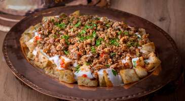 Bazen sadece doymak değil, bir sofra sıcaklığında 'evimdeyim' hissi yaşamak istersin. Kastamonu, bu hissi sonuna kadar yaşayabileceğin yerlerin başında geliyor. Anadolu&rsquo;nun zengin ge&ccedil;mişini g&uuml;n&uuml;m&uuml;ze taşıyan Kastamonu, her sokağında farklı bir lezzet sırrı saklıyor. Kastamonu, gastronomi tutkunları i&ccedil;in keşfedilmeyi bekleyen devasa bir hazine sunuyor. Karadeniz&rsquo;in yeşil doğası ile i&ccedil; kesimlerin bereketli topraklarının harmanlandığı bu y&ouml;resel mutfakta binlerce yıllık ge&ccedil;mişiyle "ilk buğday" kabul edilen siyezden d&uuml;nyaca &uuml;nl&uuml; Taşk&ouml;pr&uuml; sarımsağına kadar her malzeme, kendine has bir hik&acirc;ye anlatıyor.&nbsp; Kastamonu, kayıtlara ge&ccedil;miş 800&rsquo;den fazla yemek &ccedil;eşidi ile T&uuml;rkiye&rsquo;nin en zengin yerel mutfaklarından birine sahip. Bu şehirde sofralar, sadece karın doyurmak i&ccedil;in değil, her lokmada bir k&uuml;lt&uuml;rel mirası deneyimlemek i&ccedil;in kuruluyor. Kastamonu&rsquo;da asırlık mutfaklardan izler taşıyan ve doğallığın başrolde olduğu unutulmaz bir lezzet yolculuğuna &ccedil;ıkabilirsin. 1. Kuyu kebabı Kastamonu mutfağının zirve noktası sayılan kuyu kebabı, iki asırlık ge&ccedil;mişiyle tam bir sabır ve ustalık eseri. Bu kebabı &ouml;zel kılan şey ise yaklaşık iki metre derinliğindeki tuğla &ouml;r&uuml;l&uuml; &ouml;zel kuyularda, sadece meşe odunu ateşi ve etin kendi buharı ile pişirilmesi. S&uuml;t kuzularının &ccedil;engellere asılarak kuyunun i&ccedil;ine sarkıtılması ve kuyunun ağzının &ccedil;amurla kapatılması, etin lokum gibi yumuşacık kalmasını sağlıyor. Kuyu kebabının o isle karışmış kokusu sokağın başında seni karşılayacak. Yumuşacık etin elinde bıraktığı sıcaklık, seni yabancısı olmadığın sofralara g&ouml;t&uuml;recek. Kuyu kebabı, baharat eklenmeden sadece etin kendi doğal aroması ve meşe dumanının verdiği hafif isli tadı ile servis ediliyor. Kastamonu&rsquo;da bu kebap, geleneksel olarak sabahın erken saatlerinde bile t&uuml;ketilmeye başlanıyor. Yanında taze soğan ve fırından yeni &ccedil;ıkmış sıcak pide ile sunulan kuyu kebabı, şehrin gastronomi kimliğinin en g&uuml;&ccedil;l&uuml; temsilcisi. 2. Banduma Kastamonu&rsquo;da "bey sofrası" olarak adlandırılan en &ouml;zel lezzetlerinden biri olan banduma, kış aylarının vazge&ccedil;ilmez doyurucu ana yemeği. Bu eşsiz lezzetin temelini, incecik a&ccedil;ılmış yufkaların rulo yapılıp kesilmesi ve ardından hindi veya kaz suyuna tek tek bandırılarak tepsiye dizilmesi oluşturuyor. Yufkaların arasına bolca gezdirilen eritilmiş tereyağı ve &uuml;zerine serpiştirilen d&ouml;v&uuml;lm&uuml;ş Kastamonu cevizleri ise yemeğe hem karakteristik bir &ccedil;ıtırlık hem de derin bir aroma katıyor. En &uuml;st katmana eklenen didiklenmiş hindi etleriyle banduma, karbonhidratın protein ve sağlıklı yağlarla buluştuğu tam bir enerji deposu. Kalabalık sofraların ve &ouml;zel misafir ağırlamalarının baş tacı olan bu y&ouml;resel yemek, Kastamonu&rsquo;nun hamur işi k&uuml;lt&uuml;r&uuml;ndeki ustalığını g&ouml;steriyor. 3. Kastamonu etli ekmeği Kastamonu&rsquo;da en &ccedil;ok t&uuml;ketilen lezzetlerinden olan Kastamonu etli ekmeği, T&uuml;rkiye&rsquo;deki diğer etli ekmeklerden tamamen farklı bir hazırlanış ve sunum tekniğine sahip. İncecik a&ccedil;ılan mayasız hamurun yarısına, &ouml;zel olarak hazırlanan bol soğanlı ve baharatlı kıyma harcı yayılıyor. Ardından hamurun yarım ay şeklinde kapatılmasıyla etli ekmekler hazırlanıyor. Geleneksel olarak sac &uuml;zerinde pişirilen etli ekmek, pişme esnasında dışı hafif&ccedil;e kızaran, i&ccedil;i ise kıymanın suyuyla yumuşacık kalan kapalı bir lahmacuna benziyor. Ocaktan alındıktan sonra &uuml;zerine s&uuml;r&uuml;len taze tereyağı ise tam bir lezzet patlaması yaşatıyor. &Ccedil;arşı fırınlarında ve yerel lokantalarda sıcak sıcak, yanında bol k&ouml;p&uuml;kl&uuml; bir yayık ayranı ile deneyebileceğin Kastamonu etli ekmek, ustalık gerektiren hamur işi k&uuml;lt&uuml;r&uuml;n&uuml;n en sevilen simgesi. 4. Simit tiridi Kastamonu mutfağının israfı &ouml;nleyen ve lezzet ustalığını en g&uuml;zel şekilde &ouml;zetleyen lezzeti ise simit tiridi. Şehrin meşhur "kel simidi" &uuml;zerine inşa edilen bu lezzet, tam bir y&ouml;resel klasik kahvaltı ve akşam yemeği &ouml;ğ&uuml;n&uuml;. Simit tiridinin temelini, susamsız hazırlanan ve &ouml;zel bir pekmezli suda haşlanarak pişirilen bayat simitlerin, derin bir tabakta kemik suyu ile tek tek ıslatılması oluşturuyor. Islanan ve yumuşayan simitlerin &uuml;zerine d&ouml;k&uuml;len bol sarımsaklı s&uuml;zme yoğurt, bu yemeğe ferahlatıcı bir asidite katıyor. En &uuml;st katmana eklenen tereyağında kavrulmuş kıyma ve pul biberli sos ise simit tiridini doyurucu bir ana yemeğe d&ouml;n&uuml;şt&uuml;r&uuml;yor. Geleneksel olarak b&uuml;y&uuml;k tepsilerde sunulan ve her lokmada kemik suyunun derin aromasını hissettiren simit tiridi, Kastamonu&rsquo;nun yerel fırın k&uuml;lt&uuml;r&uuml;n&uuml;n bir par&ccedil;ası. 5. Ekşili pilav Kastamonu mutfağının en sağlıklı yemeklerinden olan ekşili pilav, d&uuml;nyaca &uuml;nl&uuml; coğrafi işaretli siyez bulgurunun başrolde olduğu, alışılmışın dışında bir ana yemek. Bu lezzet, klasik pilavların aksine s&uuml;zme yoğurt ve un ile hazırlanan ayran kıvamındaki bir suyun i&ccedil;inde pişiriliyor. Ekşili pilav, damakta bıraktığı hafif mayhoş tadından adını alıyor. Pilava asıl ruhunu veren ise Kastamonu&rsquo;nun dağlarından ve bah&ccedil;elerinden toplanan taze nane, ısırgan otu, ebeg&uuml;meci ve dereotu gibi şifalı yeşilliklerin bolca kullanılması. Ekşili pilav, &uuml;zerine eklenen tereyağında yakılmış kuru soğan ve pul biberli sosla birlikte servis ediliyor. Bu y&ouml;resel pilav, Kastamonu&rsquo;nun binlerce yıllık tarım mirasını ve doğayla i&ccedil; i&ccedil;e ge&ccedil;en mutfak k&uuml;lt&uuml;r&uuml;n&uuml; yansıtıyor. {insightBoxStart}İpucu: Kastamonu'nun enfes lezzetlerinden oluşan bu sofrada yerini &ccedil;oktan hazırladık. Peki kalacağın oteli de birlikte se&ccedil;elim mi? En iyi otel fiyatlarını tek bir yerde g&ouml;rmek, se&ccedil;eceğin otel hakkında bilgi almak ve saniyeler i&ccedil;inde rezervasyon yapmak i&ccedil;in ENUYGUN'da Kastamonu otelleri araştırmasına başlayabilirsin.{insightBoxEnd} {hotel_search_form_banner} 6. Ecevit &ccedil;orbası Kastamonu&rsquo;nun İnebolu yolu &uuml;zerindeki tarihi Ecevit Ge&ccedil;idi&rsquo;nden adını alan Ecevit &ccedil;orbası, bir yol &uuml;st&uuml; lezzetinden mutfak klasiğine d&ouml;n&uuml;şm&uuml;ş şifalı başlangı&ccedil; yemeklerinden biri. S&uuml;zme yoğurt, yumurta, un ve pirincin m&uuml;kemmel uyumu ile hazırlanan bu y&ouml;resel &ccedil;orba, ilk bakışta geleneksel yayla &ccedil;orbasını andırıyor. &Ccedil;orba, pişirilme tekniği ve i&ccedil;ine eklenen yerel malzemelerle ise bambaşka bir derinlik kazanıyor. Ağır ateşte sabırla karıştırılarak kıvam alan &ccedil;orbaya asıl ruhunu veren dokunuş ise servis esnasında &uuml;zerine gezdirilen bol naneli ve pul biberli kızgın tereyağı. Ecevit &ccedil;orbası, &ouml;zellikle kış aylarında i&ccedil; ısıtan, mideyi yormayan ve iştah a&ccedil;ıcı &ouml;zellikleri ile &ccedil;ok seviliyor. Bir kase Ecevit &ccedil;orbasının, yolculuğun omuzlarına y&uuml;klediği o yorgunluğu nasıl bir anda attığına inanamayacaksın. 7. Kastamonu &ccedil;ekme helvası Kastamonu mutfağının en ikonik simgesi sayılan &ccedil;ekme helvası, bir tatlıdan &ouml;te sabır ve ustalık gerektiren geleneksel bir sanat eseri. Saray mutfağından g&uuml;n&uuml;m&uuml;ze uzanan &ccedil;ekme helvaları, un, şeker ve bol miktarda kaliteli tereyağının saatlerce yoğrulup &ccedil;ekilmesi ile hazırlanıyor. Pişmaniyeyi andıran ancak &ccedil;ok daha yoğun, sıkıştırılmış ve ağızda anında dağılan karakteristik dokusu ile &ccedil;ekme helvası, diğer helva t&uuml;rlerinden keskin bir şekilde ayrılıyor. &Ccedil;ekme helvası, kar tanelerini andıran bembeyaz rengi ve damağa yayılan yoğun tereyağı aroması ile &uuml;nl&uuml;. Helvalar, g&uuml;n&uuml;m&uuml;zde sade halinin yanı sıra fıstıklı, kakaolu ve &ccedil;ikolata kaplı &ccedil;eşitleriyle de hem yerel sofraları s&uuml;sl&uuml;yor. &Ccedil;ekme helvası, aynı zamanda en &ccedil;ok satın alınan bir hediyelik. 8. Cırık tatlısı Kastamonu&rsquo;nun en sevilen sokak lezzetlerinden olan cırık tatlısı, &ouml;zellikle panayır ve festivallerin vazge&ccedil;ilmez simgesi. Geleneksel bir lokma &ccedil;eşidi olan bu tatlıyı &ouml;zel kılan ise mayalı hamurun kızgın yağda altın sarısı bir renk alana kadar ustalıkla kızartılması ve ardından soğuk şerbetle buluşturulması. Cırık tatlısı, dışı &ccedil;ıtır &ccedil;ıtır, i&ccedil;i ise şerbetini tam &ccedil;ekmiş yumuşacık dokusuyla damaklarda dengeli bir tat bırakıyor. Bu y&ouml;resel tatlı, Kastamonu &ccedil;arşılarında taze ve sıcak t&uuml;ketilen bir enerji deposu. Hafifliği ve samimi sunumu ile Kastamonu&rsquo;nun sosyal yaşamında da &ouml;nemli bir yere sahip olan cırık tatlısı, Kastamonu&rsquo;nun m&uuml;tevazı ama bir o kadar da iştah a&ccedil;ıcı hamur işi k&uuml;lt&uuml;r&uuml;n&uuml;n en g&uuml;zel simgesi. 9. &Uuml;ryani eriği tatlısı Kastamonu&rsquo;nun coğrafi işaretli bir değeri olan &Uuml;ryani eriği tatlısı, şehrin endemik meyve k&uuml;lt&uuml;r&uuml;n&uuml; sofralara taşıyan en &ouml;zel son dokunuş. Sadece bu b&ouml;lgeye has, ince kabuklu ve &ccedil;ekirdeğinden kolayca ayrılan m&uuml;rd&uuml;m eriği &ccedil;eşidinin kurutulmasıyla hazırlanan bu tatlı, rafine şeker kullanılmayan doğal ve mayhoş aroması ile &uuml;nl&uuml;. Genellikle az miktarda bal ile ağır ateşte pişirilerek hazırlanan bu &ouml;zel tatlı, sindirimi kolaylaştırıcı bir hoşaf olarak, &ouml;zellikle ağır et yemeklerinin ve hamur işlerinin ardından ferahlatıcı bir denge sağlıyor. Kastamonu&rsquo;nun dağlarından s&uuml;z&uuml;len doğal aromayı bir kasede buluşturan &Uuml;ryani eriği tatlısı, kentin geleneksel meyve kurutma ustalığının en lezzetli &ouml;rneği. {{campaignsSlider}} 10. Kaşık helvası Kastamonu un helvasının en zarif ve ustalık gerektiren formu olan kaşık helvası, az malzeme ile &ouml;zel bir lezzet yaratılabileceğinin kanıtı. Bu geleneksel tatlının sırrı ise un ve y&uuml;ksek kaliteli tereyağının, rengi tam kıvamına gelene ve o karakteristik kavruk kokusu yayılana kadar b&uuml;y&uuml;k bir sabırla kavrulmasında saklı. Kavurma işleminin ardından pudra şekeri eklenen ve hen&uuml;z sıcakken yemek kaşıklarıyla tek tek şekil verilen helva, ağızda anında dağılan eşsiz dokusu ile &uuml;nl&uuml;. S&uuml;slemesinde genellikle Kastamonu&rsquo;nun meşhur d&ouml;v&uuml;lm&uuml;ş cevizlerinin kullanıldığı kaşık helvası, sadeliği zarafetle buluşturması ile bayram sofralarının ve &ouml;zel misafir ikramlarının vazge&ccedil;ilmez. 11. Cevizli incir dolması Kastamonu&rsquo;nun en besleyici tatlılarından olan cevizli incir dolması, b&ouml;lgenin y&uuml;ksek kaliteli cevizlerinin başrolde olduğu bir lezzet. Kurutulmuş ve yumuşatılmış incirlerin i&ccedil;inin iri d&ouml;v&uuml;lm&uuml;ş Kastamonu cevizleri ile bolca doldurulması ile hazırlanan tatlı, az miktarda şeker ve suyla ağır ateşte, incirler şerbetini tam &ccedil;ekene kadar pişiriliyor. İncirin doğal aromasıyla cevizin karakteristik tadının m&uuml;kemmel bir uyum sağladığı dolma, servis aşamasında &uuml;zerine eklenen taze kaymak veya bolca serpiştirilen ceviz i&ccedil;iyle zenginleştiriliyor. Hafifliği ve doyuruculuğu ile bilinen cevizli incir dolması, &ouml;zellikle kış aylarında Kastamonu sofralarının en zarif ve şifalı tatlarından. 12. Eğşi (Elma veya erik) Kastamonu&rsquo;nun en &ouml;zg&uuml;n ve ferahlatıcı i&ccedil;eceklerinden olan eğşi, doğanın sunduğu saflığı sofralara taşıyan geleneksel bir meyve suyu. Bu y&ouml;resel i&ccedil;ecek, dağlarda kendiliğinden yetişen yabani elma veya eriklerin toplanıp b&uuml;y&uuml;k kazanlarda kaynatılması, ardından da ince s&uuml;zge&ccedil;lerden ge&ccedil;irilerek meyve &ouml;z&uuml;n&uuml;n &ccedil;ıkarılması ile hazırlanıyor. Eğşi i&ccedil;eriğinde hi&ccedil;bir yapay koruyucu veya rafine şeker bulunmuyor. İ&ccedil;ecek, meyvenin kendi doğal şekerinden gelen hafif mayhoş tadı ve iştah a&ccedil;ıcı aroması ile &ouml;ne &ccedil;ıkıyor. Eğşi, Kastamonu sofralarında &ouml;zellikle ağır et yemeklerinin ve yağlı hamur işlerinin yanında sindirimi kolaylaştırıcı, mideyi rahatlatıcı bir eşlik&ccedil;i olarak t&uuml;ketiliyor. Yazın buz gibi i&ccedil;ilen, kışın ise vitamin deposu olarak t&uuml;ketilen eğşi, Kastamonu&rsquo;nun doğal yaşamla kurduğu k&ouml;kl&uuml; bağın bir kanıtı. 13. Kiren (Kızılcık) şerbeti Kastamonu&rsquo;da "kiren" olarak bilinen ve dağların yama&ccedil;larından toplanan yabani kızılcıklardan hazırlanan kiren şerbeti, şehrin gastronomi k&uuml;lt&uuml;r&uuml;ndeki en ferahlatıcı i&ccedil;eceklerinden biri. Parlak yakut kırmızısı rengi ile &uuml;nl&uuml; bu geleneksel i&ccedil;ecek, meyvelerin &ouml;z&uuml;n&uuml;n &ccedil;ıkarılıp az miktarda şekerle kaynatılmasıyla elde ediliyor. C vitamini deposu olan kiren şerbeti, damakta bıraktığı kendine has buruk, mayhoş ve tatlı dengesi ile kuyu kebabı veya banduma gibi yoğun lezzetlerin yanında sofrayı dengeliyor. Kastamonu&rsquo;nun doğal yaşamını yansıtan bu aromatik şerbet, sindirimi kolaylaştırıcı etkisi ve her yudumda hissedilen meyve tazeliği ile Kastamonu kentinin i&ccedil;ecek k&uuml;lt&uuml;r&uuml;nde &ouml;zel bir yere sahip. 14. Pastırmalı ekmek Kastamonu&rsquo;nun Kayseri ile girdiği tatlıbir rekabetin eseri olan pastırmalı ekmek, şehrin fırın k&uuml;lt&uuml;r&uuml;n&uuml; ve şark&uuml;teri ustalığını tek bir lezzette buluşturuyor. İ&ccedil; har&ccedil;, doğal y&ouml;ntemlerle kurutulan, &ccedil;emen kokusuyla iştah kabartan meşhur Kastamonu pastırmalarının incecik dilimlenip bol soğan, maydanoz ve pul biberle harmanlanması ile hazırlanıyor. Bu &ouml;zel i&ccedil; har&ccedil;, ince a&ccedil;ılmış ekmek hamuruna ekleniyor. Bu lezzet, odun ateşinde taş fırınlarda dışı &ccedil;ıtır, i&ccedil;i ise pastırmanın kendi yağı ve suyuyla yumuşacık kalacak şekilde pişiriliyor. Fırından &ccedil;ıktıktan sonra pastırmalı ekmek, &uuml;zerine s&uuml;r&uuml;len taze tereyağı ile servis ediliyor. &Ouml;zellikle &ccedil;arşı i&ccedil;indeki fırınlarda sıcak t&uuml;ketilen pastırmalı ekmek, Kastamonu&rsquo;da sadece bir &ouml;ğ&uuml;n değil, k&ouml;kl&uuml; esnaf geleneklerinin de simgesi. 15. Kastamonu gazozu Kastamonu mutfağının nostaljik ve ferahlatıcı y&uuml;z&uuml;n&uuml; temsil eden Kastamonu gazozu, sofraların en sevilen eşlik&ccedil;ilerinden biri. On yıllardır değişmeyen &ouml;zel form&uuml;l&uuml; ile &uuml;retilen bu yerel gazoz, piyasadaki benzerlerinden &ccedil;ok daha hafif şeker oranı ve kendine has meyvemsi aromasıyla ayrılıyor. Kastamonu gazozu, &ouml;zellikle yoğun kıvamlı Kastamonu etli ekmeği veya fırından yeni &ccedil;ıkmış pastırmalı ekmek gibi hamur işi lezzetlerin yanında damaktaki tadı dengeliyor. Cam şişesinden gelen o nostaljik serinliği ve her yudumda hissedilen dengeli asit yapısı ile Kastamonu gazozu, sadece &ccedil;ocukların değil, her yaştan lezzet tutkununun sevdiği bir klasik. Bu enfes lezzetleri yerinde denemek i&ccedil;in Kastamonu&rsquo;da gezilecek yerler yazımızı inceleyebilir, rotanı oluşturabilirsin.