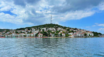 İstanbul'un adaları, şehrin kalabalığından ka&ccedil;mak isteyenler i&ccedil;in adeta birer sığınak. Bu adalardan biri de Kınalıada. Eşsiz deniz manzarası, tarihi dokusu ve sakin atmosferi ile Kınalıada, adeta bir tatil cenneti. Kınalıada, Prens Adaları&rsquo;nın d&ouml;rd&uuml;nc&uuml; en b&uuml;y&uuml;k adası ancak bir ucundan diğer ucuna y&uuml;r&uuml;mek sadece 30 dakika s&uuml;r&uuml;yor.&nbsp; Kınalıada&rsquo;nın tarihte bir&ccedil;ok ismi olmuş. Port, Proty, Akoni, Akonidis tarihteki eski isimlerinin bazıları. Şimdiki adını ise sahip olduğu bitki &ouml;rt&uuml;s&uuml; makilerin uzaktan g&ouml;r&uuml;n&uuml;ş&uuml; kızıl renkli olmasından dolayı almış. Kınalıada İstanbul&rsquo;a yakın olması nedeniyle tarihte s&uuml;rg&uuml;n adası olarak da sık&ccedil;a kullanılmış. Adaya Bostancı, Kadık&ouml;y, Emin&ouml;n&uuml;, Kabataş ve Karak&ouml;y&rsquo;den kalkan vapur ve motorlarla keyifli bir deniz yolculuğu sonucunda ulaşabilirsiniz. Sefer sıklıkları yaz-kış veya hafta i&ccedil;i-hafta sonuna g&ouml;re değişiklik g&ouml;steriyor. Gelin, Kınalıada'nın gezilecek ve keşfedilecek yerlerine birlikte g&ouml;z atalım. 1. Ada Merkezi Kınalıada&rsquo;nın merkezi k&uuml;&ccedil;&uuml;k ve sevimli d&uuml;kkanlara, restoranlara ve kafelere sahip. Burada dolaşarak yerel lezzetleri tadabilir, hediyelik eşyalar alabilirsiniz. Kınalıada'yı keşfetmek i&ccedil;in ada merkezinden bisiklet kiralayabilir veya y&uuml;r&uuml;y&uuml;ş yapabilirsiniz. Ada olduk&ccedil;a k&uuml;&ccedil;&uuml;k olduğu i&ccedil;in her yeri kolayca gezebilirsiniz. Sokak aralarında dolaşırken geleneksel ahşap evlerin g&uuml;zelliklerine tanık olabilir, evlerin &ouml;n&uuml;nde ve sokaklarda bol bol fotoğraf &ccedil;ekebilir, yerel yaşamı yakından g&ouml;zlemleyebilirsiniz. Konum Linki {insightBoxStart}Yazar Notu: Kınalıada&rsquo;dayken balık yemeden d&ouml;nmeyin deriz. Merkezde bulunan balık restoranlarının birinde g&uuml;nl&uuml;k taze olarak tutulan balıklardan ve lezzetli mezelerden oluşan g&uuml;zel bir sofrada sevdiklerinizle keyifli saatler ge&ccedil;irebilirsiniz.{insightBoxEnd} 2. Surp Krikor Lusavori&ccedil; Ermeni Kilisesi&nbsp; Kınalıada&rsquo;da bulunan Surp Krikor Lusavori&ccedil; Ermeni Kilisesi, adanın tarihi ve k&uuml;lt&uuml;rel yapısını zenginleştiren yapılardan biri. Burası adalarda bulunan ilk ve tek Ermeni kilisesi. Bu kilise, adada bulunan Ermeni cemaatinin dini ihtiya&ccedil;larını karşılaması i&ccedil;in inşa ediliyor. Adanın merkezinde bulunan bu kilisenin g&ouml;rkemli bir dış cephesi bulunuyor. 1857&rsquo;de inşa edilen kilise kurucusu Aydınlatan Aziz Gregory&rsquo;e ithaf edilmiş. Kilise Patrik Hagop III. Tarafından ibadete a&ccedil;ılmış. Kilise bug&uuml;nk&uuml; halini yeniden inşa edildiği 1988 yılında alıyor. Kilisenin Mihrab Perdesi Trabzon&rsquo;daki Aziz Auxent Ermeni Kilisesi&rsquo;nden alınmış. Konum Linki 3. Kınalıada Panayia Rum Ortodoks Kilisesi Kınalıada Panayia Rum Ortodoks Kilisesi&rsquo;si Tanrı&rsquo;nın Kutsal Anası&rsquo;nın doğumuna ithaf edilmiş. &Uuml;&ccedil; ge&ccedil;itli bir bazilika şeklinde olan kilisenin g&uuml;neyindeki avludan girilen b&ouml;l&uuml;mde bir narteks bulunuyor. Bu nartekste Bakire Meryem&rsquo;in doğumunu simgeleyen g&uuml;m&uuml;şle kaplı bir ikona bulunuyor. Bizanslı tarih&ccedil;ilere g&ouml;re İmparator V.Leon 813-820 yılları arasında bu manastırda yaşamış. Bu kilisenin temelleri kazınırken temelinden bir&ccedil;ok antik kalıntı &ccedil;ıkmış. Bu kalıntılar 6. y&uuml;zyıla ait s&uuml;tunun başları olup kilisenin bah&ccedil;esinde sergileniyor. Kazılarda ayrıca zeytinyağı yapılan aletler, şamdanlar ve mermer kalıntılar bulunmuş. Kınalıada Panayia Rum Ortoks Kilisesi, hem adanın hem de dini hayatın&nbsp; bir par&ccedil;ası olarak tarihi ve k&uuml;lt&uuml;rel anlamda &ouml;nemli bir yapı olarak karşımıza &ccedil;ıkıyor. Eğer adayı ziyaret ediyorsanız ve tarihi, k&uuml;lt&uuml;rel ve dini yapılara merakınız varsa bu kiliseyi de ziyaret listenize mutlaka ekleyin.&nbsp; Konum Linki {insightBoxStart}Yazar Notu: Kilisede her yıl 7-8 Ekim&rsquo;de &ldquo;Panigiri&rdquo;, Bakirenin Doğumu Yortusu kutlanır.&nbsp; Siz de bu tarihte adayı ziyaret ederek bu kutlamayı izleyebilirsiniz.{insightBoxEnd} 4. Hristos Tepesi ve Hristos Manastırı Kınalıada&rsquo;da bulunan Hristos tepesi, adanın en y&uuml;ksek noktalarından biri ve adanın g&uuml;neybatısında yer alır. Tepenin zirvesine ulaştığınızda sizi adanın panoramik manzarası karşılar. Buradan g&ouml;z alıcı bir manzara eşliğinde Marmara Denizi&rsquo;nin muhteşem g&ouml;r&uuml;nt&uuml;s&uuml;, adaların ve şehir sahilinin silueti tam olarak g&ouml;rsel bir ş&ouml;len sunar. &Ouml;zellikle g&uuml;n batımı saatlerinde Hristos tepesinde bulunmak size unutulmaz bir deneyim sunacak. Hristos tepesinin yanı sıra tepenin eteklerinde yer alan Hristos Manastırı da burada dikkat &ccedil;eker. Hristos manastırının ilk inşa tarihi 867 yılı olarak biliniyor. 18. y&uuml;zyıldan sonra kullanılmayıp harabeye d&ouml;nen manastırın kalıntılarının yanına 19. y&uuml;zyılda bir kilise de yapılıyor. G&uuml;n&uuml;m&uuml;zde ilk manastırdan geriye sadece d&ouml;rt tane kemerli su sarnıcı g&ouml;rebiliyoruz. Bu manastır adanın dini hayatına katkıda bulunur ve tarihi ge&ccedil;mişi olduk&ccedil;a eskilere dayanır. Hristos manastırı XX. y&uuml;zyılda bir s&uuml;re yetimhane olarak kullanılmış. I.D&uuml;nya Savaşı sırasında askeri bir kararg&acirc;h olarak işlev g&ouml;rm&uuml;ş ve 1917&rsquo;de Rus Devrimi&rsquo;nde ise Beyaz Ruslara ev sahipliği yapmış. Ayrıca İmparator V. Leo buraya g&ouml;m&uuml;lm&uuml;ş, Romen Diyojen ise hayatının sonuna kadar buraya hapsedilmiş. Manastırın etrafında sessiz ve sakin bir atmosfer hakim. Manastırın tarihi dokusunu keşfedebilir ve etrafındaki doğal g&uuml;zellikleri doyasıya yaşayabilirsiniz. Konum Linki {insightBoxStart}Yazar Notu: Her yıl 6 Ağustos tarihinde Ortodoks cemaati tarafından burada halayların &ccedil;ekildiği, dansların edildiği, sofraların paylaşıldığı bir hoşg&ouml;r&uuml; şenliği kutlanır. Ada ziyaretinizi 6 Ağustos tarihine denk getirseniz bu şenliğe siz de katılabilirsiniz.{insightBoxEnd} 5. Kınalıada plajları Tabii ki adalar denilince akla ilk gelen şeylerden biri de plajlar. Kınalıada'nın temiz ve berrak denizi, sakin plajları tatilcilerin g&ouml;zdesi haline gelmiş huzurlu bir yer olduğunu s&ouml;yleyebiliriz. Sahilde g&uuml;neşlenip denize girerek, adanın huzurlu atmosferinin tadını &ccedil;ıkarabilirsiniz.&nbsp; Kınalıada plajları, sığ denizi ile &ouml;zellikle &ccedil;ocuklu aileler tarafından tercih ediliyor. Kumluk Plajı, Teos Plajı, &Uuml;lker Halk Plajı, İskele Halk Plajı, Noya Beach Kınalıada&rsquo;da denizin ve g&uuml;neşin keyfini &ccedil;ıkarabileceğiniz plajlardan bazıları. Ulaşım İskeleden kalkan &uuml;cretsiz teknelerle veya y&uuml;r&uuml;yerek 20 dakikada gidebilirsiniz. Konum Linki {insightBoxStart}Yazar Notu: Kınalıada&rsquo;da denize girmek isterseniz rotanızı Hristos Tepesi&rsquo;nden aşağı doğru y&uuml;r&uuml;d&uuml;ğ&uuml;n&uuml;zde ulaşacağınız Ayazma plajına &ccedil;evirebilirsiniz.{insightBoxEnd}&nbsp; 6. Kınalıada İskele Halk Plajı Kınalıada iskelesinde indiğiniz anda sağ ve sol tarafında yer alan plajları da keşfedebilirsiniz. Buraya yiyecek ve i&ccedil;eceklerinizle gelebilirsiniz. Dilerseniz buradaki restoranlarda yemek yiyebilirsiniz. Kınalıada otelleri ile hafta sonu tatil molaları da organize etmek hem yaz hem de bahar aylarında iyi bir se&ccedil;enek olacak. Konum Linki 7. D&ouml;n&uuml;ş&uuml;m Manastırı Kınalıada D&ouml;n&uuml;ş&uuml;m Manastırı adanın doğu kıyısında bulunan, Bizans d&ouml;nemine kadar uzanan tarihi bir manastır olarak karşımıza &ccedil;ıkıyor. Adanın tarihi, k&uuml;lt&uuml;rel ve dini mirasının bir par&ccedil;ası olan D&ouml;n&uuml;ş&uuml;m Manastırı, Manastır Tepesinde konumlanıyor. D&ouml;n&uuml;ş&uuml;m Manastırı, burada daha &ouml;nce bulunan Bizansa ait bir manastırın kalıntıları &uuml;zerine inşa ediliyor. T&uuml;rklerin fethinden sonra manastır kaderine terk ediliyor ve yavaş yavaş yıkılmaya başlıyor ancak 1720&rsquo;li yıllarda Sakızadalı Yunan t&uuml;ccarlar tarafından yenileniyor. Bu t&uuml;ccarlar Bizans katholikonunun yerine yeni bir kilise inşa ettiriyor ve yanına Aziz Paraskevi&rsquo;ye adanmış bir şapel ekliyorlar. Birinci D&uuml;nya Savaşı bitiminde buraya Rus m&uuml;lteciler yerleştiriliyor. D&ouml;n&uuml;ş&uuml;m Manastırı, tarihi boyunca pek &ccedil;ok onarım işlemi g&ouml;rmesine rağmen tarihi dokusu ve ruhu korunmaya &ccedil;alışılmış. Ziyaret saatleri Cuma g&uuml;nleri 09.00 12.30 saatleri arasında ziyaret a&ccedil;ık {insightBoxStart}Yazar Notu:&nbsp;Kınalıada&rsquo;nın bu tarihi ve k&uuml;lt&uuml;rel noktası D&ouml;n&uuml;ş&uuml;m Manastırı&rsquo;nı gezmek ve Manastır Tepesi&rsquo;nden harika manzarayı izlemek i&ccedil;in ortalama bir saatinizi ayırabilirsiniz.{insightBoxEnd} 8. Kınalıada Camii Kınalıada Camii'nin tarihi hikayesi 1950&rsquo;de başlar. Ada halkının Kınalıada&rsquo;da bir caminin yapılması talebi &uuml;zerine Adnan Menderes d&ouml;neminde yeniden restore edilen Karak&ouml;y Meydanı&rsquo;ndaki cami&nbsp; yıkılmak istenmemiş, bunun yerine s&ouml;k&uuml;lerek deniz yoluyla adaya taşınmasına karar verilmiş. Fakat gemiye y&uuml;klenen Karak&ouml;y Camii'nin par&ccedil;aları bir s&uuml;re yol aldıktan sonra geminin yan yatması ile boğaza g&ouml;m&uuml;l&uuml;r. Bu olaydan birka&ccedil; yıl sonra Kınalıada&rsquo;ya cami yapımı projesi yeniden g&uuml;ndeme gelir. Mimar Başar Acarlı tarafından modern soyut bir mimariye sahip bir cami inşa edilir. Kınalıada Camii, mimarisi bakımından T&uuml;rkiye&rsquo;de g&ouml;rebileceğimiz en &ouml;zg&uuml;n mimariye sahip cami olduğunu s&ouml;yleyebiliriz. Kınalıada Camii&rsquo;ne kubbe yerine ışık i&ccedil;eriye daha fazla girebilsin diye birbirinin &uuml;st&uuml;ne binen par&ccedil;alardan oluşan &uuml;&ccedil;gen yapılı bir tavan yapılır. Minaresi de klasik yapılı minarelerden farklı olup adeta anıt şeklindedir. Camlarının renkli olması da camiye ayrı bir &ouml;zg&uuml;nl&uuml;k katıyor. Kınalıada&rsquo;nın tek camisi olana Kınalıada Camii farklı mimari yapısıyla hem yerli hem yabancı ziyaret&ccedil;ilerin ilgisini &ccedil;ekmeyi başarıyor.&nbsp; Konum Linki Adalar keşfine Burgazada ile devam etmek isteyenler i&ccedil;in&nbsp;Burgazada&rsquo;da gezilecek yerler&nbsp;yazımız sizi bekliyor. {hotel_search_form_banner}