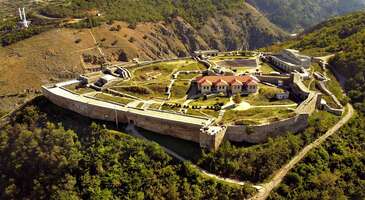 Kosova&rsquo;nın k&uuml;lt&uuml;r başkenti olarak bilinen Prizren, hem tarihi dokusu ve k&uuml;lt&uuml;rel zenginlikleri hem de doğal g&uuml;zellikleriyle Balkanlar'ın en g&ouml;zde şehirlerinden biri. Kosova'nın incisi olarak her k&ouml;şesinde Osmanlı'nın izlerini taşıyan şehirde tarihi camiler, kiliseler, k&ouml;pr&uuml;ler ve kalelerle adeta bir a&ccedil;ık hava m&uuml;zesinde geziyor gibi hissedeceksin.&nbsp; Bistri&ccedil;a Nehri'nin ikiye b&ouml;ld&uuml;ğ&uuml; Prizren, otantik dokusu ve huzurlu atmosferiyle de b&uuml;y&uuml;leyen bir atmosfere sahip. Her yıl binlerce turisti ağırlayan Prizren, tarih, doğa ve lezzet dolu bir gezi planı isteyenler i&ccedil;in g&uuml;zel bir adres.&nbsp; Prizren&rsquo;in neyi meşhur? Prizren, &ouml;zellikle tarihi ve doğal g&uuml;zellikleriyle &uuml;nl&uuml;. Osmanlı d&ouml;neminden kalma camiler, hamamlar, taş k&ouml;pr&uuml;ler ve dar sokaklar, Prizren&rsquo;e otantik bir hava katarken, &ouml;zellikle Şadırvan Meydanı, Prizren&rsquo;in kalbi olarak turistlerin en &ccedil;ok ziyaret ettiği yerlerden biri. Şehrin simgelerinden olan Prizren Kalesi, b&uuml;y&uuml;leyici manzarasıyla &uuml;nl&uuml;. Her yıl d&uuml;zenlenen Dokufest Belgesel Film Festivali ise Prizren&rsquo;i k&uuml;lt&uuml;r ve sanat tutkunları i&ccedil;in sevilen bir merkez haline getiriyor.&nbsp; Prizren&rsquo;e ne zaman gidilir? Prizren, yılın her d&ouml;neminde ziyaret edilebilecek bir destinasyon olsa da en ideal zamanlar, bahar ve yaz ayları. Nisan ile ekim arasındaki d&ouml;nem, Prizren&rsquo;in tarihi sokaklarını keşfetmek, Şadırvan Meydanı&rsquo;nda vakit ge&ccedil;irmek ve Prizren Kalesi&rsquo;nden muhteşem manzaraları izlemek i&ccedil;in en uygun zamanlar. Bu d&ouml;nemde hava genellikle ılık ve g&uuml;neşli, bu da a&ccedil;ık hava etkinlikleri i&ccedil;in ideal bir ortam sunuyor. Ayrıca her yıl ağustos ayında d&uuml;zenlenen ve uluslararası &uuml;ne sahip Dokufest Belgesel Film Festivali de Prizren&rsquo;i ziyaret etmek i&ccedil;in harika bir fırsat. Kış aylarında ise şehir, daha sakin bir atmosfere b&uuml;r&uuml;n&uuml;yor ve karlı dağlarıyla b&uuml;y&uuml;leyici manzaralar sunuyor. Prizren&rsquo;de ne yenir? Prizren, zengin mutfağıyla biliniyor ve Osmanlı, Arnavut, Balkan mutfaklarının etkilerini taşıyor. Şehirde &ouml;zellikle k&ouml;fte, kebap ve et yemekleri &ccedil;ok &uuml;nl&uuml;. Prizren&rsquo;in en pop&uuml;ler lezzetlerinden olan fliya, kat kat hazırlanmış ve &ouml;zel bir pişirme y&ouml;ntemiyle yapılan geleneksel bir hamur işi. Yerel restoranlarda sunulan pide &ccedil;eşitleri ve tava yemeklerini de mutlaka denemelisin. Prizren&rsquo;in meşhur tatlılarından biri olan trile&ccedil;e, s&uuml;t ve karamelin m&uuml;kemmel uyumunu sunuyor.&nbsp; 1. Prizren Kalesi Kosova&rsquo;nın k&uuml;lt&uuml;rel mirasının en &ouml;nemli sembollerinden olan Prizren Kalesi, tarihi ve etkileyici yapısıyla Prizren&rsquo;e hakim bir tepede y&uuml;kseliyor. Kaleden şehrin panoramik manzarasını izleyerek unutulmaz bir deneyim yaşayabilirsin. &Ouml;zellikle g&uuml;n batımında Prizren&rsquo;in tarihi taş k&ouml;pr&uuml;leri, camileri ve kiliseleriyle s&uuml;sl&uuml; manzara, adeta bir tabloyu andırıyor. Osmanlı d&ouml;neminde &ouml;nemli bir savunma noktası olan Prizren Kalesi, Roma ve Bizans d&ouml;nemlerine kadar uzanan zengin bir ge&ccedil;mişe sahip. Y&uuml;zyıllar boyunca bir&ccedil;ok medeniyete ev sahipliği yapan kale, g&uuml;n&uuml;m&uuml;zde Kosova&rsquo;nın &ccedil;ok k&uuml;lt&uuml;rl&uuml; tarihine ışık tutuyor. Prizren Kalesi&rsquo;ni ziyaret ederek, &uuml;lkenin ge&ccedil;mişine dair derin bir yolculuğa &ccedil;ıkabilirsin. Kalenin i&ccedil;indeki kazı alanları ve tarihi surlar da ge&ccedil;mişin izlerini hala korumaya devam ediyor. Aynı zamanda kale, şehrin en pop&uuml;ler turistik noktalarından biri ve kaleye ulaşmak i&ccedil;in kısa bir y&uuml;r&uuml;y&uuml;ş yaparak hem doğanın hem de tarihin tadını &ccedil;ıkarabilirsin.&nbsp; Konum Linki 2. Şadırvan Şehir Meydanı Prizren'in tarihi, k&uuml;lt&uuml;rel ve sosyal hayatların merkezi olan Şadırvan Şehir Meydanı, ismini Osmanlı d&ouml;neminde kalma şadırvan &ccedil;eşmesinden alıyor. Şadırvan, g&uuml;n&uuml;m&uuml;zde de hem halkın hem de turistlerin sevdiği buluşma noktalarından biri ve Prizren'in m&uuml;kemmel atmosferini hissetmek i&ccedil;in m&uuml;kemmel bir başlangı&ccedil; ​​noktası.&nbsp; Meydanın &ccedil;evresi, Osmanlı mimarisiyle dikkat &ccedil;eken camiler, hamamlar ve geleneksel yapılarla dolu. Burada dolaşırken tarihe tanıklık edebilir ve her k&ouml;şede g&uuml;zel fotoğraflar &ccedil;ekebilirsin. Şadırvan Şehir Meydanı, Prizren'in zengin k&uuml;lt&uuml;rel mozaiğinin bir simgesi ve hem ge&ccedil;mişin izlerini taşırken hem de modern şehir hayatını yansıtıyor.&nbsp;&nbsp; Konum Linki {insightBoxStart}Yazar Notu: Şadırvan Meydanı &ccedil;evresindeki kafeler ve restoranlarda y&ouml;resel lezzetler tadabilir, hediyelik eşyalar alabilir, &ouml;zellikle akşam saatlerinde canlı atmosferin tadını &ccedil;ıkarabilirsin.{insightBoxEnd} 3. Bistri&ccedil;a Nehri Prizren şehri, Bistri&ccedil;a Nehri ile ikiye b&ouml;l&uuml;n&uuml;yor ve her iki taraf da tarihi dokusu, k&uuml;lt&uuml;rel zenginlikleri ve doğal g&uuml;zellikleriyle keşfedilmeye değer. Bistri&ccedil;a Nehri'nin kıyısında sıralanan tarihi yapılar, Arnavut kaldırımlı sokaklar ve geleneksel evler, sana zamanda keyifli bir yolculuk yapma fırsatı sunacak. Şehrin sembol&uuml; haline gelen Taşk&ouml;pr&uuml;, nehrin iki yakasını birleştirirken tablo g&uuml;zelliğinde manzaralar i&ccedil;in de arka plan oluşturuyor. Prizren Kalesi'nin surlarına &ccedil;ıkarak da Bistri&ccedil;a Nehri'nin her yakasındaki &ccedil;arpıcı manzaraları kuş bakışı izleyebilirsin.&nbsp; Bistri&ccedil;a Nehri, kıyısında sıralanan kafe ve restoranlarda geleneksel Kosova lezzetlerini tadarak dinlendirici bir mola verebilirsin. &Ccedil;evredeki yerel pazarlarda ise el işi &uuml;r&uuml;nler, geleneksel kıyafetler ve y&ouml;resel &uuml;r&uuml;nler alabilirsin. Konum Linki 4. Prizren Saat Kulesi &nbsp; Şehrin tarihi ve k&uuml;lt&uuml;rel a&ccedil;ıdan &ouml;nemli bir simgelerinden olan Prizren Saat Kulesi, Osmanlı d&ouml;nemine ait mirasının en g&uuml;zel &ouml;rneklerinden biri. 19. y&uuml;zyılda inşa edildiği d&uuml;ş&uuml;n&uuml;len saat kulesi, Osmanlı İmparatorluğu&rsquo;nun Balkanlardaki etkisini yansıtan simgesel yapılardan. Şehrin eski &ccedil;arşısına yakın bir konumda y&uuml;kselen Prizren Saat Kulesi, hem halk hem de turistler i&ccedil;in pop&uuml;ler bir buluşma noktası. Saat kulesi, taş ile ahşap malzemelerden yapılmış zarif ve sade mimarisiyle hemen dikkat &ccedil;ekerken, Prizren&rsquo;in tarihi dokusuna da uyum sağlıyor.&nbsp; Prizren Saat Kulesi, g&uuml;zel konumuyla şehri keşfetmek i&ccedil;in ideal bir başlangı&ccedil; noktası. &Ccedil;evredeki tarihi camiler, taş k&ouml;pr&uuml;ler ve &ccedil;arşıları dolaşarak Prizren&rsquo;in b&uuml;y&uuml;leyici atmosferini tam olarak hissedebilirsin.&nbsp;Prizren Saat Kulesi, şehrin tarihine ışık tutan &ouml;nemli bir sembol olmasının yanı sıra k&uuml;lt&uuml;rel bir miras olarak da &ouml;zenle korunuyor.&nbsp; Konum Linki 5. Taşk&ouml;pr&uuml; Prizren Taşk&ouml;pr&uuml;, şehrin en ikonik yapılarından biri olarak tarih ve estetiğin m&uuml;kemmel bir birleşimini yansıtıyor. Osmanlı d&ouml;neminde inşa edilen tarihi k&ouml;pr&uuml;, Bistri&ccedil;a Nehri &uuml;zerinde yer alıyor ve Prizren&rsquo;in eski &ccedil;arşısını diğer b&ouml;lgelere bağlayan &ouml;nemli bir ge&ccedil;iş noktası. Taşk&ouml;pr&uuml;, sadeliği ve zarafetiyle Osmanlı m&uuml;hendisliğinin klasik &ouml;rneklerinden biri olarak kabul ediliyor. &Uuml;&ccedil; kemerli yapısıyla dikkat &ccedil;eken k&ouml;pr&uuml;, hem dayanıklılığı hem de estetik uyumuyla &uuml;nl&uuml;. Tarihi boyunca birka&ccedil; kez restore edilen Taşk&ouml;pr&uuml;, orijinal dokusunu koruyarak g&uuml;n&uuml;m&uuml;ze kadar ulaşmış. Taşk&ouml;pr&uuml;, aynı zamanda Prizren&rsquo;in k&uuml;lt&uuml;rel ve sosyal yaşamının &ouml;nemli bir par&ccedil;ası. K&ouml;pr&uuml;, halkın yanı sıra turistler i&ccedil;in de pop&uuml;ler bir buluşma noktası ve &ouml;zellikle g&uuml;n batımında k&ouml;pr&uuml;den Prizren&rsquo;in taş sokaklarına ve &ccedil;evredeki tarihi yapıları izlemek, &ccedil;ok sevilen bir etkinlik. K&ouml;pr&uuml;n&uuml;n hemen yanı başındaki mekanlarda oturup Bistri&ccedil;a Nehri&rsquo;nin huzur veren sesi eşliğinde kahve i&ccedil;erek Prizren&rsquo;in tadını &ccedil;ıkarabilirsin. Konum Linki {insightBoxStart}İpucu: ENUYGUN&rsquo;dan kolayca u&ccedil;ak bileti alabilir, dilediğin yeri uygun fiyatlarla keşfedebilirsin. Şimdi seyahatinin ilk adımı olan Kosova u&ccedil;ak bileti almak i&ccedil;in tıkla.{insightBoxEnd} {flight_search_form_banner} 6. Sinan Paşa Camii Prizren&rsquo;ın en &ccedil;ok ziyaret edilen tarihi yapılarından olan Sinan Paşa Camii, Osmanlı d&ouml;neminden kalma en g&ouml;rkemli mimari eserlerden. Prizren&rsquo;in tarihi ve k&uuml;lt&uuml;rel dokusunun &ouml;nemli bir par&ccedil;ası olan cami, 1615 yılında Osmanlı veziri Sinan Paşa tarafından yaptırılmış. Sinan Paşa Camii, mimari zarafeti ve detaylı s&uuml;slemeleriyle seni b&uuml;y&uuml;leyecek g&uuml;zellikte. Prizren&rsquo;in tam merkezinde hemen dikkat &ccedil;eken cami, Mimar Sinan ekol&uuml;n&uuml; yansıtan klasik Osmanlı mimarisinin en g&uuml;zel &ouml;rneklerinden. B&uuml;y&uuml;k bir kubbeye ve ince bir minareye sahip olan cami, aynı zamanda i&ccedil; mek&acirc;nındaki zarif kalem işleri ve fresklerle de g&ouml;r&uuml;lmeye değer. Avlusunda &ccedil;evredeki tarihi yapıları ve Şar Dağları&rsquo;nın muhteşem manzarasını seyrederek dinlenebileceğin Sinan Paşa Camii listende olmalı.&nbsp; Konum Linki {insightBoxStart}Yazar Notu: Sinan Paşa Camii&rsquo;nin &ccedil;evresinde Osmanlı mutfağından lezzetler tadabileceğin k&uuml;&ccedil;&uuml;k restoranlara da mutlaka uğramalısın.{insightBoxEnd} 7. Şar Dağları Milli Parkı Kosova&rsquo;nın doğal g&uuml;zelliklerinin en dikkat &ccedil;ekici noktalarından biri olan Şar Dağları Milli Parkı, Prizren şehrine yakın konumuyla b&ouml;lgeye gelen turistler i&ccedil;in pop&uuml;ler bir destinasyon. 1986 yılında milli park ilan edilen b&ouml;lge, yaklaşık 39.000 hektarlık bir alanı kapsıyor. Balkanlar&rsquo;ın en etkileyici doğal alanlarından Şar Dağları, hem bitki hem de vahşi yaşam a&ccedil;ısından b&uuml;y&uuml;k bir zenginliğe sahip. Endemik bitkilerini, nadir hayvan t&uuml;rlerini ve muhteşem manzaraları keşfedebileceğin milli park, doğa ve macera tutkunları i&ccedil;in adeta bir cennet. Dağların eteklerinde yer alan yemyeşil ormanlar, berrak nehirler ve g&ouml;ller, aynı zamanda trekking, dağcılık ve fotoğraf&ccedil;ılık gibi aktiviteler i&ccedil;in de eşsiz bir fırsat veriyor. Şar Dağları Milli Parkı, yılın her d&ouml;neminde farklı bir g&uuml;zelliğe sahip. Yaz aylarında doğa y&uuml;r&uuml;y&uuml;şleri ve kamp yapabileceğin Şar Dağları, kış aylarında ise kış sporları i&ccedil;in pop&uuml;ler bir merkez haline geliyor. Milli park, &ouml;zellikle doğal yaşamı keşfetmek isteyenler i&ccedil;in de b&uuml;y&uuml;leyici bir deneyim yaşatıyor, burada ayılar, vaşaklar, kartallar ve bir&ccedil;ok diğer hayat t&uuml;r&uuml;n&uuml; g&ouml;zlemleyebilirsin. Ayrıca parkın i&ccedil;inde yer alan geleneksel k&ouml;yler ve tablo g&uuml;zelliğinde manzaralar da harika fotoğraflar &ccedil;ekme ve b&ouml;lgenin yerel k&uuml;lt&uuml;r&uuml;n&uuml; tanıma şansı veriyor.&nbsp; Konum Linki 8. Cuma Camii Cuma Camii, Prizren&rsquo;deki Osmanlı d&ouml;nemine ait en eski ve en &ouml;nemli dini yapılardan biri olarak kabul ediliyor. 15. y&uuml;zyılda Sultan I. Murad d&ouml;neminde inşa edilen cami, Prizren&rsquo;in tarihi ve k&uuml;lt&uuml;rel dokusunu en iyi yansıtan eserlerden biri olarak g&ouml;r&uuml;lmeye değer. Şehirdeki en b&uuml;y&uuml;k cami olan Cuma Camii, geniş kubbesi, zarif minaresi ve sade Osmanlı mimarisiyle hemen dikkat &ccedil;ekiyor. Caminin i&ccedil; mek&acirc;nında yer alan hat sanatı ve s&uuml;slemeler ise Osmanlı sanatının zarafetini g&ouml;zler &ouml;n&uuml;ne seriyor.&nbsp; Caminin avlusuna adım attığında, huzurlu bir atmosfer eşliğinde şehrin tarihi dokusunu rahat&ccedil;a hissedebilirsin. Osmanlı d&ouml;neminin mimari mirasını keşfetmek, b&ouml;lgenin k&uuml;lt&uuml;rel ve tarihi zenginliklerine tanıklık etmek isteyenler i&ccedil;in Cuma Camii ziyaret edilmesi gereken bir yer.&nbsp; Konum Linki 9.&nbsp; Gazi Mehmet Paşa Camii (Bayraklı Camii) Halk arasında Bayraklı Camii olarak da bilinen Gazi Mehmet Paşa Camii, şehirde Osmanlı d&ouml;neminden g&uuml;n&uuml;m&uuml;ze kalan en &ouml;nemli yapılarından biri. 1561 yılında inşa edilen cami, geleneksel mimarisi ve tarihi atmosferiyle dikkat &ccedil;ekiyor. Caminin i&ccedil; kısmında yer alan ince hat sanatı ve kalem işleri, Osmanlı d&ouml;nemindeki sanat anlayışını incelemek i&ccedil;in ideal. Dış cephedeki taş iş&ccedil;iliği ve camiye eklenmiş olan zarif kubbe de klasik Osmanlı mimarisinin g&uuml;zel &ouml;rneklerinden.&nbsp; Caminin adı olan &ldquo;Bayraklı&rdquo;, uzun yıllar boyunca caminin minaresinde dalgalanan Osmanlı sancağından geliyor ve Kosova'daki Osmanlı etkisinin bir sembol&uuml; olarak g&ouml;steriliyor. Gazi Mehmet Paşa Camii, yanındaki tarihi yapılarla da adeta bir a&ccedil;ık hava m&uuml;zesini andırıyor. Caminin hemen yanında yer alan medrese ve hamam gibi yapılar, Osmanlı d&ouml;neminde caminin yalnızca ibadet değil, aynı zamanda bir eğitim ve sosyal merkez olduğunu anlatıyor. Konum Linki 10. Sveti Spas Kilisesi (Kutsal Kurtarıcı Kilisesi) Prizren'in inan&ccedil; turizmiyle &ccedil;ok ziyaret edilen yerlerinden biri olan Sveti Spas Kilisesi (Kutsal Kurtarıcı Kilisesi), Balkanlardaki Ortodoks Hristiyanlığı i&ccedil;in &ouml;nemli bir merkez. 14. y&uuml;zyılda inşa edilen kilise, Orta &Ccedil;ağ d&ouml;nemi Bizans mimarisi ve dini freskleriyle &ccedil;ok ilgi g&ouml;r&uuml;yor. &Ouml;zellikle fresklerdeki İsa ve aziz tasvirleri, d&ouml;nemin sanatsal ve dini anlayışı hakkında detaylı fikir veriyor. Kilise, Prizren'in kartpostal g&uuml;zelliğinde manzarasıyla uyum i&ccedil;inde, ayrıca taş iş&ccedil;iliği ve sade tasarımıyla huzurlu bir atmosfere sahip.&nbsp; Kilise, Kosova'daki farklı etnik ve dini ge&ccedil;mişlerin bir arada var olduğu k&uuml;lt&uuml;rel mozaiğin bir sembol&uuml; olarak da değerlendiriliyor. Mimari ayrıntılar ve tarihin &ouml;nemiyle Sveti Spas Kilisesi, k&uuml;lt&uuml;r ve tarih meraklıları i&ccedil;in mutlaka uğranması gereken bir yer. Tarihi yapılarla sarılı Sveti Spas Kilisesi, sadece bir ibadet yeri değil, aynı zamanda b&ouml;lgenin tarihi dokusunu &ouml;ğrenmek isteyenler i&ccedil;in eşsiz bir bilgi ve ilham kaynağı.&nbsp; Konum Linki {{campaignsSlider}} 11. Gazi Mehmet Paşa Hamamı Prizren&rsquo;in Osmanlı d&ouml;neminden g&uuml;n&uuml;m&uuml;ze ulaşan en &ouml;nemli tarihi yapılardan biri de Gazi Mehmet Paşa Hamamı. 16. y&uuml;zyılda Kanuni Sultan S&uuml;leyman d&ouml;neminde inşa edilen hamam, Osmanlı mimarisinin zarif &ouml;zelliklerini yansıtıyor. &Ccedil;ifte hamam olarak tasarlanan yapı, kadın ve erkekler i&ccedil;in ayrı b&ouml;l&uuml;mlere sahip. Hamamın kubbeli yapısı, taş ve tuğladan yapılmış detaylarının yanı sıra i&ccedil;erideki suyun akışını d&uuml;zenleyen sistemler de Osmanlı hamam k&uuml;lt&uuml;r&uuml;n&uuml;n inceliklerini g&ouml;zler &ouml;n&uuml;ne seriyor. Bug&uuml;n orijinal işlevini yitirmiş olsa da Gazi Mehmet Paşa Hamamı, tarihi atmosferiyle ziyaret&ccedil;ilerin ilgisini &ccedil;eken bir k&uuml;lt&uuml;rel miras alanı olarak hizmet vermeye devam ediyor. Konum Linki {insightBoxStart}Yazar Notu: Hamam, Prizren&rsquo;in eski &ccedil;arşısına yakın merkezi bir konumda yer alıyor ve &ccedil;evresindeki taş sokaklar ve tarihi yapılarla birlikte şehrin ge&ccedil;mişine dair kapsamlı bir yolculuk yapma şansı veriyor.{insightBoxEnd} &nbsp; 12. Sara&ccedil;hane Halveti Tekkesi Prizren'de Osmanlı d&ouml;neminden g&uuml;n&uuml;m&uuml;ze ulaşan en &ouml;nemli dini ve k&uuml;lt&uuml;rel yapılardan biri de Sara&ccedil;hane Halveti Tekkesi. 16. y&uuml;zyılda Halveti tarikatına mensup dervişlerin ibadet ve eğitim merkezi olarak inşa edilen tekke, mimari sadeliği ve manevi atmosferiyle hala &ccedil;ok ilgi g&ouml;r&uuml;yor. Sara&ccedil;hane b&ouml;lgesindeki tekke, Halvetilik geleneğini ve Osmanlı d&ouml;nemindeki tasavvuf k&uuml;lt&uuml;r&uuml;n&uuml; yansıtan &ouml;nemli bir sembol. Tekkenin i&ccedil; kısmında yer alan ibadet alanı ve zarif iş&ccedil;ilikle yapılan ahşap detaylar, Osmanlı d&ouml;nemindeki sanat ve dini yaşam anlayışını net bir şekilde yansıtıyor. Tasavvufa ilgi duyanlar ve Osmanlı k&uuml;lt&uuml;rel mirasını bırakmak isteyenler i&ccedil;in Sara&ccedil;hane Halveti Tekkesi, &ouml;nemli bir nokta. Konum Linki {insightBoxStart}Yazar Notu: Sara&ccedil;hane Halveti Tekkesi, g&uuml;n&uuml;m&uuml;zde hem halk hem de turistlerin &ccedil;ok ilgisini &ccedil;eken tasavvuf m&uuml;ziği dinletileri gibi etkinliklere ev sahipliği yapıyor.{insightBoxEnd} 13. Arasta Camii Prizren'de gezebileceğin başka bir Osmanlı d&ouml;nemi yapısı da 16. y&uuml;zyılda inşa edilen Arasta Camii. Cami, adını Osmanlı d&ouml;neminde ticaretin kalbinin attığı arasta &ccedil;arşısından alıyor. Caminin sade ancak etkileyici mimarisi, Osmanlı cami mimarisinin g&uuml;zel bir &ouml;rneği. &Ouml;zellikle taş iş&ccedil;iliği ve kubbe, d&ouml;nemin estetik anlayışını yansıtırken, caminin i&ccedil; kısmındaki ince hat sanatı &ouml;rnekleri de g&ouml;r&uuml;lmeye değer. Arasta Camii, Osmanlı d&ouml;neminde hem ibadet hem de sosyal yaşam merkeziydi ve Prizren'in k&uuml;lt&uuml;rel hayatına &ouml;nemli bir katkı sağlıyordu. Prizren'in tarihi şehir merkezindeki Arasta Camii, taş d&ouml;şeli dar sokaklar ve diğer Osmanlı eserleriyle sarılı olduğu i&ccedil;in gezi sırasında huzurlu bir mola vermek i&ccedil;in de g&uuml;zel bir adres. Konum Linki 14. M&uuml;derris Ali Efendi Camii Prizren şehri, Osmanlı d&ouml;nemine ait bir&ccedil;ok mimari esere ev sahipliği yapıyor ve bu eserlerden biri de M&uuml;derris Ali Efendi Camii. 1581 yılında inşa edildiği d&uuml;ş&uuml;n&uuml;len cami, Osmanlı mimarisinin klasik bir &ouml;rneği. Şehir merkezindeki hareketli Şadırvan Meydanı&rsquo;na &ccedil;ok yakın olan cami, g&uuml;zel konumuyla hem yerli hem de yabancı turistlerin ilgisini &ccedil;ekiyor.&nbsp; &Ouml;zellikle sade ama etkileyici taş iş&ccedil;iliği ve minaresi ile dikkat &ccedil;eken cami, ibadethane olmasının yanı sıra b&ouml;lgenin tarihine ışık tutan &ouml;nemli bir simge. M&uuml;derris Ali Efendi Camii&rsquo;nin i&ccedil; kısmı, Osmanlı d&ouml;nemi s&uuml;sleme sanatının bir &ouml;rneği olan kalem işleriyle bezenmiş. Cami, sadece klasik mimarisiyle değil, aynı zamanda huzurlu atmosferiyle de dinlenmek i&ccedil;in g&uuml;zel bir se&ccedil;enek. Konum Linki 15. Emin Paşa Camii&nbsp; Emin Paşa Camii, Osmanlı'ya ait zarif mimarisiyle Prizren&rsquo;in en dikkat &ccedil;ekici yapılarından biri. 1831 yılında inşa edilen cami, Osmanlı mimari geleneğinin son d&ouml;nem eserlerinden biri olarak &ouml;ne &ccedil;ıkıyor. Caminin sade ama estetik dış cephesi, ince iş&ccedil;iliğiyle bezenmiş taş duvarları ve zarif minaresi, Osmanlı d&ouml;neminin mimari anlayışını yansıtıyor. &Ouml;zellikle caminin i&ccedil; kısmında yer alan hat sanatı ve s&uuml;slemeler, d&ouml;nemin sanatıyla uyumlu. Emin Paşa Camii, sadece bir ibadet yeri değil, aynı zamanda Osmanlı cami mimarisinin g&uuml;zel bir &ouml;rneği olarak da tarih ve k&uuml;lt&uuml;r meraklılarının &ccedil;ok ilgisini &ccedil;ekiyor.&nbsp; Konum Linki {insightBoxStart}Yazar Notu:&nbsp;Emin Paşa Camii'nin bulunduğu b&ouml;lge de taş d&ouml;şeli dar sokakları, geleneksel evleri ve tarihi yapılarıyla adeta bir a&ccedil;ık hava m&uuml;zesini andırıyor.{insightBoxEnd} 16. Kutsal Başmelekler Manastırı Prizren'in yaklaşık 3 kilometre dışındaki Kutsal Başmelekler Manastırı, Bistri&ccedil;a Nehri'nin kıyısında &ccedil;arpıcı bir manzara sunuyor. 14. y&uuml;zyılda inşa edilen manastır, Orta &Ccedil;ağ Balkan mimarisinin en &ouml;nemli &ouml;rneklerinden biri olarak g&ouml;steriliyor. Bir zamanlar Sırp Ortodoks Kilisesi'nin en b&uuml;y&uuml;k dini yapılarından olan manastır, mimari kadar tarihiyle de dikkat &ccedil;ekiyor. Manastırın taş duvarları, Bizans ve Sırp mimarilerini harmanlayan etkileyici bir estetik sunarken, b&ouml;lgenin doğal g&uuml;zellikleri, bu tarihi yapıya m&uuml;kemmel bir atmosfer katıyor.&nbsp; Kutsal Başmelekler Manastırı&rsquo;nı Bistri&ccedil;a Nehri'nin muhteşem manzarası eşliğinde keşfedilebilir ve &ccedil;evredeki dağların tablo g&uuml;zelliğinde fotoğraflarını &ccedil;ekebilirsin. Manastır, y&uuml;zyıllar boyunca bir&ccedil;ok değişime uğrasa da hala b&ouml;lgedeki k&uuml;lt&uuml;rel ve dini oluşumların &ouml;nemli bir sembol&uuml;. Tarih, sanat ve doğayı bir arada deneyimlemek isteyen dinlemek i&ccedil;in Kutsal Başmelekler Manastırı, g&uuml;zel bir se&ccedil;enek. Konum Linki Prizren ile birlikte &uuml;lkenin farklı keşif duraklarını gezmek istersen Kosova&rsquo;da gezilecek yerler yazımıza g&ouml;z atabilirsin.