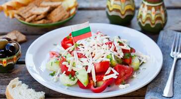 Bazen bir sokak &ouml;tede &ccedil;ocukluğumuzdaki o pazar kahvaltılarının kokusunu buluruz ya işte Bulgaristan da sınırın &ouml;tesinde olmasına rağmen o tanıdık sofraların unutulmaz lezzetleriyle buluşmanı sağlayacak &uuml;lkelerden biri. Tarih&icirc; ve doğal g&uuml;zelliklerin yanı sıra birbirinden lezzetli yemeklere ev sahipliği yapan Bulgaristan, mutfağıyla da b&uuml;y&uuml;k beğeni topluyor. Balkan mutfağının en karakteristik duraklarından biri olan Bulgaristan &lsquo;da, Osmanlı, Balkan ve Slav mutfaklarının izlerini g&ouml;rebilirsin. Et, yoğurt, sebze ve hamur işlerinin &ouml;n planda olduğu Bulgar mutfağında sade ama lezzetli tariflere rastlamak m&uuml;mk&uuml;n. Mevsimsel &uuml;r&uuml;nlerin, ev yapımı tatların ve doyurucu porsiyonlarıyla dikkat &ccedil;eken Bulgar mutfağının sevilen lezzetlerini bir araya getirdik. Hadi birlikte keşfedelim. 1. Banitsa Bulgaristan&rsquo;ın en meşhur hamur işlerinden biri olan banitsa, incecik a&ccedil;ılmış yufkaların arasına beyaz peynir ve yumurta karışımı eklenerek hazırlanıyor. Bazı versiyonlarında ıspanak, pırasa ya da kıyma da kullanılabilen bu lezzet genellikle kahvaltıda t&uuml;ketiliyor. Fakat g&uuml;n&uuml;n her saatinde bulabilirsin. Fırından yeni &ccedil;ıkmış, dışı &ccedil;ıtır, i&ccedil;i yumuşak banitsanın enfes tadına doyamayacaksın. 2. Kebapche Geleneksel bir Bulgar yemeği olan kebapche, g&ouml;r&uuml;n&uuml;m olarak k&ouml;fteyi andırsa da baharat karışımı olarak bildiğimiz k&ouml;ftelerden ayrışıyor. Kıyma, kimyon, karabiber ve sarımsakla yoğrularak mangalda pişirilen bu lezzet, genellikle patates kızartması, ekmek ve yoğurt bazlı soslarla servis ediliyor. Mangalın isli kokusu ve yanında k&ouml;zlenmiş biberlerle enfes bir &ouml;ğ&uuml;n olan kebapche, Bulgaristan&rsquo;ın sokak lezzetleri arasında da olduk&ccedil;a pop&uuml;ler. 3. Shopska salata Bulgar mutfağının en bilinen lezzetlerinden olan shopska salata, domates, salatalık, biber ve soğanın &uuml;zerine rendelenmiş beyaz peynir ile hazırlanıyor. Zeytinyağı ve sirke ile tatlandırılan bu salata, Bulgaristan&rsquo;da &ccedil;ok sık t&uuml;ketiliyor. Hafif yapısı ile b&uuml;y&uuml;k beğeni toplayan shopska salata, &ouml;zellikle et yemeklerinin yanında sık&ccedil;a tercih ediliyor. 4. Kyufte Kebapcheye benzeyen fakat daha yuvarlak bir forma sahip olan kyufte, Bulgaristan&rsquo;da sık&ccedil;a t&uuml;ketilen bir k&ouml;fte &ccedil;eşidi. Izgara ya da tavada pişirilerek sunulan bu lezzete, hem evlerin hem de restoranların men&uuml;lerinden eksik olmuyor. {insightBoxStart}İpucu: Bu sofrada sen de bir sandalyen olsun istersen, en konforlu konaklama se&ccedil;enekleri i&ccedil;in biz hep buradayız. Birlikte planlamak i&ccedil;in ENUYGUN'da Bulgaristan otelleri araştırmasına başlayabilirsin.{insightBoxEnd} {hotel_search_form_banner} 5. Tarator &Ouml;zellikle yaz aylarında tercih edilen soğuk bir &ccedil;orba &ccedil;eşidi olan tarator, yoğurt, salatalık, ceviz, sarımsak ve dereotu ile hazırlanıyor. Ferah bir tada sahip olan bu &ccedil;orba, yaz aylarının sıcak g&uuml;nlerinde sık&ccedil;a t&uuml;ketiliyor. T&uuml;rk cacığını andıran tarator, i&ccedil;indeki ceviz ile kendine has bir aromaya sahip olarak cacıktan ayrışıyor. Sence hangisi daha ferah? İ&ccedil;indeki ceviz, dengeleri değiştirebilir, bizden s&ouml;ylemesi. 6. Sarmi Lahana veya asma yaprağıyla yapılan sarmi, pirin&ccedil;li ve etli bir har&ccedil;tan oluşuyor. Lezzet ve g&ouml;r&uuml;nt&uuml; olarak bildiğimiz yaprak ve lahana sarmasına benzeyen sarmi, yoğurt ile servis ediliyor. 7. Musaka (Bulgar usul&uuml;) Yunan versiyonundan farklı olarak patates ağırlıklı olan Bulgar musakası, kat kat patates ve kıyma dizilerek hazırlanıyor. Fırından aldıktan sonra yoğurt ve yumurtayla hazırlanan sos eklenerek servis edilen musaka, Bulgaristan&rsquo;da &ouml;zellikle ev yemekleri sunan restoranlarda sık&ccedil;a bulunuyor. 8. Shkembe chorba İşkembe &ccedil;orbasının Bulgar mutfağındaki karşılığı olan shkembe chorba, sarımsak, sirke ve kırmızı biberle tatlandırılıyor. T&uuml;rkiye&rsquo;de olduğu gibi &ouml;zellikle gece ge&ccedil; saatlerde ya da soğuk havalarda tercih edilen bu geleneksel &ccedil;orbayı Bulgaristan seyahatinde mutlaka denemelisin. 9. Meshana skara Karışık ızgara anlamına gelen meshana skara, kebapche, kyufte, sucuk benzeri kırmızı etlerin ve bazen de tavuk etinin bir arada servis edildiği yemek t&uuml;r&uuml;. &Ouml;zellikle et severler i&ccedil;in g&ouml;z doyurucu bir yemek olan meshana skarayı, Bulgaristan&rsquo;da bir&ccedil;ok restoranda bulabilirsin. 10. Airyan Bulgaristan&rsquo;da yaygın olarak t&uuml;ketilen i&ccedil;ecekler arasında yer alan airyan (ayran), &ouml;zellikle yoğurdun kaliteli olmasıyla birlikte olduk&ccedil;a lezzetli. Et yemeklerinin yanında sık&ccedil;a t&uuml;ketilen bir i&ccedil;ecek olan ayranı, hemen her yerde bulman m&uuml;mk&uuml;n. {{campaignsSlider}} 11. Boza &Uuml;lkemizde sevilerek t&uuml;ketilen i&ccedil;eceklerden biri olan boza, Bulgaristan&rsquo;da da yaygın. Kıvamlı ve hafif tatlı yapısıyla fermente bir i&ccedil;ecek olan boza, &ouml;zellikle kış aylarında bolca t&uuml;ketiliyor. 12. Rakia Bulgaristan&rsquo;ın en bilinen alkoll&uuml; i&ccedil;eceği olan rakia, &uuml;z&uuml;m, erik ve kayısı gibi meyvelerden &uuml;retiliyor. Genellikle yemek &ouml;ncesi aperatif olarak t&uuml;ketilen bu i&ccedil;ecek Bulgar sofralarının vazge&ccedil;ilmezleri arasında yer alıyor. 13. Bulgar şarapları Bu toprakların binlerce yıllık sırlarından biri olan mavrud &uuml;z&uuml;m&uuml;, d&uuml;nyanın belki de başka hi&ccedil;bir yerinde bulamayacağın şaraplara hayat veriyor. K&ouml;kl&uuml; bir şarap &uuml;retim geleneğine sahip olan Bulgaristan, &ouml;zellikle kırmızı şaraplarıyla biliniyor. Yerel &uuml;z&uuml;m &ccedil;eşitlerinden &uuml;retilen bu şaraplar, hem kaliteli hem de uygun fiyatlı olması nedeniyle ilgi g&ouml;r&uuml;yor. G&uuml;zelce doyduysak, şimdi gezme zamanı. Bulgaristan&rsquo;ın birbirinden g&uuml;zel lezzetlerini en g&uuml;zel mek&acirc;nlarda denemek ve keyifli bir keşfe &ccedil;ıkmak i&ccedil;in Bulgaristan&rsquo;da gezilecek yerler yazımıza g&ouml;z atabilirsin.