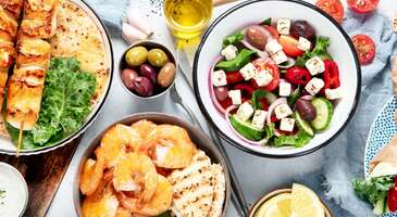 Tarih&icirc; ve doğal g&uuml;zellikleriyle Yunanistan&rsquo;ın en g&uuml;zel sahil şehirlerinden biri olan Kavala, mutfağıyla da dikkat &ccedil;ekiyor. Ege ve Balkan mutfağından lezzetlerin bir arada sunulduğu Kavala mutfağında, deniz &uuml;r&uuml;nlerinden hamur işlerine, sokak lezzetlerinden geleneksel tatlılara kadar bir&ccedil;ok &uuml;r&uuml;n&uuml; g&ouml;rmek m&uuml;mk&uuml;n. Bu nedenle Kavala&rsquo;ya adım attığın anda hissedeceğin duygu yabancılık değil, yıllardır g&ouml;rmediğin bir dostunun sofrasına oturacakmışsın gibi aşina bir duygu olacak. Yunan mutfağının tipik Ege tatlarını bir araya getiren Kavala mutfağı, Osmanlı d&ouml;neminin izlerini de taşıyor. Deniz &uuml;r&uuml;nleri, zeytinyağlılar, hamur işleri ve taze sebzelerden oluşan bu zengin mutfakta T&uuml;rkiye&rsquo;den g&ouml;&ccedil; eden toplulukların etkisiyle tanıdık lezzetlere de rastlayabilirsin. Kavala&rsquo;nın tarih&icirc; ve doğal g&uuml;zelliklerini gezdikten sonra keyifli bir lezzet turuna &ccedil;ıkmayı planlıyorsan şehrin en &ouml;nemli yemeklerini senin i&ccedil;in bir araya getirdik. Hadi Kavala&rsquo;da mutlaka denemen gereken lezzetleri birlikte keşfedelim. 1. Kavala kurabiyesi Kavala denince aklına ilk Kavala kurabiyesi geldiğini biliyoruz. Badem, tereyağı ve bol pudra şekeri ile yapılan bu kurabiye, ağızda dağılan yapısıyla hayranlık uyandırıyor. Şehrin genelinde hemen her pastanede taze olarak bulabileceğin Kavala kurabiyesini sevdiklerine hediye olarak da g&ouml;t&uuml;rebilirsin. Kavala&rsquo;nın dar sokaklarında gezerken burnuna gelen o taze badem ve pudra şekeri kokusu, &ccedil;ocukluğundaki bayram sabahlarını hatırlatacak. Peki kavala kurabiyesinin o eşsiz lezzetinin ardındaki sırrın, ustaların kuşaklar boyu sakladığı fırın ateşi derecesinde olduğunu daha &ouml;nce duymuş muydun? 2. Gouna Yunan mutfağının tipik lezzetlerine rastlayacağın Kavala mutfağında, deniz &uuml;r&uuml;nlerine &ccedil;ok&ccedil;a yer veriliyor. G&uuml;neşte kurutulmuş uskumrunun ızgarada pişirilmesiyle yapılan gouna, Kavala&rsquo;nın meşhur lezzetleri arasında yer alıyor. Lezzetiyle deneyen herkesi kendine hayran bırakan bu lezzeti mutlaka denemelisin. 3. Midyeli pilav Deniz &uuml;r&uuml;nleri denince Kavala&rsquo;ya gittiğinde denemen gereken bir diğer lezzet de midyeli pilav. Midye, pirin&ccedil;, soğan, rendelenmiş domates ve dereotunun bir araya gelmesiyle oluşan bu yemeği, şehrin genelinde bir&ccedil;ok restoranda bulabilirsin. 4. Saganaki Kızartılmış peynir olarak bilinen saganaki, Kavala mutfağının vazge&ccedil;ilmez lezzetleri arasında yer alıyor. &Ouml;zellikle deniz kenarında bulunan tavernalarda sık&ccedil;a servis edilen bu meze, karidesli ve midye &ccedil;eşitleriyle de biliniyor. Peynir, kaşar peyniri, domates, yeşil biber, kekik ve zeytinyağıyla yapılan karidesli saganakiyi de mutlaka denemeni &ouml;neriyoruz. 5. Gyros Yunan mutfağının en bilinen sokak lezzetleri arasında yer alan gyros, Kavala&rsquo;da da yaygın olarak yapılıyor. Tavuk ya da domuz etiyle hazırlanan bu yemek, patates kızartması, pita ekmeği, soğan ve caciki sosuyla servis ediliyor. Hızlı ve doyurucu olan gyros lezzetli alternatifler arasında yer alıyor. 6. Soutzoukakia Baharatla hazırlanan k&ouml;ftelerin domates sosuyla pişirilmesi sonucu ortaya &ccedil;ıkan soutzoukakia, Kavala mutfağının en sevilen lezzetleri arasında yer alıyor. Pilav veya patatesle servis edilen bu yemek, doyurucu olmasıyla da dikkat &ccedil;ekiyor. 7. Kalamar dolması Deniz &uuml;r&uuml;nlerine sık&ccedil;a rastladığımız Kavala mutfağında bir diğer beğenilen lezzet de kalamar dolması. Hemen her mevsim bulabileceğin bu yemek, &ouml;zellikle yaz aylarında sık&ccedil;a tercih ediliyor. Kalamar, zeytinyağı, domates ve sarımsak ile yapılan bu lezzeti mutlaka denemeni &ouml;neriyoruz. 8. Kalamar tava Kavala mutfağının yıldızlarından biri olan kalamar tava, kesinlikle denemen gereken lezzetler arasında yer alıyor. Dışı &ccedil;ıtır, i&ccedil;i yumuşacık olan bu lezzet, hemen her restoranda bulabileceğin yemeklerden. Enfes lezzetiyle deneyen herkesin hafızasında yer edinen kalamar tava, yanında servis edilen limonun taze kokusuyla birlikte Ege&rsquo;nin t&uuml;m enerjisini hissettiriyor. Bu lezzeti denemeden Kavala&rsquo;dan ayrılmamanı &ouml;neririz. 9. Koulouri Kavala&rsquo;da, &ouml;zellikle sabahın erken saatlerinde kahvaltılık olarak yiyebileceğin bir lezzet var ki &ccedil;ok tanıdık gelecek. &Uuml;lkemizde &ccedil;ok&ccedil;a sevilen lezzetlerden biri olan simite, Kavala&rsquo;da da rastlayacaksın. Koulouri adı verilen bu simitler, g&ouml;r&uuml;n&uuml;m ve lezzet olarak bizim simitlerimize olduk&ccedil;a benziyor. 10. Kardydaki Glyko Kavala&rsquo;da yetişen cevizlerden yapılan bir tatlı &ccedil;eşidi olan kardydaki glyko, mutlaka denenmesi gereken lezzetler arasında yer alıyor. Ceviz re&ccedil;eli olarak tanımlayabileceğimiz bu lezzet, g&ouml;r&uuml;nt&uuml; olarak da re&ccedil;eli andırıyor. {{campaignsSlider}} 11. Feta peyniri G&ouml;r&uuml;nt&uuml;s&uuml;yle beyaz peyniri andıran feta peyniri, Kavala&rsquo;nın en sevilen lezzetleri arasında yer alıyor. Koyun ve ke&ccedil;i gibi k&uuml;&ccedil;&uuml;kbaş hayvanların s&uuml;t&uuml;nden elde edilen ve tuzlu, hafif ekşimsi bir aromaya sahip olan bu peynir, salamurda olgunlaşıyor. Genellikle salatalarda kullanılan feta peynirini mutlaka denemelisin. 12. Fava Ana malzemesi sarı bezelye olan fava, &ouml;zellikle balık men&uuml;lerinin olmazsa olmazı. Kekik, zeytinyağı ve soğan gibi malzemelerle yapılan bu lezzet, Kavala seyahatinde mutlaka denemen gereken lezzetler arasında yer alıyor. 13. Caciki İsim olarak bildiğimiz cacıkı andırsa da hazırlama y&ouml;ntemi ve tat olarak farklılaşan caciki, Kavala&rsquo;nın vazge&ccedil;ilmez mezeleri arasında yer alıyor. Cacıktan farklı olarak i&ccedil;ine su ilave edilmeyen bu lezzet, salatalık, yoğurt, sarımsak ve &uuml;zerine hafif zeytinyağı gezdirilerek hazırlanıyor. Kaşığı daldırdığında yoğun kıvamın i&ccedil;inden gelen sızma zeytinyağının ve sarımsağın keskin ve taze kokusu iştahını a&ccedil;acak. 14. Yunan salatası Kavala&rsquo;da, &ouml;zellikle restoranlarda sık&ccedil;a karşılaşacağın mezelerden biri olan Yunan salatası, enfes lezzetiyle dikkat &ccedil;ekiyor. Akdeniz yeşillikleri ve Yunanistan&rsquo;ın meşhur zeytinyağı ile hazırlanan bu salatayı mutlaka denemen gerekiyor. 15. Loukoumades Hamurların kızartılarak bal veya şerbetle servis edilmesiyle meydana gelen loukoumades, Kavala&rsquo;nın en sevilen tatlıları arasında yer alıyor. Bazı yerlerde &ccedil;ikolata ve tar&ccedil;ınla da sunulan bu tatlı, &uuml;lkemizdeki lokum tatlısını andırıyor. 16. Yunan kahvesi Kavala seyahatin sırasında hemen her kafede karşılaşacağın lezzetler arasında yer alan Yunan kahvesi, k&ouml;p&uuml;kl&uuml;, orta veya şekersiz olarak servis ediliyor. Bu y&ouml;n&uuml;yle T&uuml;rk kahvesine olduk&ccedil;a benziyor. {insightBoxStart}İpucu: Kavala&rsquo;nın sıcak sofralarında senin i&ccedil;in de bir sandalye &ccedil;ekmemizi istersen en iyi otel fiyatlarını tek bir yerde g&ouml;rmek, se&ccedil;eceğin otel hakkında bilgi almak ve saniyeler i&ccedil;inde rezervasyon yapmak i&ccedil;in ENUYGUN'da Kavala otelleri araştırmasına başlayabilirsin.{insightBoxEnd} {hotel_search_form_banner} 17. Frappe Kavala&rsquo;da ilk akla gelen soğuk i&ccedil;eceklerden biri olan frappe, &ouml;zellikle yaz aylarında sık&ccedil;a t&uuml;ketiliyor. Bardaktaki buzların birbirine &ccedil;arparken &ccedil;ıkardığı o ses, daha da serinlemeni sağlayacak. Arkadaşlarınla Kavala sahilinde otururken keyifle yudumlayacağın bu lezzet, seyahatin boyunca elinden d&uuml;şmeyecek.&nbsp; 18. Ouzo Yunanistan&rsquo;ın meşhur anasonlu i&ccedil;eceği ouzo, Kavala&rsquo;da da yaygın olarak t&uuml;ketiliyor. Genellikle deniz &uuml;r&uuml;nleri ve mezelerle t&uuml;ketilen bu i&ccedil;eceği, deniz kenarında bulunan tavernaların &ccedil;oğunda deneyebilirsin. Bazı tavernalarda ouzo&rsquo;nun yanına sadece tek bir buz koyulduğunu g&ouml;rebilirsin. Bu hareket, sohbetin ve lezzetin ısınmasına izin vermeyen yerel bir nezaket olarak biliniyor. Kavala&rsquo;da yemek fiyatları, genel olarak Yunanistan ortalamasına yakın ilerliyor. Sokak lezzetleri ve gyros gibi &uuml;r&uuml;nlerin, deniz kenarındaki tavernalarda servis edilen balık ve deniz &uuml;r&uuml;nlerine g&ouml;re daha uygun fiyatlı olduğunu s&ouml;yleyebiliriz. Yemekler genellikle doyurucu porsiyonlardan oluşuyor. Kavala seyahatin sırasında yerel lezzetleri keşfetmek istiyorsan sahil tavernalarından k&uuml;&ccedil;&uuml;k pastanelere kadar bir&ccedil;ok farklı noktaya uğramanı &ouml;neririz. Kavala&rsquo;nın ardından Yunanistan&rsquo;da keşfe devam etmek istersen Yunanistan&rsquo;da gezilecek yerler yazımıza da g&ouml;z atabilirsin.