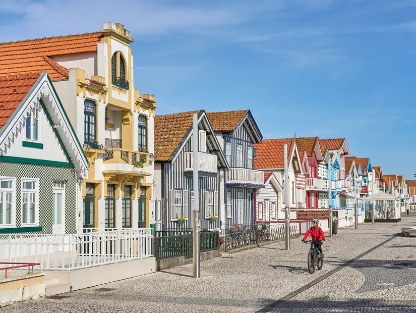 Portekiz'in Aveiro kenti yakınlarındaki Costa Nova do Prado'nun renkli ahşap evlerinin önünde elektrikli dağ bisikletiyle pedal çeviren kadın.