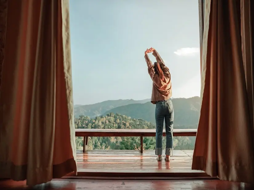Dağ manzarasını ve sabah sisini görebilen balkonda dinlenen kadın