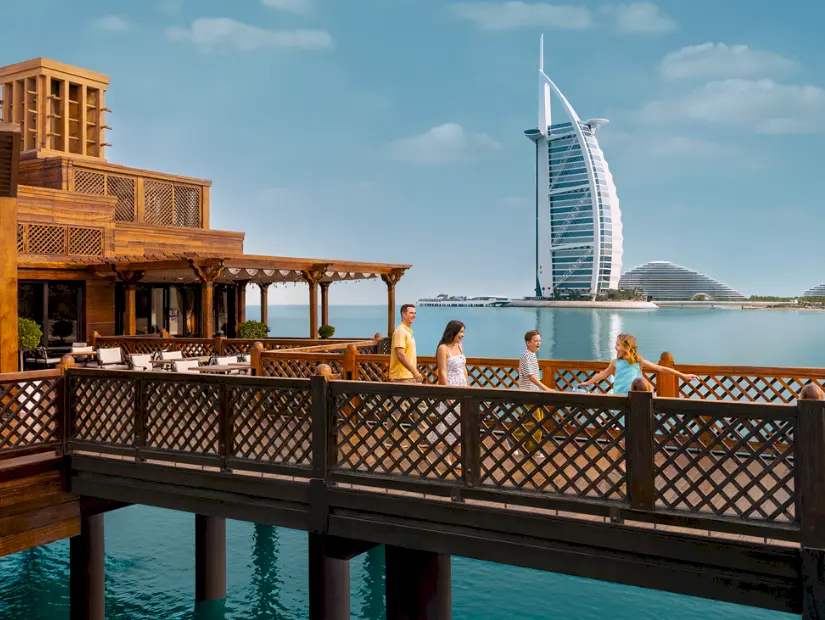 Dubai Madinat Jumeirah ahşap iskelesinde yürüyen aile ve arkada Burj Al Arab manzarası