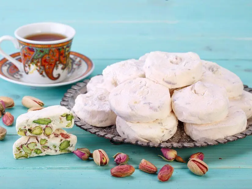 Geleneksel İran ve Fars beyaz nugat tatlısı (Gaz) (İsfahan şehrinden), Antep fıstığı ile birlikte, turkuaz mavisi ahşap bir arka plan üzerinde bir fincan çay 