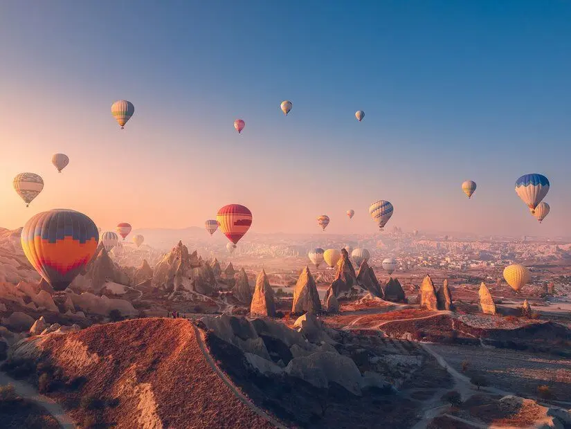 Kapadokya'da muhteşem gün doğumu manzarası, derin kanyonlar ve vadiler üzerinde gökyüzünde süzülen rengarenk sıcak hava balonlarıyla. 