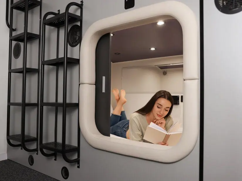 Kapsül tipi hostelde kitap okuyan genç bir kadın.