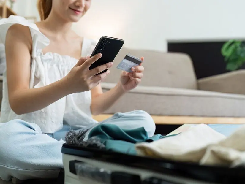 Kredi kartıyla seyahat acentesinden tatil rezervasyonu yapan veya online otel rezervasyonu yapan mutlu genç kadın.