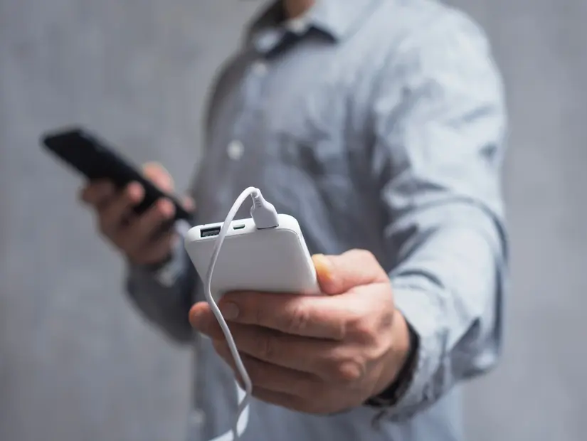 Gri beton bir duvara karşı Akıllı Telefon ve Güç Bankası tutan tişörtlü bir adam