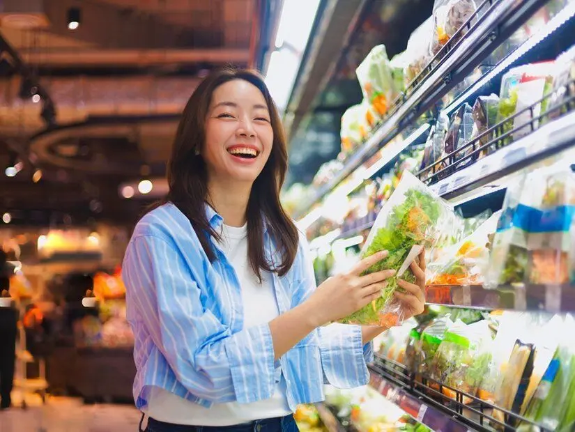 Süpermarkette alışveriş yapan Asyalı kadın, gülümseyerek sağlıklı yiyecekler seçiyor