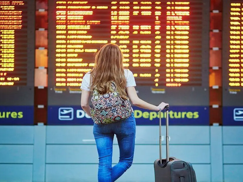 Sırt çantası ile güzel genç turist kız ve uçuş bilgi kurulu yakınında, uluslararası havaalanında bagaj taşımak