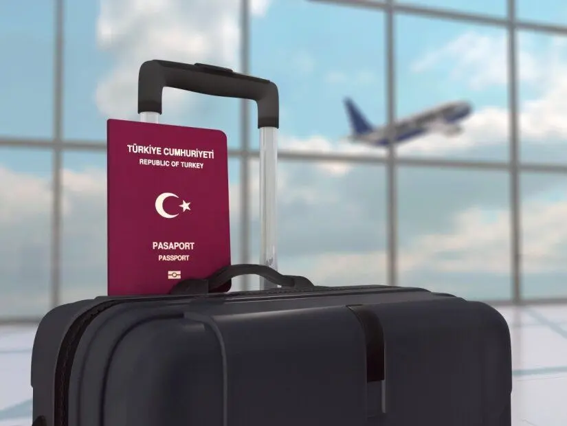 Siyah bagaj çantası üzerinde Türkiye pasaportu ve uçağın kalktığı odaklanmamış havaalanı arka planı