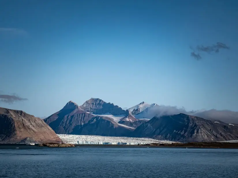 Norveç'in Svalbard şehrinde, açık mavi gökyüzünün altında kutup dağları ve buzulların çarpıcı bir manzarası, doğal güzellikleri ve sükuneti gözler önüne seriyor.