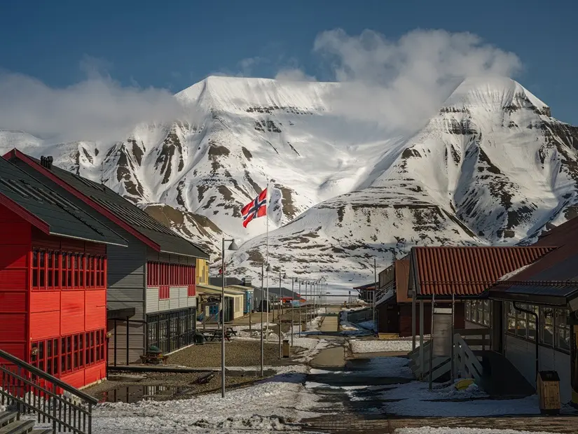 NORVEÇ'İN BAĞIMSIZLIK GÜNÜNDE BOŞ BİR LONGYEARBYEN SOKAĞI, PARLAK RENKLİ DÜKKANLAR VE ARKA PLANDA KARLA KAPLI BİR DAĞ, ARKTİK'TE SVALBARD'DA GÜZEL BİR GÖKYÜZÜ