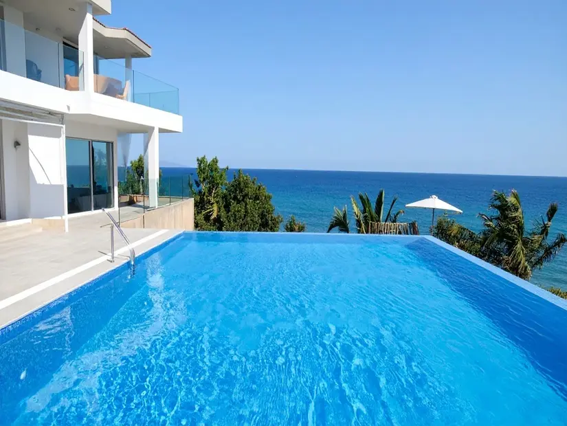 Modern beyaz bir villadan okyanusa bakan şaşırtıcı sonsuzluk havuzu. 
