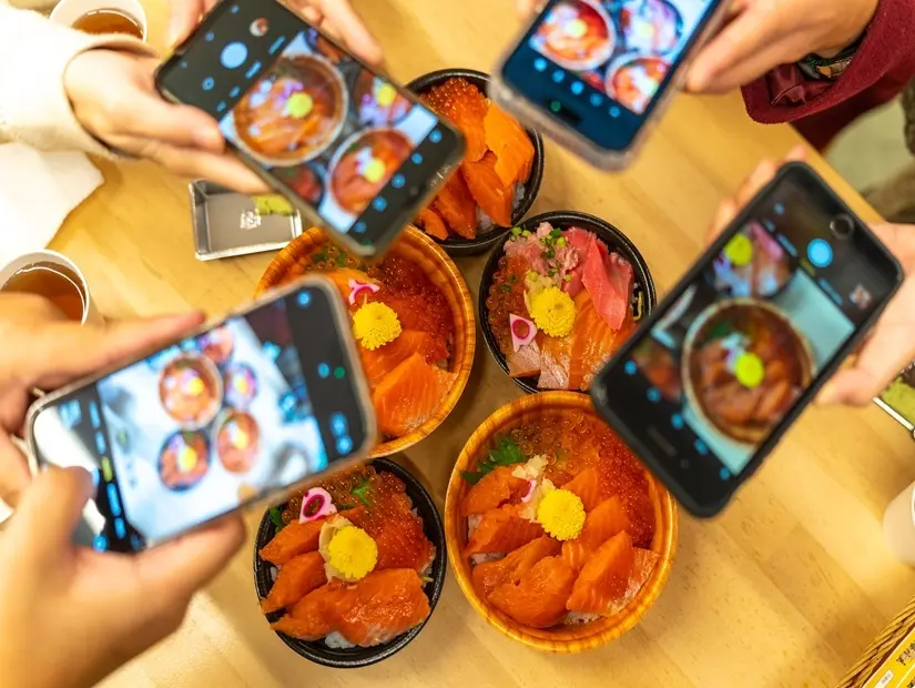  Japonya'nın Tokyo kentindeki bir balık pazarındaki bir restoranda cep telefonuyla deniz ürünleri sashimi pirinç kasesinin fotoğrafını çeken bir grup insan